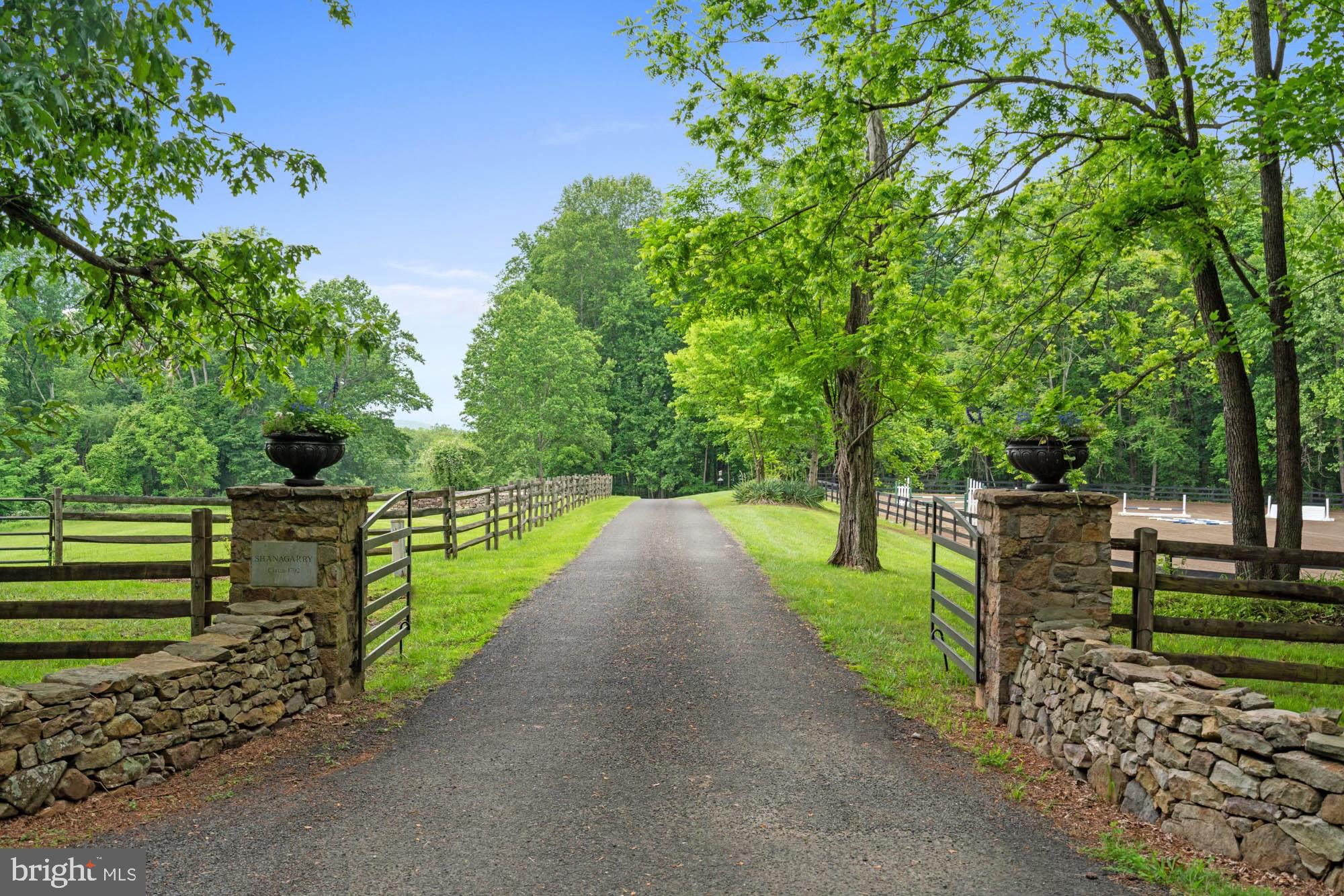Shanagarry Farm on more than 51 acres is available for the first time in nearly four decades. A bucolic estate near the foothills of the majestic Blue Ridge mountains in Castleton, Virginia just 15 minutes from Warrenton. Shanagarry means “old garden” in Gaelic and these gardens certainly deliver on the name. They’re full of rare, antique varieties of roses and heritage plants surrounded by 150 year old boxwoods highlighted by tiered flagstone terraces with a salvaged millstone inlayed within the entrance courtyard. The four bedroom farmhouse dates back to the 18th century. In fact, letters written in quill pen were discovered in the walls and date back as far as 1792. Much of this family home embraces the elegant history with original wide floorboards in the formal dining and living room including an antique wood burning stove. The warmth and character is carried throughout two levels with reclaimed floors and beams, a pantry door from the former Gold Cup course and a barn stall door used as an interior wall. It’s a home of tranquility and splendor where every corner whispers tales of timeless charm and boundless potential. The bright kitchen featuring lacquered wood countertops and a new Viking range opens to a double height eat-in sunroom with views of the rear grounds, covered stone terrace with pizza oven and dazzling views of a nearly one acre pond stocked with Bass, Catfish and others along with incredible birdlife. The oversized family room is designed for entertaining and features a custom wet bar with backlit bottle storage and two wine refrigerators. You’ll find two more bedrooms in the 1800’s chestnut log cabin straight out a storybook which captures the essence of rustic elegance. It was originally built just outside of Gettysburg, Pennsylvania and dates back to 1824. The cabin features a stone fireplace, custom wet bar made from original boards found on the farm and a living room projector system with drop down screen to stream your favorite series and movies. Shanagarry Farm also features a six stall bank barn with generous stalls, drive-in hayloft, rubber non-slip footing, heated wash stall, paneled tack room, numerous paddocks, two run-in sheds and a generous riding arena. Unparalleled privacy and serenity doesn’t mean you’re isolated. Shanagarry Farm is located in Virginia’s thriving restaurant and winery territory, just ten minutes from three star Michelin rated, Inn at Little Washington, Patty O’s Cafe and Bakery, Blue Door Kitchen and Inn as well as Glen Gordon Manor. Sperryville is only 15 minutes away which is home to Three Blacksmiths and the threshold of Shenandoah National Park. Embrace the allure of country living at its finest in this farmhouse estate where every sunset plants a masterpiece against the rolling hills.