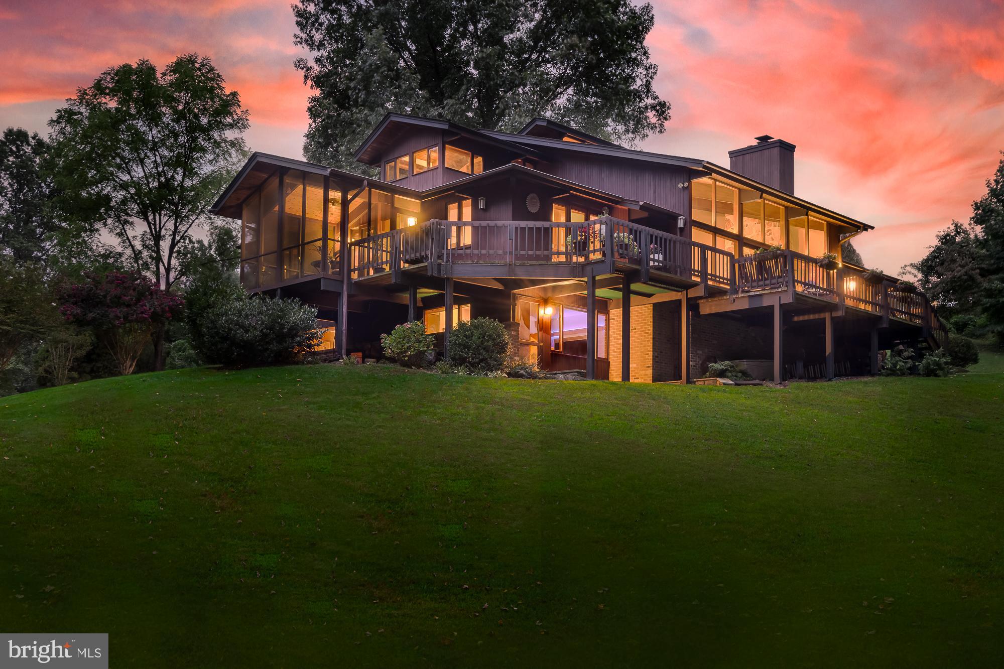 Welcome to this stunning contemporary and rare custom built Deck Home.  
Through the use of complementary cedar, mahogany and brick materials and colors, this Deck Home is perfectly harmonized with its natural surroundings, forming a unique and masterful sense of elegance and calm.  This is truly a one of a kind home that is not found in this area.  The main home spans 4,834 finished SF on 1.95 acres to include an 1,824 SF garage and workshop.  This home offers a serene retreat, backing up to Mason District Park. This park offers access to scenic trails, an amphitheater, sports fields, a playground and more right from your doorstep.
The residence features an open floor plan enhanced by soaring cedar ceilings with wood beams, bringing a sense of spaciousness and light. Floor-to-ceiling windows in the two-story living room offer panoramic views of the surrounding forest, while a stone natural wood fireplace with a slate hearth and mahogany mantel adds a touch of rustic charm. The living area is complemented by a wet bar with quartz countertops, a wine refrigerator, and custom-designed mahogany shelving, perfect for entertaining.
The expansive kitchen features a center island, soft-close drawers, quartz countertops, and top-of-the-line  appliances, including a cooktop, refrigerator, oven, and microwave. Large windows in the kitchen offer panoramic views of the surrounding landscape, seamlessly integrating the indoor space with the outdoors. Adjacent to the kitchen is a screened porch with a vaulted cedar ceiling and ceiling fan, providing a delightful space to further enjoy the picturesque setting.

The main level includes a luxurious BR suite featuring a built-in platform bed, cedar-lined walk-in closets, and cathedral ceilings. French doors open from the bedroom to a deck, offering beautiful views. The main bath has been meticulously renovated with a walk-in shower, a soaking tub, and heated floors. Additionally, a second bedroom with a separate bath is also located on this level, providing both comfort and privacy.

Upstairs, an expansive loft area opens to a 3rd BR with a private outdoor Trex deck, a bathroom with skylight, & exquisite office space.  The office is designed to inspire productivity and creativity, featuring breathtaking 180-degree views that immerse you in the beauty of the surrounding landscape. The room is bathed in natural light from surrounding windows, creating a bright and inviting atmosphere.  The office is furnished with a custom-built cherry desk, which exudes sophistication and craftsmanship. This elegant desk provides ample workspace and integrates seamlessly with the room’s design, making it a perfect setting for both work and reflection.

The finished lower level offers a spacious suite to include a 4th bedroom with a full bath, den, and large entertainment area.  Unique to the lower level is its spa like atmosphere which includes a large cedar lined dry/wet sauna to help maximize your health and well being.   The suite provides convenient access to the outdoors, enhancing your living experience with seamless indoor-outdoor flow. Additionally, the large storage room features a high ceiling and custom shelving for all your storage and organizational needs.

This home features a 3-car Attached Garage with Custom Cabinetry and a Fully Renovated Detached Garage/Workshop, which includes Heated Floors and Extra Storage or Vehicle Space.

Improvements:   Modern HVAC Systems |  Roof Replacement for  Main House &  Detached Garage |  All-New Skylights | Custom Gutters | Renovated Detached Garage/Workshop with Custom Cabinets | Custom Workbenches |  New Garage Door | Heated Floors | Newer  Washer and Dryer | Repaved Driveway | Custom Lighting throughout | Swarovski Crystal Chandelier in the Foyer.

This Deck Home, with its harmonious blend of natural materials and contemporary design, offers a unique and inviting living experience.  Don’t miss your chance to own one of the most unique homes in Northern VA