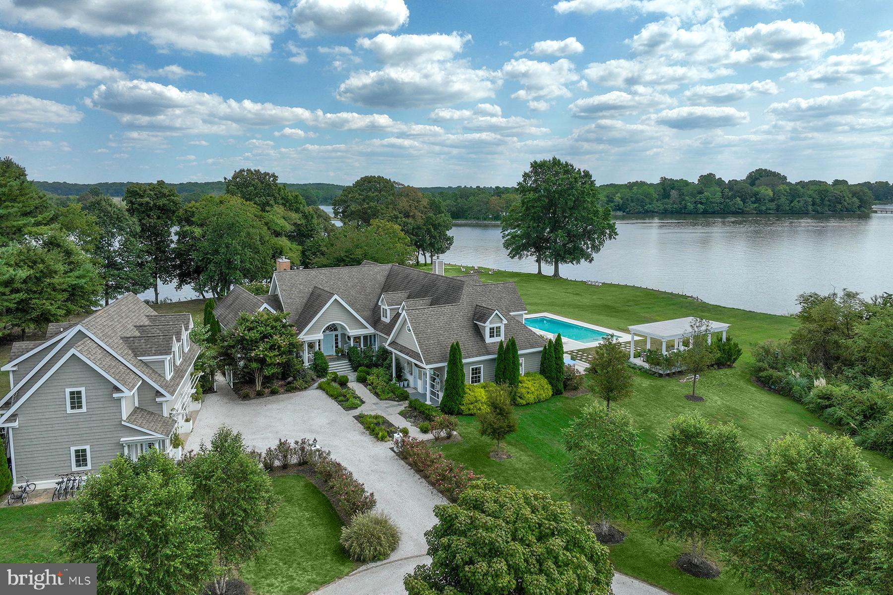 Experience unparalleled luxury and serenity at 141 River Run, a stunning 3.45-acre peninsula with sweeping views of the Wye River. This property blends a gorgeous setting with a luxurious interior in an extraordinary way, from garden paths of lush roses opening to a peaceful sitting area, to a waterfront recreation room that can be opened on both sides to get the breeze from the water. Once you arrive at 141 River Run, you won’t want to leave  because all the fun happens on site: swimming in the saltwater pool, crabbing off the dock, taking the boat for a spin on the Wye River, hanging out at the waterside bar, late afternoons with a book beneath the poolside pergola and evenings under the stars in the hot tub. The updated private pier accommodates two boats — one with a lift. A boat ramp and waterside deck complete the offering..
What makes this property so special – beside the approximately 700 ft of shoreline -- is the complete feeling of relaxation that encompasses you upon arrival. It is peaceful and authentic, yet there’s an underlying elegance to the coastal finishes.  When you step into the foyer with its Palladian window, the living room and its cathedral ceiling, built-in shelving, gas fireplace, and French doors that open to a charming patio with a pergola, seems to merge completely with the gardens and water beyond. The home was designed to offer water views and privacy from almost every room. Adjacent is the great room where your family or guests will find happiness helping the chef or relishing the views from a comfy seating area. The soaring ceiling and walls of windows frame the water and grounds. This chef’s dream space has high-end stainless-steel appliances, a beverage fridge, dual ovens, marble countertops and backsplash, and a central island with bar seating. The space effortlessly connects to a dining area which can easily accommodate ten people but does not feel overly formal. The screened porch is a delightful place to enjoy a meal too, with direct access to the pool.  
The main level owner’s suite is privately situated at one end of the home, with waterside access and a private lounging deck, and features a spacious bedroom. The newly renovated, spa-like bathroom offers two separate spaces individual privacy, a soaking tub with waterfall faucet, and a fabulous water view shower. Separate, custom built closets will help with organization. There are two additional bedrooms on the main level that share a renovated hall bath – one of the bedrooms has water views. There is a lovely water view office, formal powder room, and a full bathroom that’s perfect for guests to access from the pool. Upstairs there’s a second huge owner’s suite with a private waterside deck and deluxe bathroom. The upstairs suite has several additional rooms that would be perfect for exercise, a second office, or a nursery. 
The attached converted garage now functions as a versatile indoor/outdoor game room with contemporary clear garage doors on both sides and a full bar overlooking the hot tub, pool and river. An auxiliary wall unit keeps this space warm in winter and cool in the summer. A 2-car detached garage, complete with an adjoining workshop, has a fully updated in-law suite above. This stylish space includes a living room, a full kitchen with an island, bedroom, bathroom, laundry, and a bunk room.
In addition to extensive interior renovations, the owners have thoughtfully and meticulously updated the exterior amenities. Outside, a newly surfaced pea gravel driveway, extensive new plantings including dozens of specimen trees and plants, a kitchen garden, and two sheds. The expansive salt-water pool, hot tub, and deck provide the perfect backdrop for warm weather relaxation or entertaining. Conveniently located, it’s an easy boat ride for lunch at Kent Narrows, St. Michaels, or Annapolis, and with a short drive to the Bay Bridge, this exceptional property is ideally situated for commute access.
