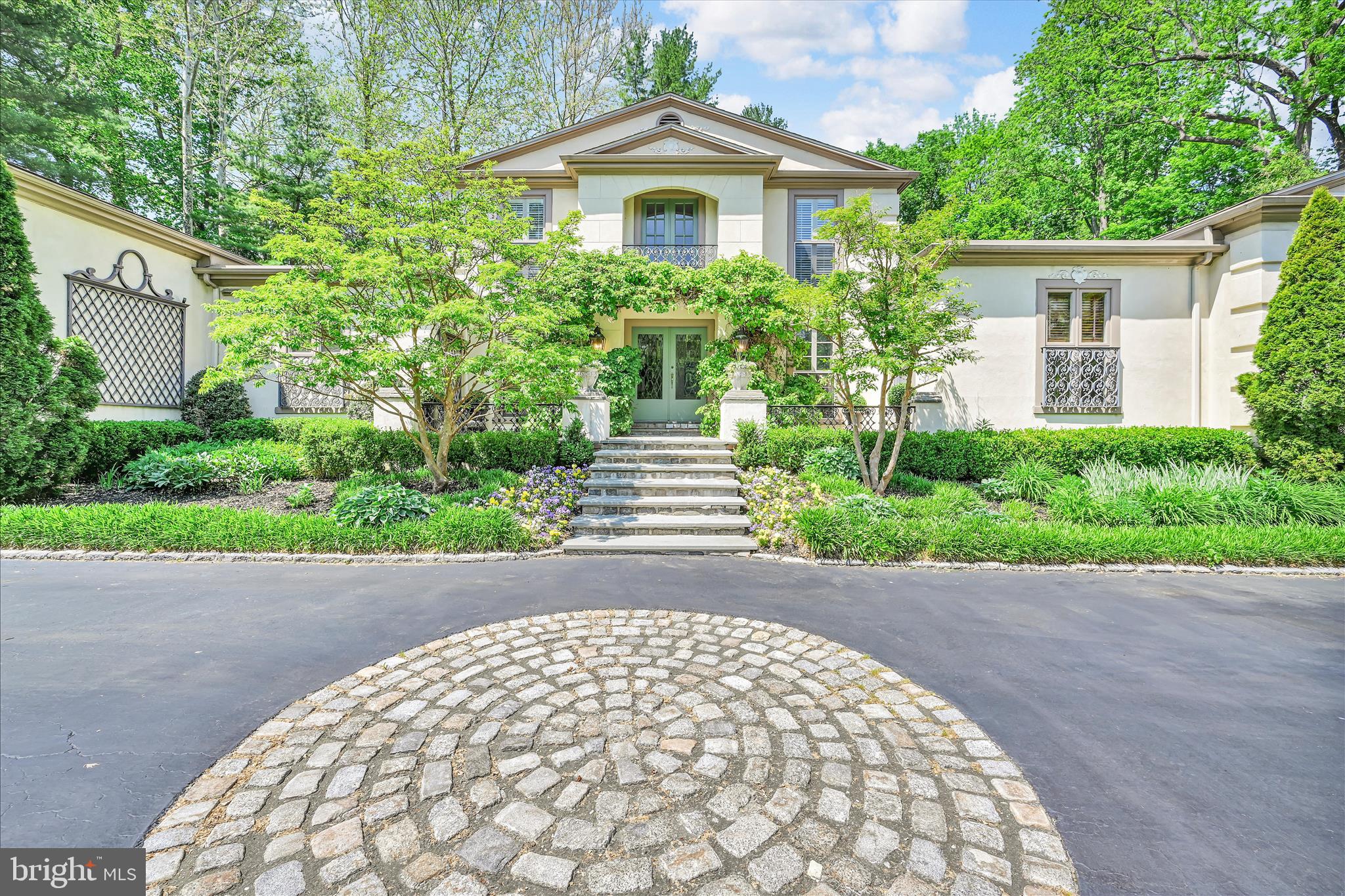 Nestled in the heart of Gladwyne, this custom French Château-inspired home blends timeless European elegance with beautifully updated modern living. Offering 5–6 bedrooms and 4.5 baths, this extraordinary residence showcases stunning architectural details, expansive living spaces, and exceptional craftsmanship throughout.
A grand double-door entrance opens to an impressive foyer designed for entertaining, complete with a stylish bar area and seamless access to the main living spaces. The gourmet kitchen is the heart of the home, featuring a large center island and a dramatic atrium window that floods the space with natural light — perfect for both everyday living and hosting unforgettable gatherings.
The main level offers remarkable versatility, including: A luxurious first-floor primary suite with separate his-and-her baths and generous closet space, An additional first-floor bedroom, an office (6th bedroom), A game and entertainment room with 12ft. ceilings, Elegant formal living and dining rooms and A spacious family room. Three fireplaces — two wood burning and one gas  — add warmth and charm throughout the first floor.
Nearly every main living area opens to the stunning rear flagstone patio, surrounded by lush perennial gardens, a tranquil outdoor water feature, mature trees, and picturesque stone walls that create a private, serene setting.
Upstairs, you’ll find three additional bedrooms, including: One bedroom with its own en-suite bath and Two other bedrooms connected by a Jack-and-Jill bathroom. 
This exceptional residence blends sophisticated European elegance with modern comfort, thoughtful functionality, and stunning outdoor living spaces, all within one of the Main Line’s most prestigious communities. Ideally situated just minutes from charming local villages, fine dining, transportation, premier shopping, King of Prussia, and Philadelphia, this remarkable home offers an unparalleled balance of privacy, luxury, and convenience.