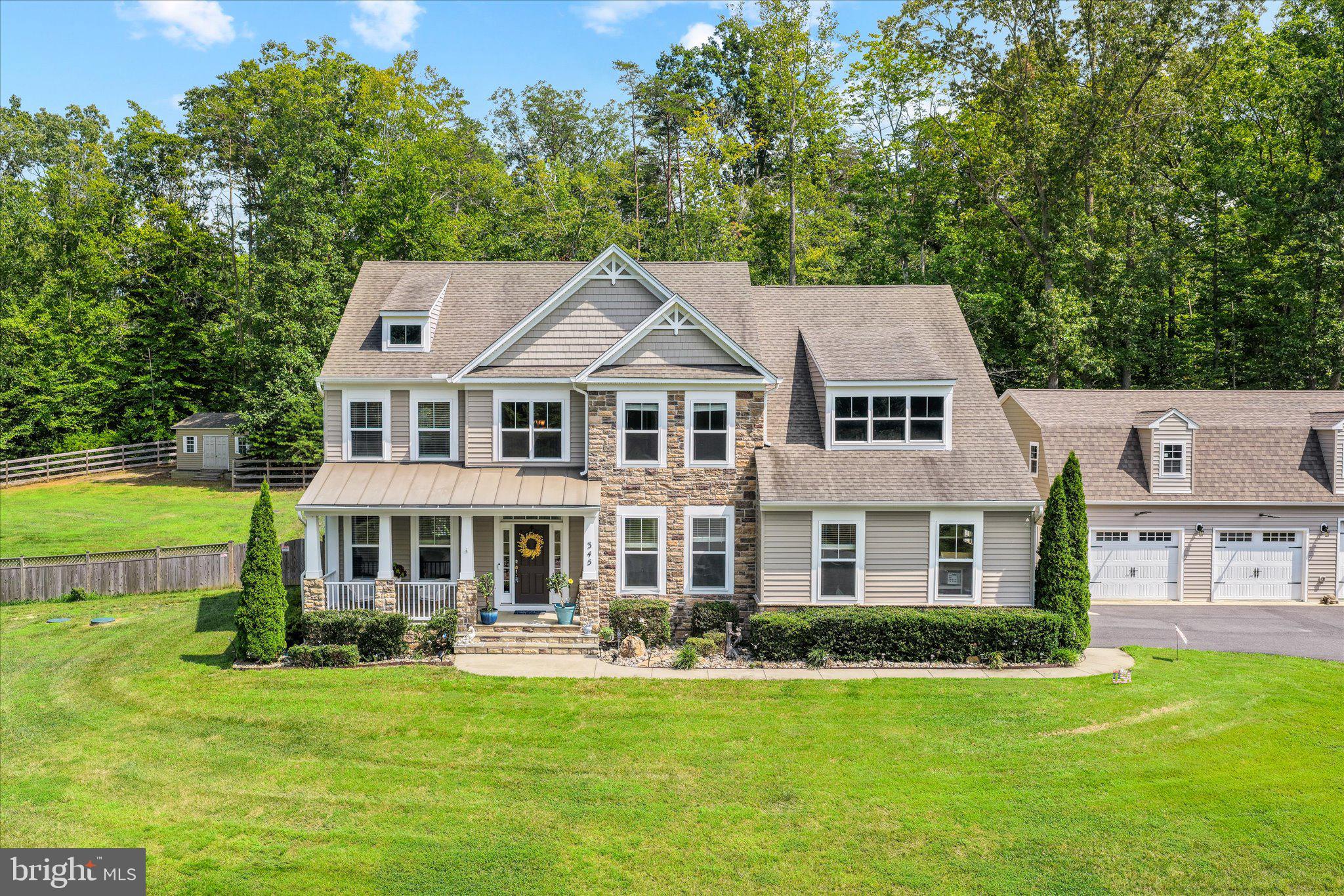 There is something undeniably special about this home... spanning its pool utopia, five- car garage spaces (and room for a workshop/home office!) and incredible updates. Introducing 345 Long Meadow Drive!
Nestled on a 3.09-acre corner lot in Stafford Estates, this residence offers 5 bedrooms, 4.5 baths and approximately 5,000 square feet of beautifully balanced living space. It was built in 2015 and has been meticulously cared for (and upgraded!) under its current owners’ care since 2022. Set on a gentle rise, the front yard welcomes you with a slight slope, manicured bushes hugging the home’s sandy beige stone façade and an inviting covered porch that sets the tone before you ever step inside. As a corner lot, it offers presence and privacy, with the side yard sloping more subtly and hardwoods framing nearly half the property. The backyard is where this property truly shines as a personal resort! Fully fenced, with a secondary fence securing the pool area, it is designed for both fun and peace of mind. The like-new, custom pool is a total showpiece: three lighted waterfalls cascade against a stone wall, a colored lighting system transforms evening swims, and an 18-inch ledge runs the entire length, perfect for partial submersions in
the water. An oversized heater extends the swim season, while a top-grade cover and Polaris cleaning robot keep maintenance seamless. A pergola anchors the entertainment area, and beyond the fence line, wooded acreage invites exploration and even sledding in winter months! Car enthusiasts and hobbyists will appreciate the rare combination of an attached two- car garage with whole-house surge protection and generator connection, plus... a custom- built 3-car garage complete with electricity, water access, large ceiling fans and an expansive loft. The owner thoughtfully used the upper-level space for woodworking and acrylic projects, but the possibilities are endless. WOW! Inside, the main level flows effortlessly. To the right, a private office with two windows; to the left, a built-in-lined library. Hardwood flooring carries through the foyer, dining room and into the heart of the home - a light-filled family room with gas fireplace and a gourmet kitchen featuring granite countertops, stainless steel appliances, gas cooktop, double-door pantry and an island with bar seating. Just beyond, a sunroom wrapped in windows opens directly to the pool. Fresh carpet enhances the office and living areas and wrought-iron stair details add understated elegance. Upstairs, the primary suite is bathed in light from five windows and offers two walk-in closets and a spa-like bath with separate tub and shower. One secondary bedroom enjoys an ensuite bath, while two others share a hall bath. A generous linen closet adds practical storage. The walk-up basement is designed for entertaining, with a 12-foot wet bar complete with two refrigerators, beermeister, water access and dual wine racks. Additional lower-level highlights include a full bath, flex room and tons of storage. Systems-wise, the home is equipped with two furnaces, sump pump with battery backup, water softener and newer 80-gallon hot water heater. An ADT security system and irrigation system add further peace of mind. Everything has been wonderfully maintained! Life in Stafford Estates includes an active HOA with annual chili cook-off, a Thanksgiving turkey trot and even Santa arriving by fire truck. All of this is within 10 minutes of shopping and dining along Route 17, 10 minutes to Curtis Park and The Gauntlet golf course, and just 20 minutes to the heart of downtown Fredericksburg. This property is also located approximately two miles away from the new high school and elementary school opening this fall (2026). 345 Long Meadow Drive is the total package - a rare blend of privacy, community and absolutely extraordinary features!