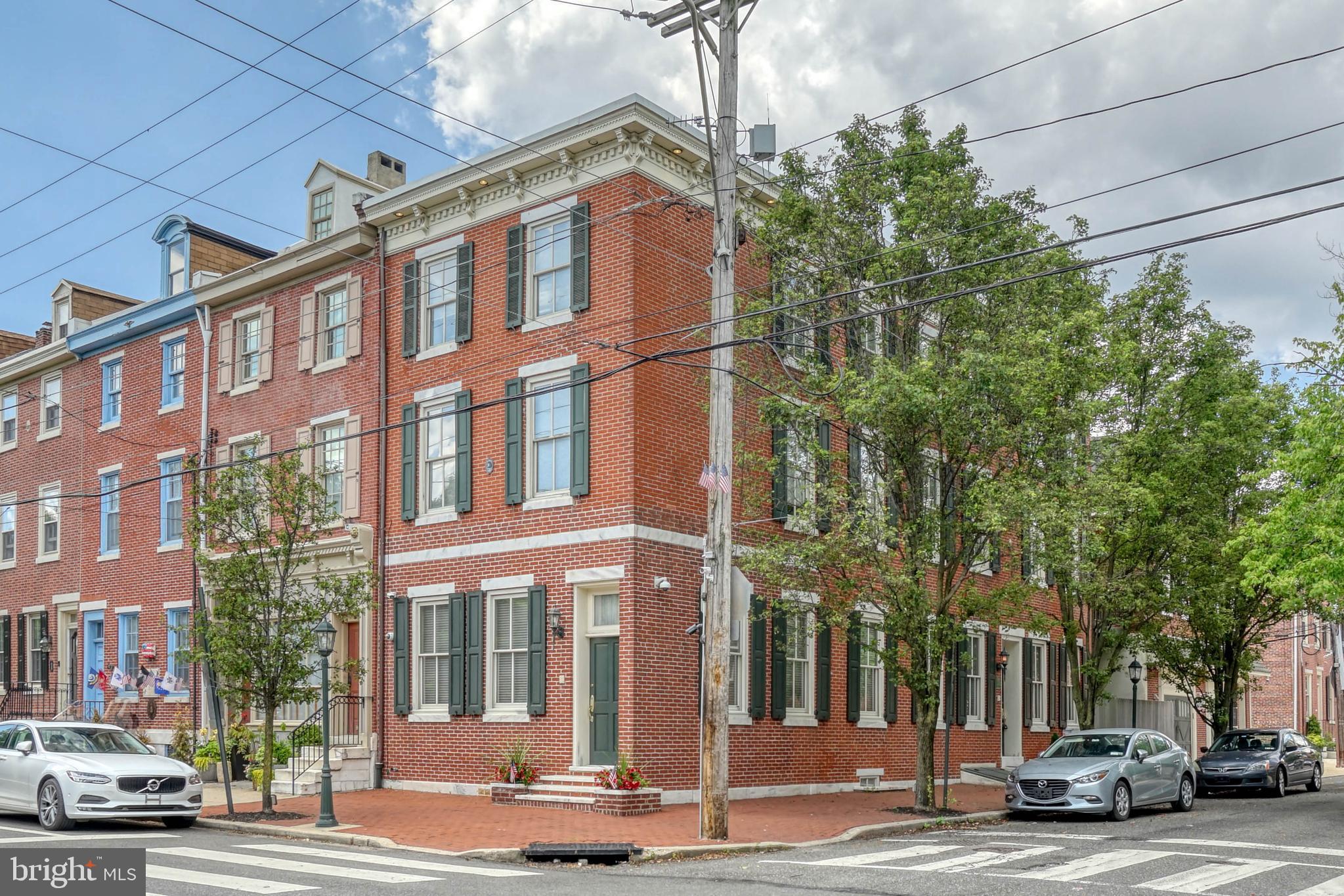 Unique landmark single-family home, 824 S. Front Street aka 104 Queen Street. 
One-of-a-kind is the only way to describe 824 S. Front Street aka 104 Queen Street. Sitting prominently along the corner at Front and Queen Streets, this home  was transformed into a stately city mansion offering 5 bedrooms and 3.5 bathrooms, The exterior of this towering 3-story home is historic Philadelphia at its best, featuring a pristinely kept red brick facade and tall windows framed by shutters and marble stone. Inside, the expansive main level is made for entertaining with plenty of room for guests to gather and two street level entrances. It's completely open and filled with natural light from nine windows that trace the north and east walls. Ornate banisters trim openings to the family room, kitchen, and staircase below, creating a bright, airy feel. The center opening extends up all three stories to a skylight on the roof, forming a lightwell in the middle of the home. Beautiful hardwood floors extend to a mudroom with a storage closet and a closet for the gas furnace plus you'll also find the gas water heater and a washer/dryer. Additionally, on the lower level of the home, there's a cozy family room with a fireplace, built-ins, and an aquarium at the front. In the middle, the dining area flanks one side of the staircase, with a pantry and powder room on the other side. The large kitchen is fitted with inset cabinetry, top-of-the-line stainless steel appliances, a wood-burning pizza oven, and a peninsula with seating. Off the kitchen, there's a secluded courtyard patio, perfect for enjoying a morning cup of coffee or an evening glass of wine from the humidity-controlled wine cellar. The home's second level has three bright bedrooms, one currently used as a walk-in closet, and a full bathroom with access to a private balcony. On the third level of the home, the primary suite sits at the front. There's a large bedroom anchored by a fireplace, a spa-like ensuite bathroom equipped with a dual head rainfall shower, a bidet, and a full walk-in closet. Completing this level is another bedroom suite and a laundry closet. All this located in the highly sought-after Queen Village earning a Walk Score of 89! Nearby, South St is lined with friendly shops, popular restaurants, and markets, including Whole Food. Target, Wine & Spirits, Ikea, and Lowes are also close by. Plus, multiple parks are within walking distance, and there's easy access to I-95 and South Jersey. Schedule your in-person or virtual tour today!