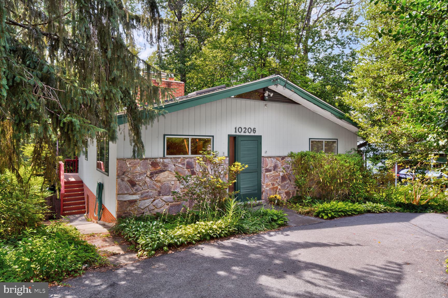 Welcome to 10206 Frederick Avenue, a mid-century modern treasure in the heart of Kensington. Perfectly sited on a beautifully landscaped .29-acre lot, this architectural gem offers a rare combination of privacy, character, and walkability to everything that makes Kensington such a beloved community. A circular driveway welcomes you to this secret retreat hidden behind mature landscaping. Step inside and prepare to be captivated by the unique mid-century modern architecture with vaulted ceilings, skylights, and a wonderful sense of open space. The light filled living room with soaring ceiling, has a wood burning fireplace and custom mantel. The spacious kitchen and dining area continue the theme with the vaulted ceiling, skylights and view to the covered back porch- perfect for morning coffee, or quiet evenings overlooking the beautiful yard.  The layout is ideal for comfortable everyday living and entertaining. Primarily one level living  with an amazing walkout lower level . The  rear of the home offers a truly special experience.  Perched among the trees, it feels like you are living in your own private treehouse. The covered back porch overlooks the spectacular backyard, providing a peaceful setting to unwind and enjoy nature. The main level includes the primary suite with private bath, two more generously sized bedrooms and hall bath with skylight. The walkout lower level includes a family room with gas fireplace, brick wall, and raised flagstone hearth, light-filled home office/ multi-use room, and large laundry/ storage room with front loading Whirlpool washer and dryer. Hot water heater and boiler were replaced at the end of 2016. The rear exterior is simply stunning with a large flagstone patio with steps to a garden area and deep, private, wooded yard. For anyone who wants to walk to BabyCat Brewery  – this is the one! The location is ideal.  This home is a short stroll to what everyone loves about Kensington – its parks, restaurants, shops, Antique Row, the weekly Farmer’s Market, Noyes Children’s Library, the MARC train, and vibrant community events that make Kensington such a special place.  Walk to your favorite spots and come home to this special home enhanced with many special features. Architecturally distinctive, beautifully maintained, and ideally located, 10206 Frederick Avenue offers a rare opportunity to enjoy the best of Kensington living. Welcome home!