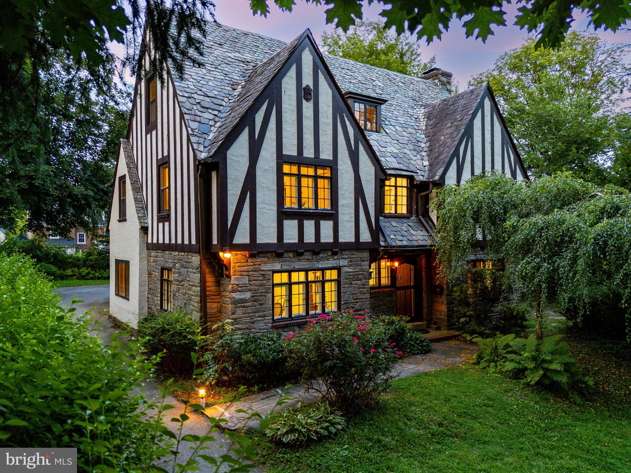 Set back from the street behind a sweeping lawn and mature trees, 1419 County Line Road is a rare offering: a Wallace & Warner-designed English Tudor where architectural integrity, historic detail, and modern convenience come together in perfect harmony.
Built in 1920 and cherished by its third owner for over four decades, this 6-bedroom, 3.5-bath home welcomes you with a curved arched front door, leaded glass, and original slate roof with copper gutters—a testament to the craftsmanship of the era. As you step inside, you’re immediately greeted by the warmth of hardwood floors and a gracious center hall floorplan that flows naturally from room to room.
To the right, the living room spans the depth of the house, filled with sunlight from large divided-light windows and anchored by a double-sided fireplace. French doors open to a flagstone-floor sunroom that feels like a secret garden lounge, ideal for morning coffee or evening unwinding.
To the left, the formal dining room features decorative molding  setting the stage for holidays and special gatherings. The adjacent eat-in kitchen is outfitted with sleek updated cherry cabinetry, granite countertops, stainless steel appliances, and a family dining area overlooking the back patio. A convenient attached two-car garage completes this floor along with a powder room.
Upstairs, the primary suite features a large walk-in closet, and a luxurious oversized bathroom with rain shower. Three additional bedrooms share a large hall bath and large laundry room. The full height third floor offers two more bedrooms and a full bath beneath charming dormer ceilings—perfect for guest rooms, home offices, or creative studios and a lovely sitting area.
Throughout the home, you’ll find hidden treasures: ample storage closets, original hardware, and vintage wood details that speak to the home’s timeless soul.
The location couldn’t be more convenient. From your front door, you can walk 4 minutes to the Rosemont Regional train station and catch the R5,  5 minute walk Ashbridge Parks,  easy access for 476, Bryn Mawr Film Institute, Mom's Market, La Colombe, Skirt and MORE. This is true walkable Main Line living, with easy access to top-ranked Lower Merion schools, Villanova University and three more nationally ranked colleges, and the award-winning Lower Merion Library.