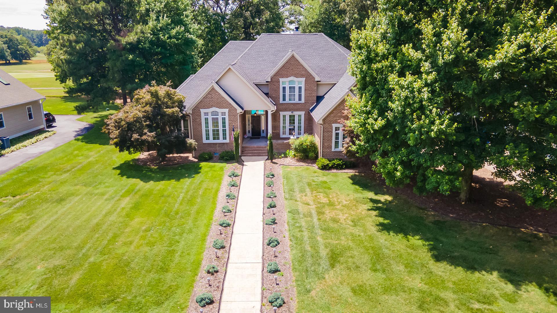 Nestled on a beautifully landscaped 0.61-acre lot overlooking the Nutters Crossing Golf Course, this stately residence combines timeless elegance with exceptional indoor and outdoor living. A grand foyer welcomes you and is flanked by a formal dining room and a distinguished library featuring French doors, built-in shelving, and rich wood flooring. Straight ahead, the sunken living room serves as a stunning centerpiece with a gas fireplace and a dramatic curved wall of windows that frame picturesque views of the private pool and backyard oasis. Designed for both everyday living and entertaining, the spacious kitchen offers abundant cabinetry, a gas cooktop, double wall ovens, a center island with counter seating and pendant lighting, and a bright breakfast nook. The kitchen flows seamlessly into the family room, creating an inviting gathering space. A convenient powder room and main-level laundry room add to the home's functionality. The main-level primary suite provides a luxurious retreat, complete with two walk-in closets and a private sitting room or library featuring French doors, built-in shelving, and a fireplace. The ensuite bath is thoughtfully appointed with a jetted soaking tub, dual vanities, a step-in shower, private water closet, and abundant natural light. Upstairs, three generously sized bedrooms and three full bathrooms provide comfortable accommodations for family and guests. Car enthusiasts and hobbyists will appreciate the oversized four-car garage with two separate entrances, each accommodating two vehicles. Outside, the manicured grounds showcase carefully designed landscaping surrounding the covered front entrance, while the fenced backyard is an entertainer's dream. Extensive hardscaping surrounds the private pool, complemented by colorful flower beds and ample space for large gatherings, outdoor dining, and recreation. Residents of Nutters Crossing enjoy access to a substantial clubhouse and an acclaimed golf course, all within an established neighborhood setting just east of downtown Salisbury. Offering a peaceful, pastoral atmosphere with convenient access to local amenities, this exceptional property presents a rare opportunity to enjoy refined living in one of the area's most desirable communities.