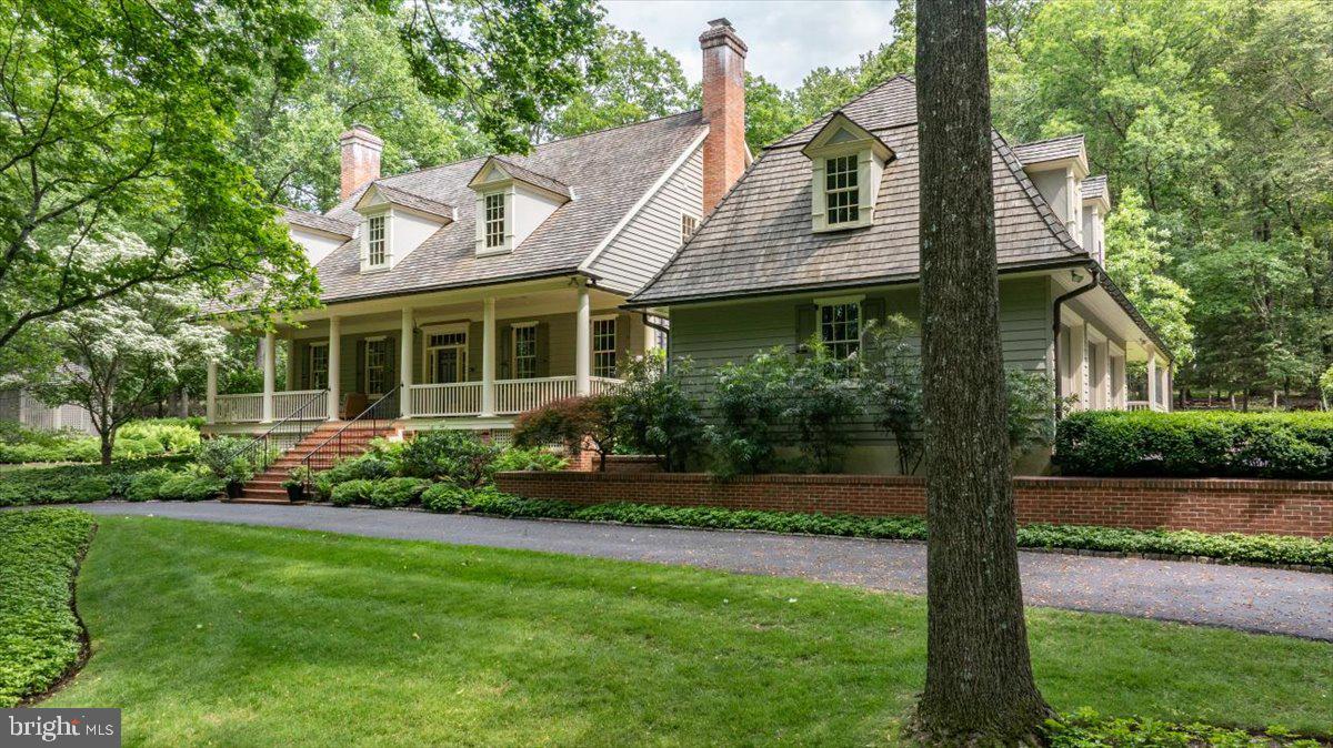 The epitome of refined elegance is presented at 6420 Old Carversville Rd, a sanctuary where tranquility and beauty coexist. This pristine residence is being introduced to the market for the first time, showcasing exemplary architectural design by Lynn Taylor and masterful craftsmanship executed by Jarrett Vaughn.
Ensconced in understated glamour, the home's frontage boasts a covered porch, supported by stalwart columns that frame a welcoming entrance, an idyllic spot for relaxation. The main level is a testament to sophisticated luxury, featuring walnut hardwood flooring, towering ceiling heights, and intricate millwork. The formal parlour emanates style, furnished with bespoke library shelving, a gas fireplace, and an aesthetic reminiscent of Ralph Lauren inspired interiors. The adjacent two-story living room exudes warmth and comfort, filled with natural light from a wall of French glass doors that open to picturesque views of the patio garden and fountain. The gourmet chef's kitchen is outfitted with a recently installed Wolf range cooktop, a bespoke-crafted hood, double ovens, a Sub Zero refrigerator, and a granite-topped center island that is gracefully positioned above radiant heated flooring. This eat-in kitchen is encased by panoramic windows, creating a truly remarkable ambiance for dining. The rear patio, equipped with a retractable awning, allows for effortless entertaining throughout all seasons in a peaceful woodland setting. On more ceremonious occasions, the octagonal dining room is an ideal space for special occasions and features a wall of built-in cabinetry for all of your fine dining accoutrements.  Notably, the spacious primary suite is situated on the home's first level, appointed with a luxurious soaking tub, glass shower, and walk-in closet. On the second level, two guest bedrooms share an adjoined bathroom, while further down the corridor lies an additional spacious en-suite bedroom. The fourth bedroom suite offers ideal guest accommodations, with access from the second floor or a private entrance off the driveway—providing a quiet, comfortable, and secluded retreat. The fully finished lower level boasts a temperature-controlled wine and cigar cellar, a mini bar, a gym area, a gaming room, and an abundance of additional storage space. Exquisitely manicured exterior landscaping, a charming cottage garden, a full house generator, copper gutters, cedar shingles, and extensive brick walls complete this impeccable property. The quaint township of Carversville, nestled in the heart of Bucks County, PA, boasts a rich history that harks back to the 1700s and continues to flourish as a coveted residential address. Sitting in proximity to the captivating old mills on the Paunacussing Creek, the recently refurbished Carversville Inn, the renowned Black Bass Hotel, the Lumberville General Store, and a variety of cycling trails offering sensational views of the Delaware River, this location is the epitome of a country retreat.  Despite its tranquillity, Carversville is still conveniently located close to all main commuter routes, and proudly sits within the boundaries of the acclaimed New Hope Solebury School District.  We cordially invite you to tour this exquisite residence for an intimate glimpse into the embodiment of residential perfection.