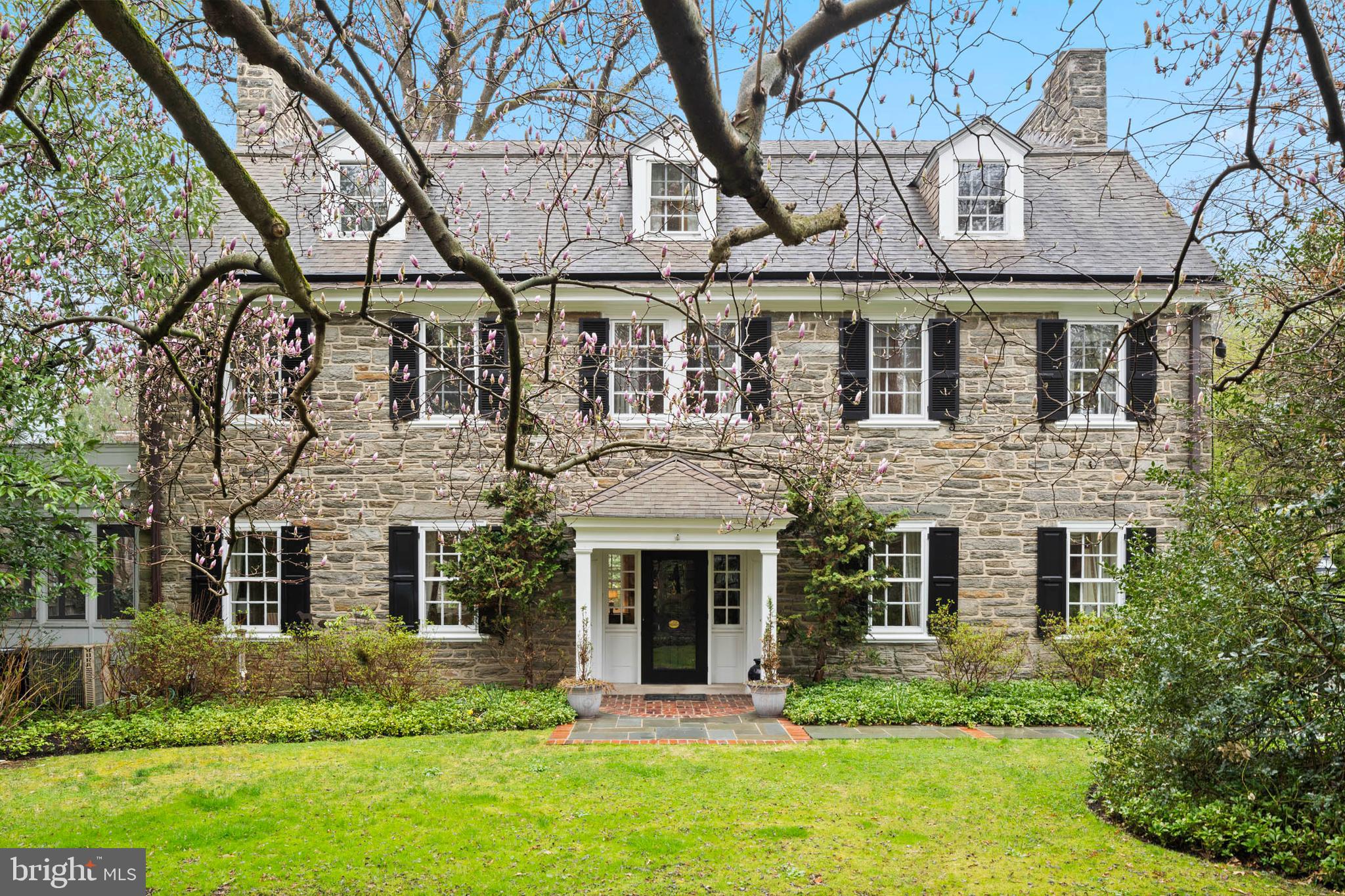 Nestled along West Bells Mill Road near the entrance to Forbidden Drive sits this timeless center hall colonial that offers a blend of historic charm and modern comfort. Surrounded by mature trees, lush gardens, and wildlife, this home feels like a private retreat while remaining conveniently close to vibrant shopping and dining options in Chestnut Hill. A Dutch door welcomes you into the gracious center hall, where original, random-width hardwood floors set the tone for the home’s enduring elegance. At the rear, a second Dutch door opens to a beautifully designed slate patio, gracefully shaded by a mature canopy tree and framed by lush, thoughtfully curated gardens—an inviting outdoor room ideal for quiet reflection or effortless entertaining. The inviting living room features a wood-burning fireplace with a granite mantel, crown molding with picture rails, and a bay window flanked by custom built-ins. French doors lead to a charming screened porch with a brick floor and access to the patio. Original glass-paned French doors open to the formal dining room, showcasing classic wainscoting, a fireplace with stone mantel, and a beautiful arched built-in. A cozy den with built-in bookshelves and adjoining powder room offers a comfortable spot for reading or unwinding. The thoughtfully updated kitchen features granite countertops, custom cabinetry, a large center island with Wolf range, and a vaulted, beamed ceiling. High-end appliances include Viking double ovens, a Miele dishwasher, and a paneled refrigerator. The kitchen offers access to the patio, while a charming vestibule connects to the driveway—providing convenient everyday entry for family and friends alike. Adjacent to the kitchen, the original butler’s pantry adds character and functionality, with glass-front cabinetry, a hammered copper sink, and second dishwasher, and access to the rear staircase. The grand staircase leads to a spacious landing with a large bay window provides a peaceful vantage point over the rear patio. The hallway includes custom built-ins and leads to the study. The light-filled primary bedroom features a wood-burning fireplace, built-ins, and full bath. Two additional bedrooms share a walk-through bathroom, while a separate bedroom suite includes generous closet space and a private full bath. The laundry room offers ample storage space and the original Stiffel & Freeman safe. The expansive third floor includes a very large room with built-ins and abundant storage which is perfect for a play room, studio or entertainment room, a cedar closet, and access to the full hall bath. Two additional bedrooms both with access to an additional hall bath complete the upper level. An in-ground pool and plenty of yard space for a game of football complete this lush, 3.22-acre property that is just a short walk from the trails along Forbidden Drive. This exceptional home offers timeless craftsmanship in a setting that captures the natural beauty and architectural richness of Chestnut Hill. A true legacy property waiting to be cherished by its next steward.
