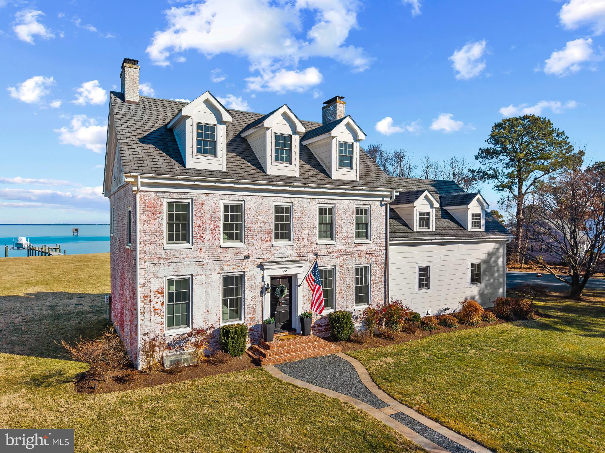 Originally built in 1778 and fully reimagined by Blue Heron Contracting during a meticulous 2012–2013 restoration and expansion, this extraordinary waterfront home in Kent Island Estates offers something rarely found: authentic 18th-century character paired seamlessly with modern coastal luxury.

Set on 1.3 acres with 175 feet of shoreline, the home captures sweeping, unobstructed views of Eastern Bay from every room. Reclaimed pine floors, four original brick wood-burning fireplaces, and pocket doors preserve its historic soul, while thoughtful expansion and design elevate it for today’s lifestyle.

The waterside chef’s kitchen flows effortlessly into the family room, creating an inviting gathering space where walls of glass frame panoramic water views. Whether hosting sunset dinners or enjoying a quiet morning coffee, the Bay is always center stage.

Upstairs, five spacious bedrooms include a generous primary suite retreat. Four fully renovated designer baths,  including heated floors in the primary, blend timeless finishes with refined comfort. A stylish main-level powder room completes the interior.

Outside is where the Chesapeake lifestyle truly unfolds. A private 150-foot pier with 8,000-lb boat lift and sun deck invites spontaneous cruises and long summer days on the water. The bulkheaded shoreline with riprap provides both protection and natural beauty. A 30’ x 26’ waterside paver patio and fire pit create the perfect setting for sunset gatherings overlooking the Bay, all surrounded by expansive lawns and mature trees that offer privacy and serenity.

Additional features include a 26’ x 44’ detached garage with EV charging, workshop and boat storage, partially finished conditioned basement, dual geothermal heat pumps (5 zones), a 20KW generator, and an owned 1,000-gallon buried propane tank.

This is more than a historic home. It is a true Chesapeake Bay legacy property,  where boating, entertaining, and panoramic views become part of everyday life.

Experience waterfront living the way it was meant to be.