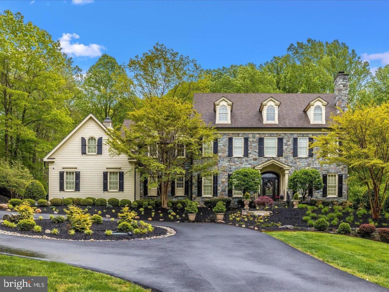 Experience unparalleled luxury in this extraordinary estate, boasting over 10,000 square feet of expertly crafted living space. Designed by acclaimed architect Ted Visnic, this residence showcases timeless design with an impressive use of locally sourced Carderock stone from Bethesda, featured throughout the exterior—from the stately front elevation and twin chimneys to the entry pillars and retaining walls. A newly widened and paved driveway, framed by stone columns and wood fencing, sets the stage for a truly grand arrival. The circular driveway and additional parking pad provide ample room for hosting guests with ease. Step through a solid wood front door beneath a graceful transom and into an expansive foyer with soaring arches, rich wood trim, and custom plantation shutters on every window. Warm walnut flooring is paired with exquisite wood wainscoting, creating a welcoming yet refined atmosphere. The formal living and dining rooms flank the entry and feature large windows and fireplace. A butler’s pantry with wet bar and wine fridge leads seamlessly into the dining area—perfect for entertaining. Sunlight pours into the rear of the home through glass atrium doors, opening to a lanai overlooking a private backyard oasis with new landscaping, a spacious stone patio, and a sport court. The main-level library offers two full walls of built-in shelving, a cozy fireplace, and French doors for added privacy. At the heart of the home lies the gourmet kitchen, complete with custom cabinetry, McKenzie Childs light fixtures, a massive granite island, and high-end appliances including a Sub-Zero refrigerator and freezer, six-burner gas range, double ovens, and designer hood. The adjacent breakfast room is wrapped in windows and flows into a stunning family room with a coffered ceiling, custom built-ins, and yet another fireplace. The walk-out lower level is designed for entertaining, featuring a full guest suite, private patio, wet bar, and a professional home theater outfitted with reclining leather seating. Upstairs, five spacious bedrooms offer comfort and privacy, each with new custom hardwood floors. The primary suite is a retreat unto itself with three walk-in closets and a spa-inspired bath. An additional bedroom suite occupies the top level, complete with new flooring and a private full bath. Modern amenities include a full Control4 smart home automation system with integrated cameras, geo-thermal heating and cooling, and a whole-home generator powered by a 1,000-gallon propane tank. Impeccably maintained and thoughtfully upgraded, this home offers a rare combination of architectural beauty, premium finishes, and everyday functionality.