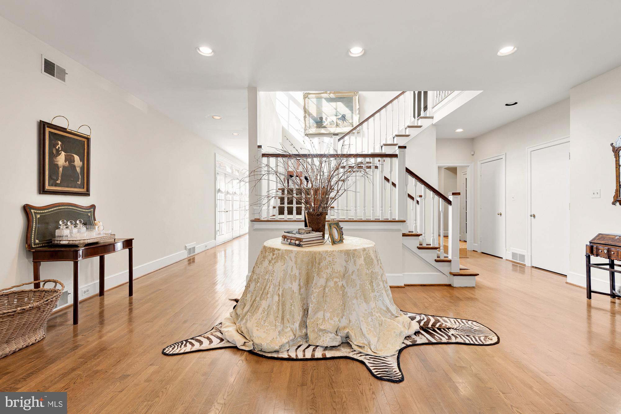 PRICE IMPROVEMENT!  Tucked away from the illustrious Iron Gate Road in the heart of highly sought-after Potomac Village is this handsome country estate. Sited on 2.18 wooded acres, at the end of a winding driveway, the approach makes an inviting yet dramatic first impression. Originally custom-built with interiors inspired by Katherine Hepburn’s Connecticut farmhouse, the home exudes timeless elegance, augmented by a sturdy brick facade and slate roof to withstand the test of time. Surrounded by wisteria vines, double doors reveal ethereal interiors sprawled across a substantial 9,463 square feet. Artistic in the way it flows in, natural light bathes the main staircase in a warm glow. Pocket doors off the foyer reveal a cozy octagonal study, with French doors leading out. The embassy-sized living room, measuring over 32-feet in length, is enveloped in natural light flooding in from skylights in the recessed cathedral ceiling. Two sets of French doors bring the outside in, while a roaring central fireplace, one of four in the home, retains a sensation of warmth within the vast space. Subtly elegant, the oval-shaped dining room features inlaid hardwood floors and overlooks the rear lawn. The country kitchen has been fully modernized, with a commercial grade range top, honed marble countertops, custom inset cabinetry, and a suite of SubZero-Wolf appliances. Touches such as the built-in bookshelf and adjacent breakfast area with fireplace enhance livability. A family room with three walls of windows and as well as a large screened porch overlooking the pool area complete the stunning main level. The primary bedroom’s raised ceilings and large fireplace contribute to the overall feeling of spaciousness, establishing an oasis. Twin walk-in closets and primary baths encompass all of the ubiquitous amenities, including a splendid clawfoot tub nestled beneath exposed wood beams and a walk-in glass and marble shower. Three additional large bedrooms, two full baths, and a cozy upstairs lounge are all thoughtfully designed. The lower level consists of an open space anchored by a billiards room with built-in seating and a recreation room with built-in shelving. A full wet bar, fitness room, lounge, full bath, and exceptional storage augments practicality and enables entertaining. The sprawling verdant lawns are surrounded by mature foliage for total privacy. Extensive hardscaping covers the acres of flat, usable space and includes large flagstone patios. A spectacular 50-foot lap pool with automatic cover sits against this natural backdrop for shaded swims on humid summer days. Timeless design, artfully restrained interiors, and a central Potomac location make 10004 Iron Gate Road the epitome of estate living.
