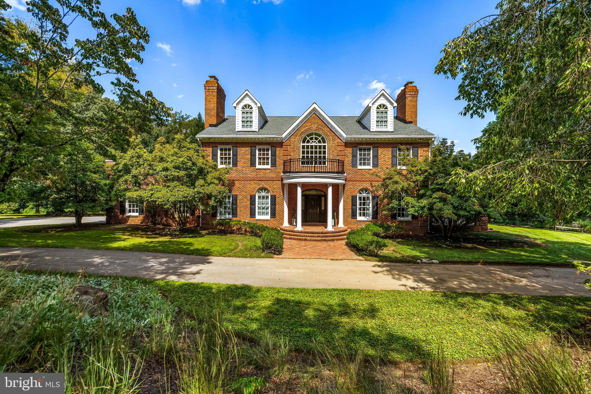 Set within the prestigious Hillstead community of Lutherville, 904 Hillstead Drive is a custom-built Georgian estate offering over 6,500 square feet of elegant, thoughtfully designed living space. With seven bedrooms, five full baths, and two half baths, this stately all-brick home is perfectly situated on a professionally landscaped 2.68 acre lot. Rich architectural detailing, formal and casual living areas, and seamless indoor-outdoor flow create a timeless residence suited for both entertaining and everyday comfort. The main level welcomes guests through a striking two-story foyer accented by black-and-white marble floors, where a semi-circular oak staircase rises beneath a vaulted ceiling. Off the foyer, the living room features hardwood floors, a tray ceiling, and a wood-burning fireplace with a marble mantel believed to be from the H.L. Mencken house. Four sets of French doors open onto a covered porch, extending the living space outdoors. The adjoining formal dining room showcases its own fireplace with a framed brick accent wall, perfect for gatherings both grand and intimate. A butler’s pantry, complete with cherry cabinetry, granite counters, and a glass tile backsplash, connects the dining area to the kitchen. The kitchen is both functional and inviting, featuring cherry cabinetry with custom details, a large island with granite top, and high-end appliances, including Sub-Zero and Thermador. The spacious breakfast area, beneath a coffered ceiling with skylights, opens to a screened porch and a wood deck, creating an ideal setting for casual meals and outdoor dining. Nearby, the richly appointed library offers custom mahogany built-ins, a concealed bar, and elegant finishes. A hall provides flow between the garage, kitchen, and formal spaces, while a main-level powder room off the foyer completes the layout. Upstairs, the second level offers a luxurious primary suite with a fireplace, walk-out access to a private roof deck with hot tub, and a custom-fitted double closet. The en suite bath features a freestanding soaking tub, quartz-topped vanity, rain shower, and beautifully finished tile work. Three additional bedrooms are found on this level, one with a fireplace and custom built-ins, and are supported by a shared bath and a hall bath. A laundry room and walk-out access to a second roof deck round out the floor. The third level offers two more spacious bedrooms, each with walk-in closets, built-in bookcases, and arched dormer windows, as well as a full bath and additional storage. The finished lower level adds flexible living space with a large recreation room, complete with Vermont Castings wood stove and French doors opening to the patio and pool area. A private office, wine room, seventh bedroom with en suite bath, and a half bath provide options for guests, work, and entertaining. The lower level also includes multiple storage areas. Outside, the home is surrounded by mature landscaping, tiered outdoor spaces, and classic hardscaping. A brick walkway leads to the stately front entry, while the rear features multiple covered and open-air entertaining spaces, including a screened porch, expansive deck, and bluestone-bordered patio leading to an in-ground pool with fenced enclosure. With a circular driveway, generous parking, and peaceful privacy, 904 Hillstead Drive offers a rare blend of timeless architecture, modern livability, and gracious acreage in one of Lutherville’s most desirable neighborhoods.
