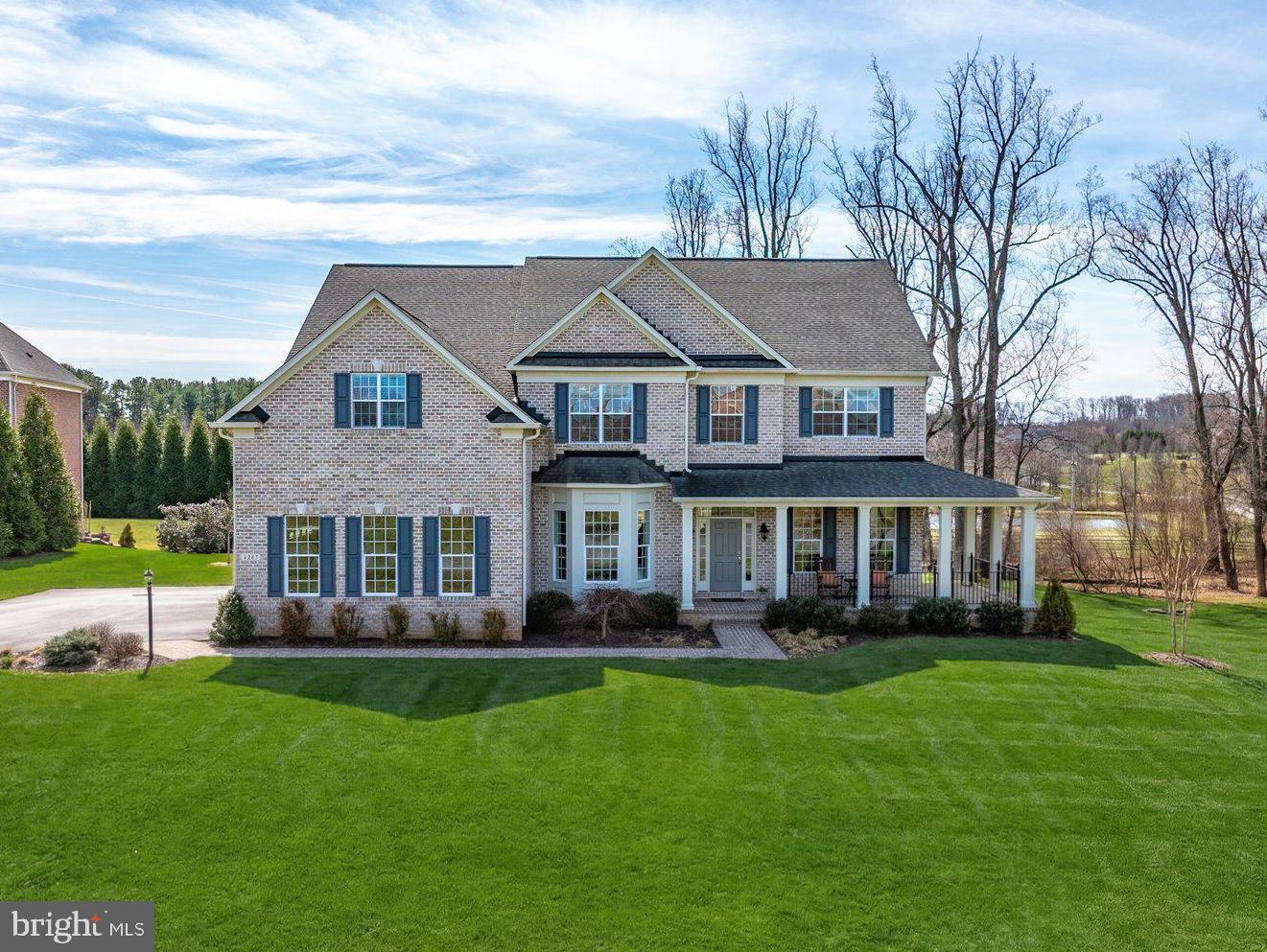 Open House Canceled!  Offer has been accepted. Elegant, timeless, and masterfully customized, this award‑winning Williamsburg Homes Dorchester II offers refined luxury in The Preserve at Clarksville, one of the area’s most prestigious communities. Built in 2014 with classic four‑sided brick construction, this expanded residence sits at the end of a quiet cul‑de‑sac on a premium 1.09‑acre level lot, perfectly positioned to capture sweeping views of the pond and adjacent forest preserve. The result is a rare combination of privacy, serenity, and sophistication.
A 7-foot-wide wraparound front porch sets an inviting tone, offering a gracious welcome and a peaceful place to enjoy the natural setting. Inside, the home’s expanded floor plan showcases ten- and nine-foot ceilings, generous room sizes, rich hardwood flooring, detailed millwork, and a seamless layout ideal for both elegant entertaining and comfortable everyday living. At the heart of the home is the gourmet kitchen, featuring a large center island, upgraded countertops, pantry, abundant workspace, and open flow to the sunlit breakfast room and the expanded family room with a striking stone gas fireplace. From here, access to the outdoor living spaces makes indoor‑outdoor living effortless. A main‑level library/office with an adjoining full bath provides exceptional flexibility, perfect for a guest suite or multigenerational living. The welcoming foyer, flanked by a bright living room and an elegant dining room with bay window and a butler’s pantry, creates a refined first impression. A well‑designed laundry/mudroom is conveniently located just steps from the garage. Upstairs, the luxurious primary suite offers a private retreat with a sitting room, tray ceiling, abundant closet space (three separate walk-in closets), and a spa‑inspired bath designed for relaxation. Three additional spacious bedrooms, plus a 15×17 bonus room/fifth bedroom, provide outstanding versatility for a variety of lifestyle needs. A standout feature is the expansive unfinished lower level, filled with natural light from full‑sized windows and already equipped with a full bath rough‑in. With walkout access to the 680 sq. ft. custom stone paver patio, this impressive space is a blank canvas ready for a home theater, fitness studio, guest suite, or any future vision. Outdoor living is equally exceptional, featuring landscape lighting, a large 980 sq. ft. composite deck overlooking the lush lawn and tranquil pond views, complemented by the custom stone patio below. A three‑car side‑entry garage and Energy Star design with natural gas heating complete the home’s thoughtful and efficient design. Ideally located near River Hill Village Center shopping and dining, and served by top‑rated schools, this extraordinary property offers luxury, privacy, and unlimited potential in one of Clarksville’s most sought‑after neighborhoods.