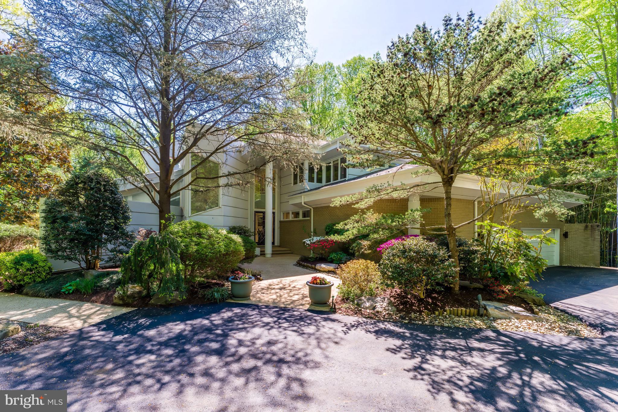 Spectacular does not begin to describe this fabulous residence! Tucked away at the end of a quiet cul-de-sac behind private gates, 9 Oaklyn Court is one of the most striking contemporary residences to come to the market in Potomac this year. Perfectly sited on 2.24 private, level acres with mature landscaping and a resort-style pool, the property offers a serene, parklike setting with exceptional outdoor space and a true sense of seclusion. Designed to impress, the home is filled with natural light, soaring interiors, and captivating views from almost every room. 
A dramatic two-story covered entry introduces expansive living spaces defined by 20+- foot vaulted ceilings, walls of glass, and skylights that flood the home with light. The main level is thoughtfully designed for both grand-scale entertaining and everyday living, with a seamless indoor-outdoor flow. The impressive, step-down living and family rooms are separated by a two-sided gas fireplace, and walls with steps for displaying artwork. The family room has a built-in bar. Each light-filled room has sliding glass doors to the back yard and swimming pool. 
Even the most discerning cook will appreciate the beautiful, renovated kitchen with top-of-the-line appliances, dramatic cabinetry, a center island, built-in buffet, circular designer-glass eating space with stool, and an adjacent eating area that overlooks one of the two large patios, perfect for outdoor eating and barbecuing. Off the kitchen is the dining room with special lighting and floor-to-ceiling windows overlooking the side yard. 
The main level also features the spacious primary suite, a delightful retreat with access to the pool and grounds. The bedroom has a custom wall of built-ins with cabinets, lighted niches, and room for a TV. The adjacent study could also be used as a sitting room, and there are two well-designed large walk-in closets. Two full bathrooms include three separate vanities, a step-up tub, and step-up stall shower. Completing this level are a handsome, cherry-paneled library, two powder rooms, and a large laundry room.
The upper level features four bedrooms, two with en-suite bathrooms and a third full bathroom. The balcony overlook offers an impressive view of the stunning main level.
The light-filled lower level provides a variety of options for informal gatherings. A huge recreation room, lounge with bar area, exercise room, hot tub room and separate bathroom, an additional bedroom with en-suite bathroom, and plenty of storage space complete the interior of this fabulous, approximately 9,900-square-foot house.
The grounds are equally impressive, with a gated, lighted long driveway; beautiful post lanterns; heated pool; expansive patios; and beautifully fenced grounds with room for a future tennis or pickleball court. Ideally located adjacent to Avenel, without the restrictions of an HOA, this exceptional offering combines architectural presence, privacy, and convenience in one of Potomac’s most desirable settings.