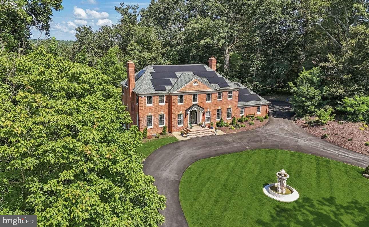 A distinguished contemporary brick colonial in the coveted Potomac View Estates subdivision, thoughtfully remodelled in 2021–22.
Set on a picturesque corner lot of 2.57 acres backing to protected wooded parkland, this home blends timeless colonial architecture with subtle French-inspired elegance. A grand circular driveway with fountain and sweeping manicured lawn creates an unforgettable first impression.

Spanning 6,609 square feet across three levels, the home opens to a soaring two-story marble foyer with ornate wrought-iron staircase and cascading crystal chandelier. Principal rooms include a floor-to-ceiling wood-panelled library, formal living and dining rooms with intricate plaster dentil crown moulding, and a Viking chef’s kitchen with Calacatta marble island, mosaic backsplash, and dual crystal chandeliers.

Four fireplaces throughout — formal living room, family room, Master Suite, and a stone fireplace in the lower level — create warmth across every level. The fully finished lower level features a full second kitchen, wet bar, and projector screen. The Master Suite offers a spa-calibre bathroom with freestanding soaking tub and mosaic art walls.

Outside: a pergola with mosaic pizza oven, covered outdoor kitchen with full grill station, expansive multi-level deck, private balcony, full-size tennis/pickleball/basketball court, and 3-car side-loading garage. New Grand Manor Architectural Shingle roof and integrated solar panels.