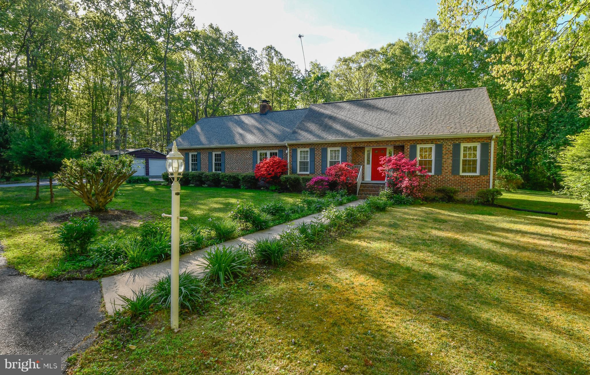 Nestled on 5.26 picturesque acres surrounded by mature trees and beautiful perennial gardens, this classic brick homes offers the perfect blend of privacy, comfort, and country charm.  A sweeping horseshoe driveway welcomes you home, creating a first impression of "Ahhh" as you are welcomed by exquisite beauty.   Step inside to discover a spacious and thoughtfully designed floor plan. The main-level primary bedroom provides convenient one-level living, while the large living room, featuring a charming built-in corner cabinet, and the sun-filled dining room both showcase stunning views. The generous kitchen is designed for both everyday living and entertaining, offering a center island, dedicated coffee bar type area, large pantry, and additional dining space overlooking the backyard through French doors. Step outside to the covered brick patio, an ideal setting for relaxing and enjoying the peaceful surroundings. Just off the kitchen, the family room centers around a beautiful brick hearth with a wood-burning fireplace insert, creating a warm and welcoming gathering space throughout the seasons. Upstairs, you'll find three additional bedrooms, including two with walk-in closets, plus access to an enormous and tall unfinished above garage attic space. This exceptional space offers endless possibilities, whether you envision a home office, studio, hobby space or just want easy walk in space for storage. The unfinished basement is equally impressive adding unlimited potential for future finishing. Convenient stair access from both the kitchen and attached garage adds to the home's functionality. The oversized attached two-car garage features an attractive epoxy-coated floor, while two detached out buildings offer incredible flexibility. One includes its own power source, and the other is currently being used for dry wood storage.  Either would be ideal for workshop space, hobbies, equipment storage, or recreational vehicles.  With over five acres of beautiful natural surroundings, amazing perennials, multiple garage/out buildings, abundant storage, expansion potential, and dependable fast internet, this property offers a rare opportunity to enjoy peaceful country living without sacrificing convenience. As an added bonus, the owner works from home and is including the Starlink equipment, providing excellent internet service.  Properties with this combination of acreage, versatility, and timeless appeal seldom become available.  Back on the market through no fault of the seller!