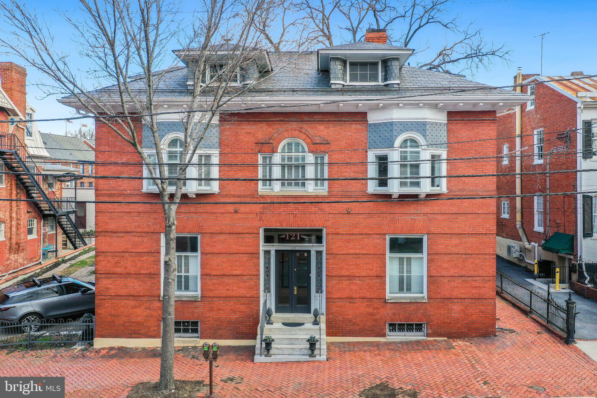 Historic Luxury in the Heart of Downtown Frederick. Located on the coveted west side of the historic district, literally steps from Baker Park and Market Street, 121 W Church Street is an exceptional period residence that seamlessly blends historic charm with custom, designer-level modernization. The result is a harmonious blend of early 20th Century elegance with stunning modern finishes and appointments. This meticulously restored home showcases original architectural details alongside modern luxury upgrades throughout. The home underwent a comprehensive primary renovation featuring a gourmet chef’s kitchen with custom solid wood cabinetry, illuminated glass display cabinets, Cambria quartz countertops, and a dramatic copper-accented design. Premium top of the line appliances include a Wolf six-burner range, Sub-Zero refrigerator, dual-temperature wine cooler, under cabinet ice maker, and a Wolf under-counter drawer microwave. A spacious 9-foot prep island, copper farm sink, custom copper hood, and designer lighting create an ideal space for entertaining and everyday living. The luxurious primary suite offers a spa-inspired retreat with a large glass-enclosed shower featuring Carrara marble, multiple shower heads, quartz benches, and heated marble flooring. The suite also includes custom dual vanities, a soaking tub illuminated by crystal chandeliers, and an expansive walk-in closet with custom cabinetry and elegant lighting. Throughout the home, original heart pine floors have been carefully refinished, while historic elements such as stained glass panels, and restored pocket doors maintain the property's authentic character.
Elegant lighting fixtures, including crystal chandeliers and antique European pieces, enhance the formal living and dining spaces. The living room also features a working gas fireplace. Additional interior improvements include a redesigned family room with built-in cabinetry, a fully remodeled second-floor guest bathroom with marble and designer finishes, a spacious guest room with access to the balcony overlooking the courtyard, and a converted attic space offering flexible office, workout, or guest space along with a convenient second laundry area with new front load washer and dryer. Outdoor living spaces have also been enhanced with a 425-square-foot brick patio in a herringbone pattern, custom brick planters, and a fountain water feature—creating a private and elegant courtyard setting. Exterior upgrades include restored shutters, painted and sealed brickwork, cedar fencing with dual gates. Modern systems have been addressed with new upstairs and downstairs HVAC systems, appliance upgrades, and continued restoration work to preserve the home’s historic integrity. With its blend of historic craftsmanship, high-end finishes, and extensive renovations, 121 W Church Street offers a rare opportunity to own a turnkey historic residence in one of downtown Frederick’s most desirable locations.
