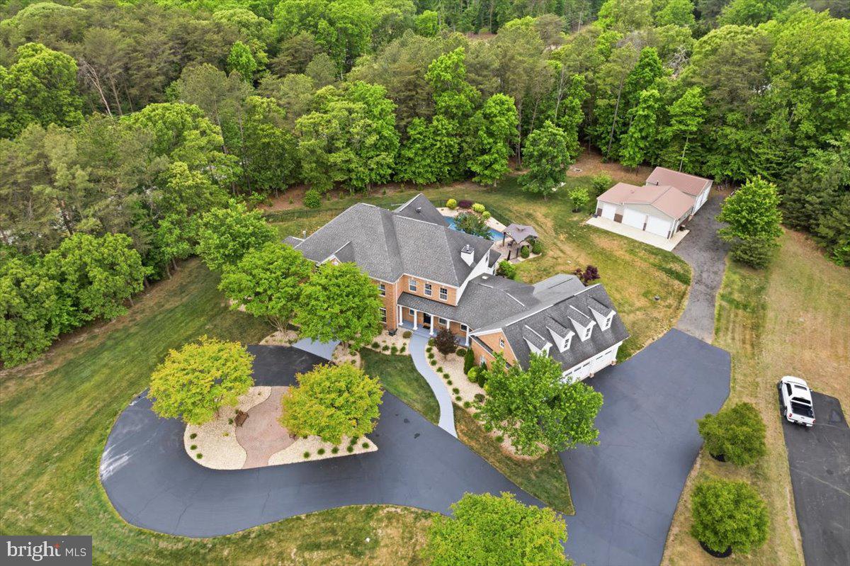 ***$20,000 PAID for Buyers*** Closing costs, interest rate buy-down, price reduction-- YOU CHOOSE! MOVE-IN NOW. Multi-Generational Estate with Resort-Style Backyard + Extensive Workshop/Garage Space on 2 Private Acres. Welcome to this exceptional custom-built 8,600+ SF estate designed for multi-generational living, large-scale entertaining, and luxury everyday comfort in the heart of mid-Calvert County. Perfectly situated on 2 private acres, this one-of-a-kind brick-front home with a 1500+ SF attached garage offers the ideal setup for extended family, in-laws, adult children, live-in care, au pair living, or long-term guests, all with flexible spaces that rarely come available in Southern Maryland. Inside, the thoughtfully designed main level features a private in-law suite/guest wing with a separate entrance and screened porch, creating true independent living potential while still feeling connected to the home. The expansive floorplan includes a large eat-in kitchen, formal dining room, executive office with custom wood accent walls, spacious family room, and a stunning morning room with soaring 12-foot ceilings and marble flooring. Hardwood floors span most of the main level. Upstairs, the luxurious owner’s retreat feels like a private sanctuary with tray ceilings, a fireplace, a coffee bar, and spa-like proportions. Three additional oversized bedrooms and two full baths complete the upper level. The fully finished walk-up lower level was built for entertaining and flexible living, featuring a second full kitchen, media room, billiards area, built-in entertainment space, a fourth fireplace, and a full bath with a tiled shower—ideal for pool access, guest overflow, or private lower-level living arrangements. Step outside into your own private resort. The outdoor living space centers around a stunning 20'x40' heated pool with a tanning shelf, diving board, stone waterfall, and expansive patio spaces designed for unforgettable gatherings. Two oversized pavilions create the ultimate setup for outdoor entertaining, celebrations, cookouts, and summer weekends at home. A separate fenced pet area adds even more convenience. For car enthusiasts, hobbyists, contractors, small business owners, or anyone needing serious storage and workspace, the property also includes two detached outbuildings with four additional garage bays, workshop space, water, electric, and slab foundations. This is more than a home—it’s a rare opportunity to own a private family compound-style estate with luxury amenities, flexible living options, and unmatched entertaining potential. Home warranty conveys. Did we mention the incredibly low utility bills?