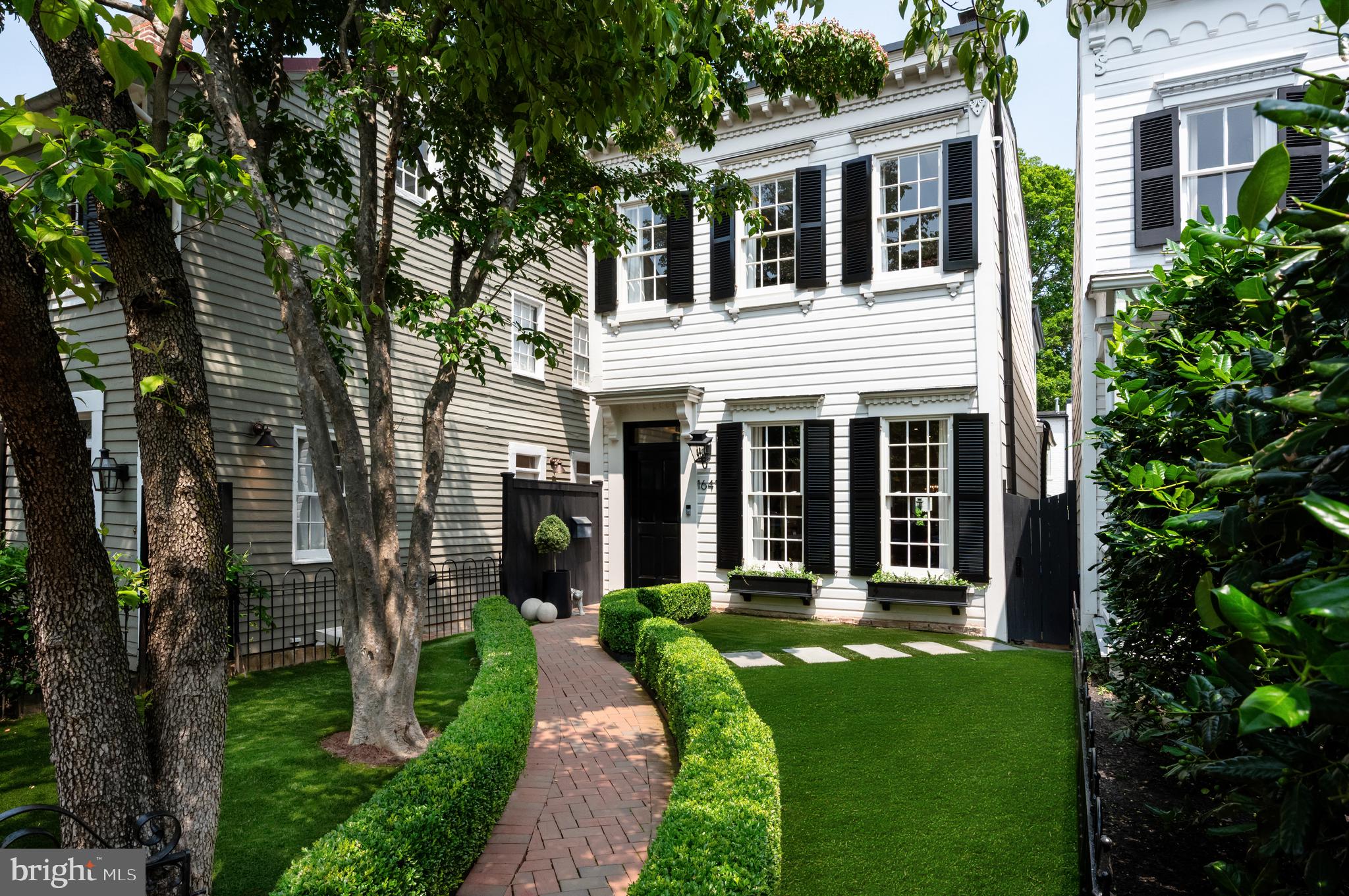 A distinguished residence in Georgetown’s storied West Village, 1641 35th Street NW is a masterwork by Akseizer Residential. Originally constructed at the turn of the century, this elegant, fully detached home underwent a full-scale renovation in 2022, redefining it for modern luxury living.
 
Set back from the street, a newly turfed front lawn is shaded by mature trees, offering privacy and tranquility. A brick paver walkway, flanked by manicured hedges, leads to the classic Colonial façade, where crisp white siding, dark shutters, and intricate trim detailing create a timeless and chic first impression.
 
Inside, refined craftsmanship and elevated design set the tone. Thick, multi-piece crown molding, picture frame millwork, and custom built-ins speak to meticulous attention to detail. The formal living room features floor-to-ceiling shelving surrounding a Calacatta marble fireplace, while ten-foot ceilings, herringbone white oak floors, recessed lighting, integrated surround sound, and contrasting dark accents lend a sense of modern sophistication. Tucked into the corner is a formal powder room with a substantial marble vanity—discreet and stylish.
 
At the heart of the home lies the chef’s kitchen, as beautiful as it is functional. Slab Carrara marble wraps the backsplashes and thick ogee-edge countertops, draping over a generous central island. Inset cabinetry conceals state-of-the-art appliances, including a 48” Wolf range and full-size SubZero refrigeration, as well as a column wine cooler. The adjacent dining area, with its deep coffered ceiling and wall of built-ins, opens through double glass doors to the rear terrace.
 
Outdoors, the flagstone-lined patio is framed by mature landscaping and offers complete privacy. A built-in grill and outdoor entertainment center create an idyllic setting for al fresco dining and entertaining.
 
Upstairs, the primary suite overlooks the front garden and features custom cabinetry, a dressing area, and a spa-like bath with Waterworks fixtures, marble mosaic flooring, double vanity, and a glass-enclosed shower with multiple heads. Two additional spacious bedrooms share a similarly luxurious marble hall bath.
 
The lower level was designed with entertaining in mind, anchored by a full-length family room featuring a wet bar at one end and a media center at the other. A fourth bedroom—currently outfitted as a fitness room—full bath, and fully appointed laundry room complete the level.
 
A rare detached carriage house adds exceptional versatility. The lower level offers a one-car garage with epoxy flooring and an EV charger, while the upper suite includes a full bath, walk-in closet, and a wall of built-ins—ideal for use as a home office or guest quarters.
 
Every inch of this home is immaculately maintained, thoughtfully designed, and flawlessly finished with a fresh, sophisticated touch by acclaimed Edith Gregson Interiors. Positioned on one of Georgetown’s most coveted streets, 1641 35th Street NW represents the pinnacle of elegant city living.
