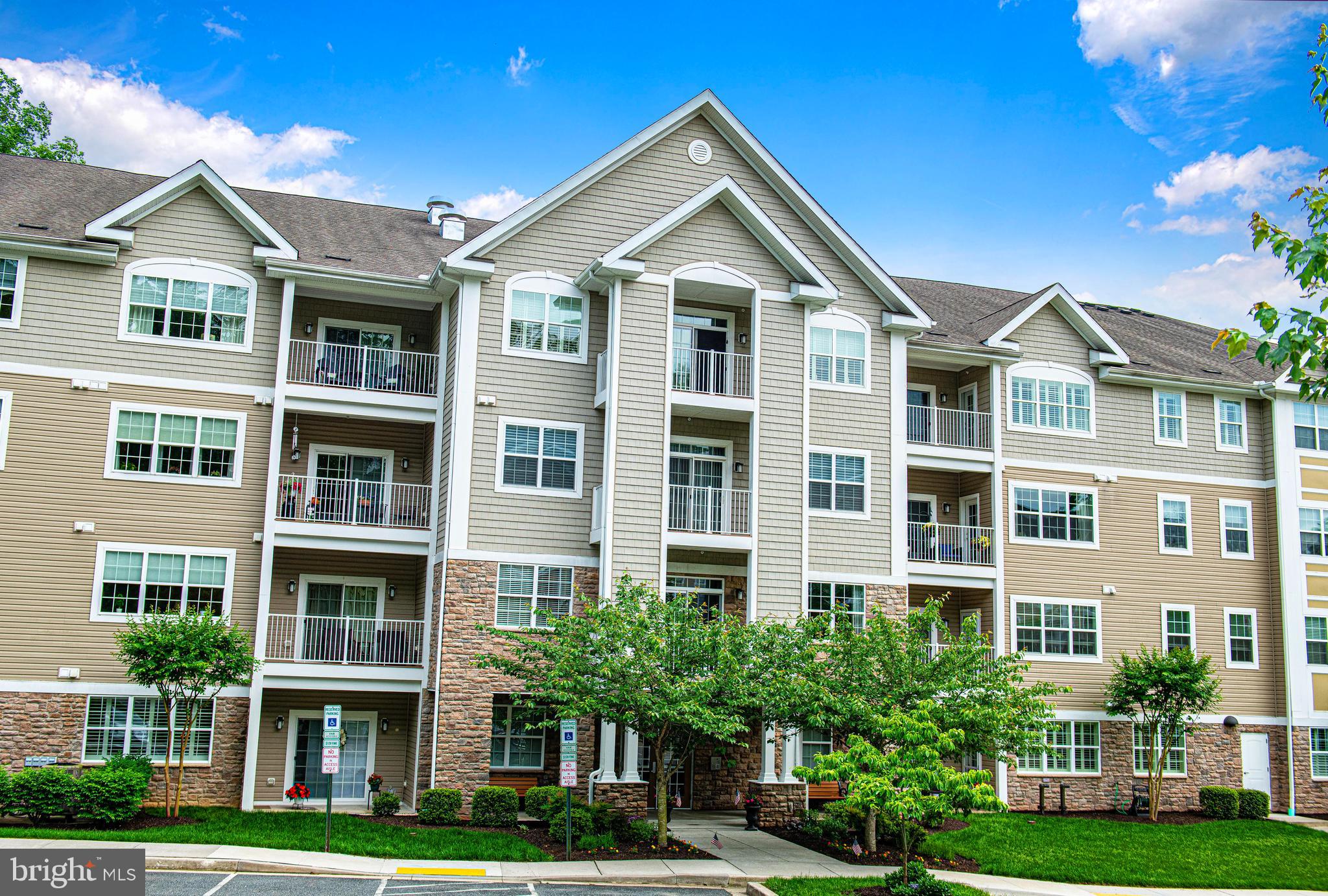 Tucked within the peaceful setting of Overlook at MacPhail Woods, this top-floor condo offers comfort, privacy, and low-maintenance living in a highly desirable 55+ community surrounded by wooded scenery. Located in one of the newer buildings, this mid-hall unit enjoys no direct neighbors on either side, creating an added sense of privacy. Designed with both style and function in mind, the open layout features 9-foot ceilings, crown molding, and abundant natural light that enhances the spacious feel throughout. As you enter, beautiful hardwood flooring extends from the front door through the main living areas, creating warmth and continuity throughout the home. The kitchen offers stainless steel appliances, a granite breakfast bar, pantry storage, 42” cabinetry, and generous prep space. The adjoining family/living room with plantation shutters opens to a private Trex balcony, also accessible from the spacious primary bedroom—perfect for enjoying fresh air or quiet mornings. The primary suite includes two closets, including a walk-in, along with a private bath featuring a double vanity, ceramic tile, grab bars, linen storage, and a walk-in shower with built-in seating. A second bedroom with plantation shutters and a full bath provide flexibility for guests, office space, or hobbies.  Residents enjoy secure building access, elevators, fire safety features, scenic walking trails, social gatherings, a community room with fitness equipment, and the peace of mind of a backup generator supporting key common-area functions. Complete with private storage and lower-level covered garage parking with side entry and remote access, plus two deeded parking spaces (#27 & #27A), this home offers simple, convenient living in a beautiful setting.