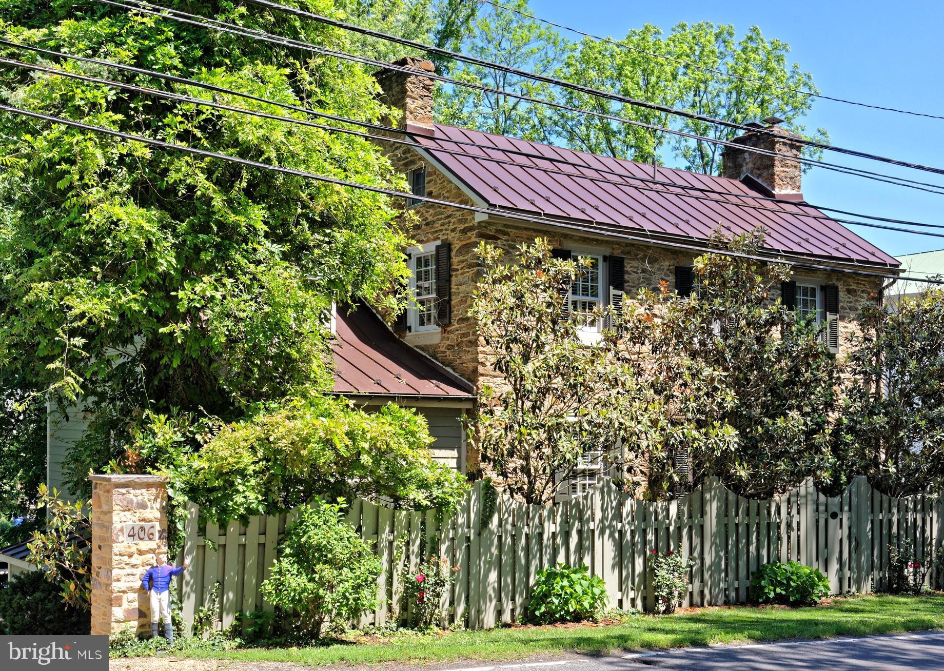 The Jacob Mann House, circa 1817 and once home to Middleburg’s local tanner, is a charming fieldstone residence ideally located on the eastern edge of the historic village. Rich in character and thoughtfully updated, the home offers three bedrooms and two full baths including a main level primary suite. Step inside to find original hardwood floors, two fireplaces, built-ins, custom cabinetry, and abundant natural light throughout. The designer kitchen features high-end appliances and looks out over a bright enclosed back porch overlooking a deck, the private gardens and a swimming pool. The finished walk-out lower level includes a spacious Tavern Room upgraded with exposed beams, custom cabinetry, a gas fireplace, and a mini-split system, along with a private office space and a Butler’s Pantry with more custom cabinetry and an exposed stone wall. Just steps from the main house, the restored Smoke House provides exceptional flexibility with a full bath, heated hardwood floors and a fireplace making it ideal as a guest suite, home office, artist’s studio or workout room. The fully fenced grounds offer rare privacy within town limits and are enhanced by mature landscaping, including more than 50 boxwoods, laurels, arborvitae, hollies, and pines. Other improvements include pool renovations, updated fencing, a tar-based pea gravel driveway, three mini-split systems, a retractable pool cover and a hot tub. Savor the privacy of a secluded in-town setting, while enjoying an easy walk to Middleburg’s shops, restaurants, library, and post office along with quick access to local wineries, breweries, and nearby walking trails through the Salamander Resort. Unique corner parcel on .48 acres fronts three streets and has subdivision potential. A rare opportunity to own a beautifully preserved historic home in Middleburg. Don't miss!
