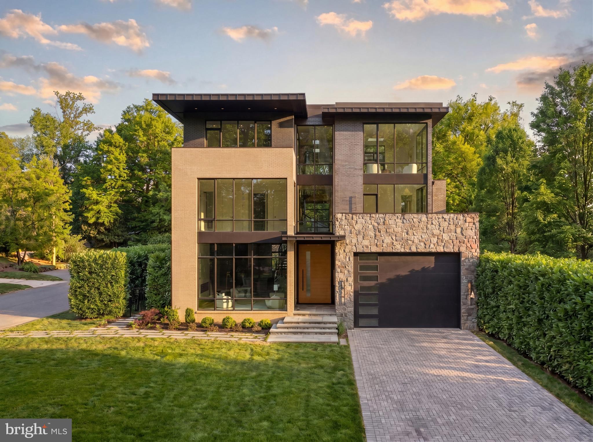 Tucked away on a quiet, wooded street in coveted Chevy Chase DC, 2717 Tennyson Street NW is a newly constructed contemporary residence distinguished by an exceptional connection to its natural surroundings. Immediately bordering the verdant sanctuary of Rock Creek Park, the home captures rare, uninterrupted views of lush greenery, an experience seldom found within the city. Crisp angles, a blend of contrasting materials, and expansive glass area by Kolbe & Kolbe creates a dramatic curb appeal. A custom 11-foot aluminum and wood entry door introduces the grand interior, opening into a gallery-like foyer with through sightlines to the rear terrace and framed by a sweeping staircase. Spanning nearly 10,000 square feet, formal and informal rooms are thoughtfully arranged for both grand-scale entertaining and comfortable daily living. European white oak flooring, installed using a special glue-down method, recessed baseboards, solid-core doors with 1½-inch jambs, and bespoke maple wall paneling create a refined, gallery-like interior and serve as a testament to the attention to detail found in every square inch of the property. Throughout, floor-to-ceiling windows and oversized glass doors frame the verdant canopy of Rock Creek Park, flooding the interiors with natural light and creating a constant dialogue with the outdoors. In the principal living spaces, broad panes of glass transform the surrounding trees into a living backdrop, changing with the seasons. Four Napoleon fireplaces infuse warmth into these spaces. The centerpiece of the residence’s more casual spaces is the striking chef’s kitchen. Equipped with a comprehensive suite of Thermador Professional Series appliances, neatly integrated into fully custom cabinetry and natural stone surfaces imported from Brazil, the space is a poster child for streamlined luxury. Adjacent living and dining spaces flow seamlessly outward to terraces and outdoor entertaining areas, extending the home’s connection to its serene setting. Upstairs, the primary suite serves as a private retreat, complete with a private terrace offering sweeping wooded views, a generous dressing room, and a lavish primary bath clad in Porcelanosa marble, featuring a steam shower room and radiant heated floors. Seven additional bedrooms and ten bathrooms throughout are each outfitted with exotic stonework and Delta fixtures, offering ample accommodation. The home is a hub for thoughtfully integrated wellness and recreation amenities. A dedicated fitness center with professional rubber flooring is supported by a sauna and promotes a wellness-oriented lifestyle, while a climate-controlled wine cellar with 200-bottle capacity adds a refined entertaining element. Mechanical systems supporting the property promote energy efficiency, including four-zone Carrier high performance HVAC controlled by Nest smart thermostats, a garden roof, EV charging station, and permeable driveway and patios. The outdoor space is another showstopper. The highlight of which is an expansive 40-by-20-foot lap pool with integrated spa anchoring the rear grounds to create a private resort-like setting. Above, a rooftop terrace prepared for an outdoor kitchen and grilling station offers elevated entertaining space and unbroken vistas. With its striking architecture, painstaking attention to detail and unparalleled location, 2717 Tennyson Street NW is a refreshingly sophisticated modern residence representing a forward-looking ideology into the notion of luxury urban living.