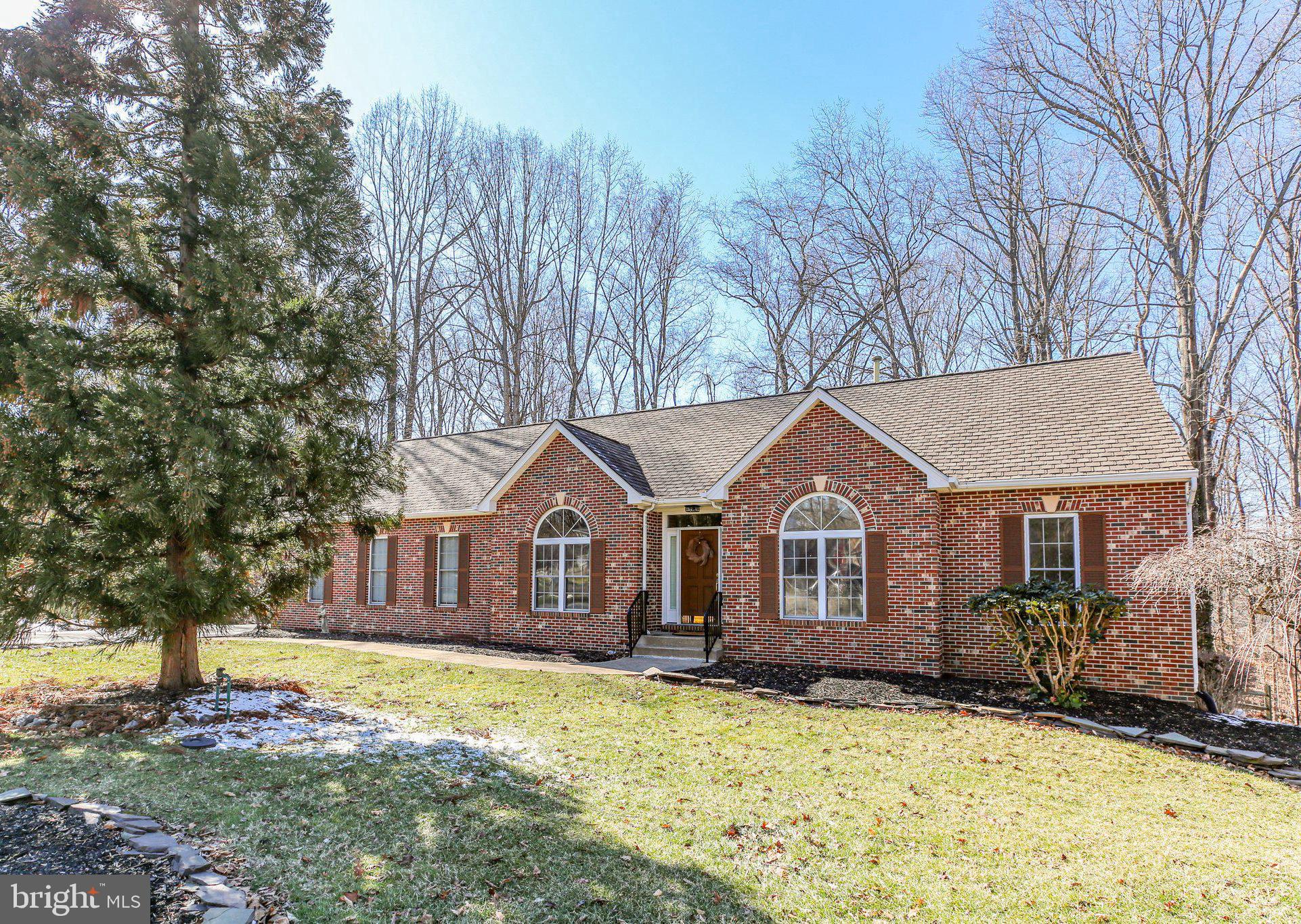 Nestled at the end of a quiet cul-de-sac in the desirable Lee’s Hill South community, this gracious brick home on Ramsay Court offers a perfect blend of elegance, warmth, and functionality. Surrounded by mature trees, the setting provides a peaceful retreat while maintaining close proximity to modern conveniences.  As you step inside, the welcoming foyer leads to a formal living room on the right, where a two-sided fireplace and a large, sunlit window create a cozy and inviting atmosphere. This space could also serve as a perfect home office. On the left, the formal dining room is well-suited for entertaining, offering plenty of space for gatherings. Moving beyond the foyer, the spacious family room features large windows that frame picturesque wooded views, while the two-sided fireplace adds charm and warmth, making it an ideal spot to relax on cool evenings.  Brand new carpet has been installed throughout the main level. To the right of the family room, two generously sized bedrooms share a bright hall bathroom with transom windows and classic white ceramic tile accents. On the opposite side of the family room, the casual dining area boasts ceramic flooring and ample windows, creating a cheerful space for everyday meals. 
At the heart of the home, the kitchen and breakfast area are designed for both functionality and socializing, offering abundant space for guests to gather. The kitchen has been freshly painted and features gleaming cherry cabinets and granite counters with custom backsplash. A seamless flow into the formal dining room and breakfast nook enhances the open feel, while a door leads to a Williamsburg-style screened porch with charming Chippendale design accents, providing a serene, tree-top view.  
The primary suite, located on the left wing, is a true retreat. Spacious enough for a large bed and additional furnishings, it even allows for a private sitting area. A generous walk-in closet ensures ample storage, while the en-suite bath features dual vanities, a soaking tub, a remodeled walk-in shower, and a linen closet—all complemented by a large corner window that invites natural light. Just down the hall, a sizable laundry room provides extra storage and convenience.  If privacy is a concern, this home is ideally located without view of your neighbors. Downstairs, the home reveals even more space to enjoy. The lower level includes a spacious library or second home office with built-in bookshelves, French doors that open to the backyard, and new carpet. A vast recreation room, complete with sliding glass doors leading to a covered patio, offers an excellent space for entertaining, with shelter from the screened porch above. At the far end of this level, a comfortable guest bedroom and a full bath provide a private retreat for visitors. The unfinished portion of the basement serves as a valuable utility and storage space, featuring built-in shelving, ample electrical outlets, and even a refrigerator and 14 cubic ft. steel vault that convey with the home.  The oversized side-load garage is thoughtfully designed with additional storage & workspace, including a dedicated area for gardening tools or a potting station. A built-in wooden ramp enhances accessibility & makes moving in a breeze, though it can easily be removed if desired.  Lawn sprinkler system box is located in the garage, too. Step outside & explore the beautifully wooded grounds, where nature surrounds you in every direction.  Residents of Lee’s Hill South enjoy fantastic community amenities, including a nearby pool, tot lots, and basketball courts, while golf enthusiasts will appreciate the Lee’s Hill Golf Club just down the road, with memberships available to new homeowners. Conveniently located near I-95, hospitals, shopping, and historic Fredericksburg, this home is perfectly positioned for both relaxation and convenience. With its thoughtful layout, abundant space, and timeless appeal, this property is ready to welcome you home.