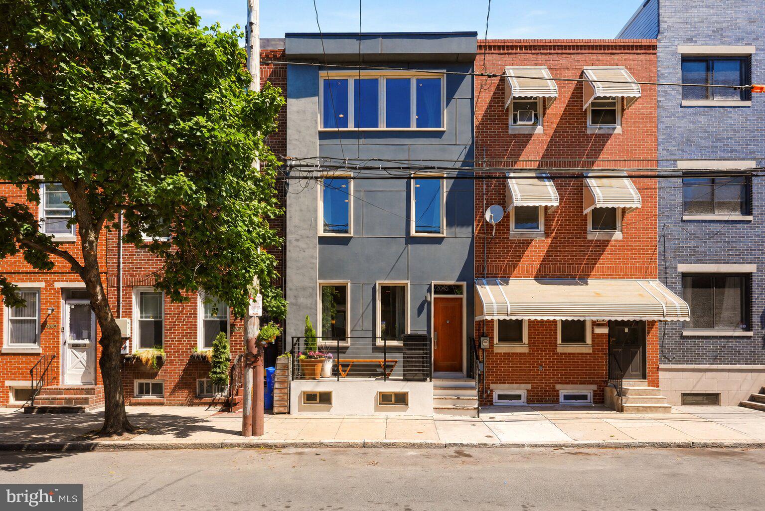 2045 Federal Street isn’t just a home — it’s a front-row seat to one of Point Breeze’s most connected and welcoming blocks. Neighbors know each other here. Annual block parties, packed Halloween nights, morning coffee conversations on the stoop — this is the kind of Philadelphia street people hope to find and rarely do.

And the stoop itself sets the tone immediately: one of the largest on the block, offering a true extension of the living space. Start the day with coffee as the neighborhood wakes up around you, or unwind in the evening under the glow of the streetlight just outside, keeping the block warm, inviting, and beautifully lit after dark.

Inside, the home opens up in a way that immediately feels different — expansive sightlines, oversized rooms, and a layout designed for both entertaining and everyday comfort. Rich hardwood floors, recessed lighting, warm wood tones, and sleek industrial railings create a modern aesthetic that still feels grounded, cozy, and inviting. The open-concept living and dining spaces flow effortlessly into the kitchen, where dark espresso cabinetry, granite countertops, pendant lighting, stainless steel appliances, and a large island with seating create a natural gathering space filled with light from the rear patio doors.

Out back, the private patio offers a completely different atmosphere — quiet, tucked away, and ideal for entertaining. Just steps from the kitchen, it creates seamless indoor-outdoor living for summer dinners, weekend gatherings, or a peaceful escape from the city buzz.

The second floor features two generously sized bedrooms with abundant closet space and oversized windows that pour in natural light, along with a full hallway bathroom and a conveniently located laundry closet that makes daily living easy and efficient. The entire third floor is dedicated to the primary suite — a true retreat featuring soaring ceilings, a spa-inspired en-suite bath with large-format porcelain tile, floating double vanity, soaking tub beneath the window, and an open walk-in shower with pebble stone flooring.

The finished basement adds even more versatility with ample space for a media room, gym, office, or guest area, plus a convenient half bath and an additional storage closet tucked neatly beneath the stairs.

The home has also been thoughtfully upgraded throughout the years, including new HVAC and mini-split systems, Pella windows with near hurricane-grade sound dampening on the first floor, James Hardie front facade, fresh paint, updated bathroom flooring, and a fully renovated basement — giving the next owner the benefit of extensive improvements without the projects.

And beyond the home itself, the location continues to rise. Point Breeze and the west side of Washington Avenue are in the midst of an exciting transformation, bringing new energy, restaurants, and development to the neighborhood while preserving the authentic community feel that makes this block so special. Chew Playground, Aldi, CVS, Dock Street Brewery, Ringo’s, and American Sardine Bar are all just moments away — making everyday life walkable, connected, and effortlessly convenient.