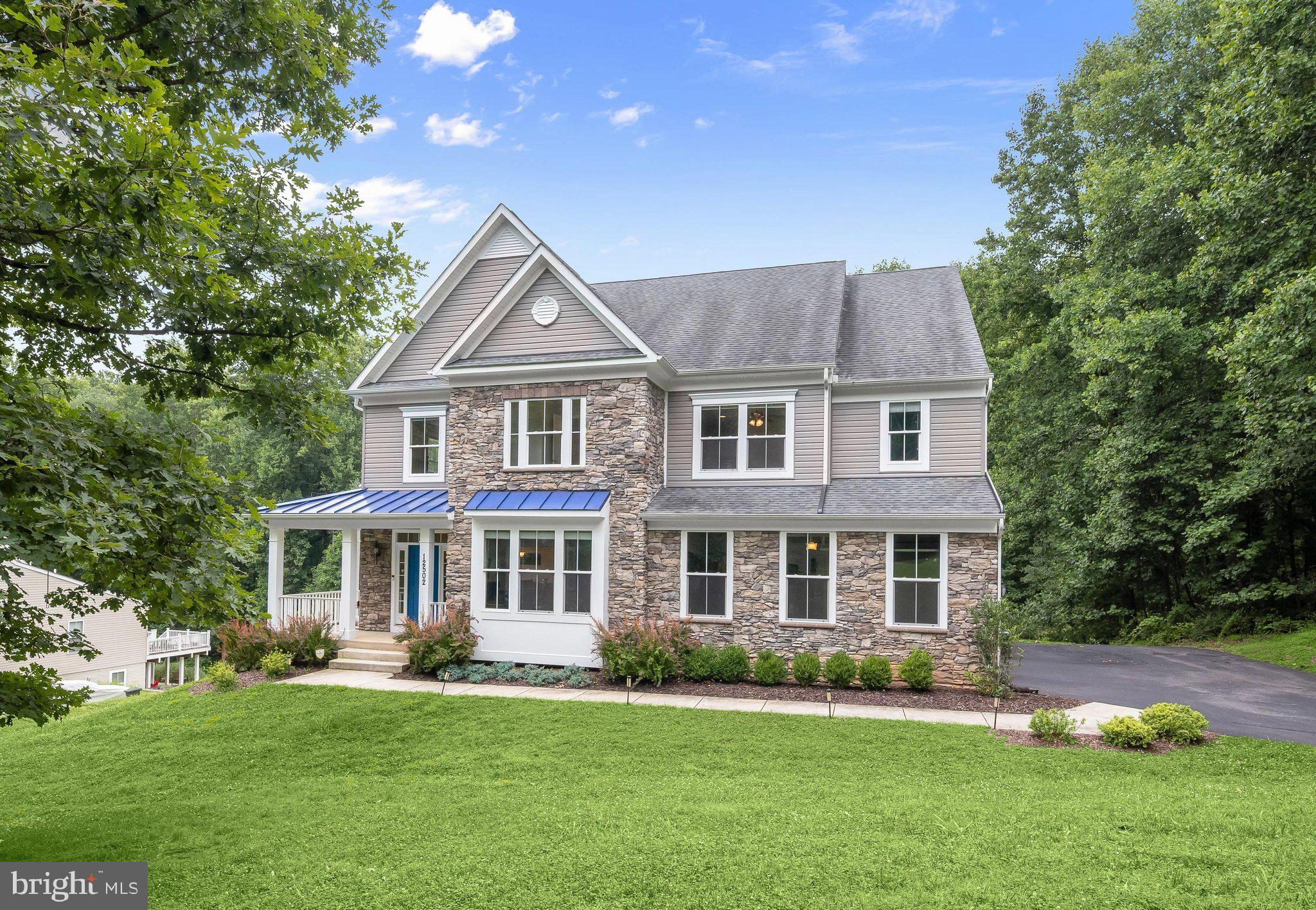 Gracefully positioned on 1.16 picturesque acres along a tree lined road, this exceptional stone accented colonial offers the peaceful feel of a private retreat while remaining just minutes from everyday conveniences. Backing to conservation land and encompassing more than 6,000 square feet across three finished levels, the home has been thoughtfully designed with six bedrooms, 5.5 baths, abundant storage, and flexible living spaces to accommodate a variety of lifestyles.
A charming wraparound covered front porch framed by beautiful landscaping creates a warm and inviting first impression. Inside, an open floor plan showcases hardwood flooring throughout much of the home, a neutral paint color that flows throughout, and light-filled living spaces designed for both everyday comfort and entertaining. The impressive great room is the heart of the home, highlighted by a soaring two story ceiling and a stunning floor to ceiling stone fireplace.
Flowing seamlessly from the great room, the gourmet kitchen combines timeless style with exceptional functionality. White cabinetry, quartz countertops, stainless steel appliances including a gas cooktop, double wall ovens, and two dishwashers are complemented by a pantry and a large center island with seating, creating the perfect gathering space. The adjoining breakfast room captures tranquil wooded views and opens to the composite deck through a sliding glass door, offering an effortless connection to outdoor living. Crown molding enhances the formal dining room, while French doors lead into a dedicated home office ideal for working remotely. A mud room with optional laundry hookups and a half bath complete the main level living areas.
Offering remarkable flexibility, the main level suite is perfectly suited as either a luxurious primary bedroom or private guest retreat. This spacious sanctuary includes a walk-in closet, a sitting room with direct deck access, and an elegant en-suite bath featuring a double vanity, soaking tub, and frameless glass shower finished in timeless subway tile.
Upstairs, each of the four bedrooms enjoys direct access to a full bath, providing both privacy and convenience. The expansive primary suite features a tray ceiling, an oversized walk-in closet, and a spa-inspired bath with heated floors, an extended double vanity, soaking tub, and beautifully tiled shower. Two additional bedrooms share a thoughtfully designed bath with a separate water closet, while another bedroom enjoys the privacy of its own en-suite. A conveniently located laundry room completes the upper level.
The finished walkout lower level offers outstanding versatility with a spacious recreation room, kitchenette featuring quartz countertops, stainless steel appliances, and bar seating, a sixth bedroom, full bath, storage and utility rooms, making it an excellent option for an in-law suite, apartment, or extended guest accommodations.
Surrounded by peaceful wooded views, the outdoor living spaces are equally inviting with a composite deck, paver patio, and a built-in shed tucked beneath the deck. Additional highlights include a finished side loading two car garage, widened and extended driveway, recently painted exterior, active radon mitigation system, extensive closet space with added shelving throughout, and exceptional storage at every turn.
Perfectly situated on Triadelphia Road, this home enjoys convenient access to Turf Valley Towne Square, The Mall in Columbia, Historic Ellicott City, Patapsco Valley State Park, Centennial Park, golf courses, highly regarded Howard County public schools, and major commuter routes including Route 29, I-70, Route 40, and MD-100, providing easy access to Columbia, Baltimore, Washington, D.C., and BWI Airport.