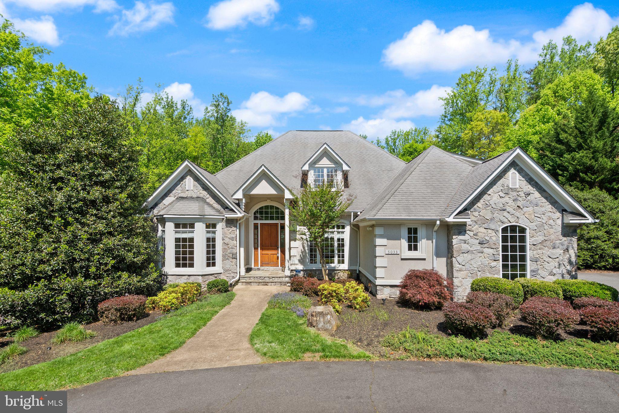 Set on 5 private wooded acres in a prime Fairfax location, this custom-built 5-bedroom, 5.5-bath French Country estate delivers the space, privacy, and resort-style living that rarely come to market, all just minutes from major commuter routes and everyday conveniences. From the moment you arrive, the circular driveway, stately stone and stucco exterior (DryVit system), and 3-car side-loading garage create a strong sense of arrival and set the tone for what’s inside.

Step through a tall wood entry door into a dramatic two-story foyer, where hardwood floors, a sweeping staircase, and natural light immediately highlight the home’s scale and craftsmanship. Designed with both everyday living and entertaining in mind, the main level offers a seamless flow between formal and casual spaces, including a office with bay window, and a spacious living room anchored by a stone fireplace and a wall of windows overlooking the property.

The gourmet kitchen is built to perform and impress, featuring granite countertops, a tumbled marble backsplash, cherry cabinetry, high-end stainless steel appliances, a gas cooktop with vented hood, wine chiller, and a large walk-in pantry. It opens directly to the dining area and outdoor living spaces, making it ideal for hosting at any scale.

A true highlight for today’s buyers, the main-level owner’s suite offers both convenience and privacy, complete with a sitting area, private balcony, custom walk-in closet with washer/dryer hookup, and a spa-style bath with dual vanities, jetted tub, and an oversized walk-in shower.

Upstairs, four generously sized bedrooms provide flexibility for guests, or work-from-home needs, each with access to private or dual-entry baths, along with a bright upper-level laundry room.

The fully finished walkout lower level expands the home’s versatility with high ceilings, bamboo hardwood flooring, multiple recreation spaces, a game room, kitchenette, full bath, and a dedicated bonus/hobby room, making it ideal for entertaining or multigenerational living.

Outside is where this property truly separates itself. A custom natural stone patio surrounds a pool featuring a diving board, slide, waterfall, and all set against a backdrop of mature trees and open lawn, creating a private, resort-style setting that’s difficult to replicate in Northern Virginia.

While the setting feels completely private, the location keeps you connected, with quick access to Braddock Road, Fairfax County Parkway, Routes 29 and 50, and I-66. Fairfax Corner, Fair Oaks Mall, and the Mosaic District are all within easy reach, along with George Mason University and a wide range of dining, shopping, and entertainment options.

A rare opportunity to own acreage, a custom build, and a resort-style outdoor experience in one of Fairfax County’s most convenient locations. Schedule your showing today!