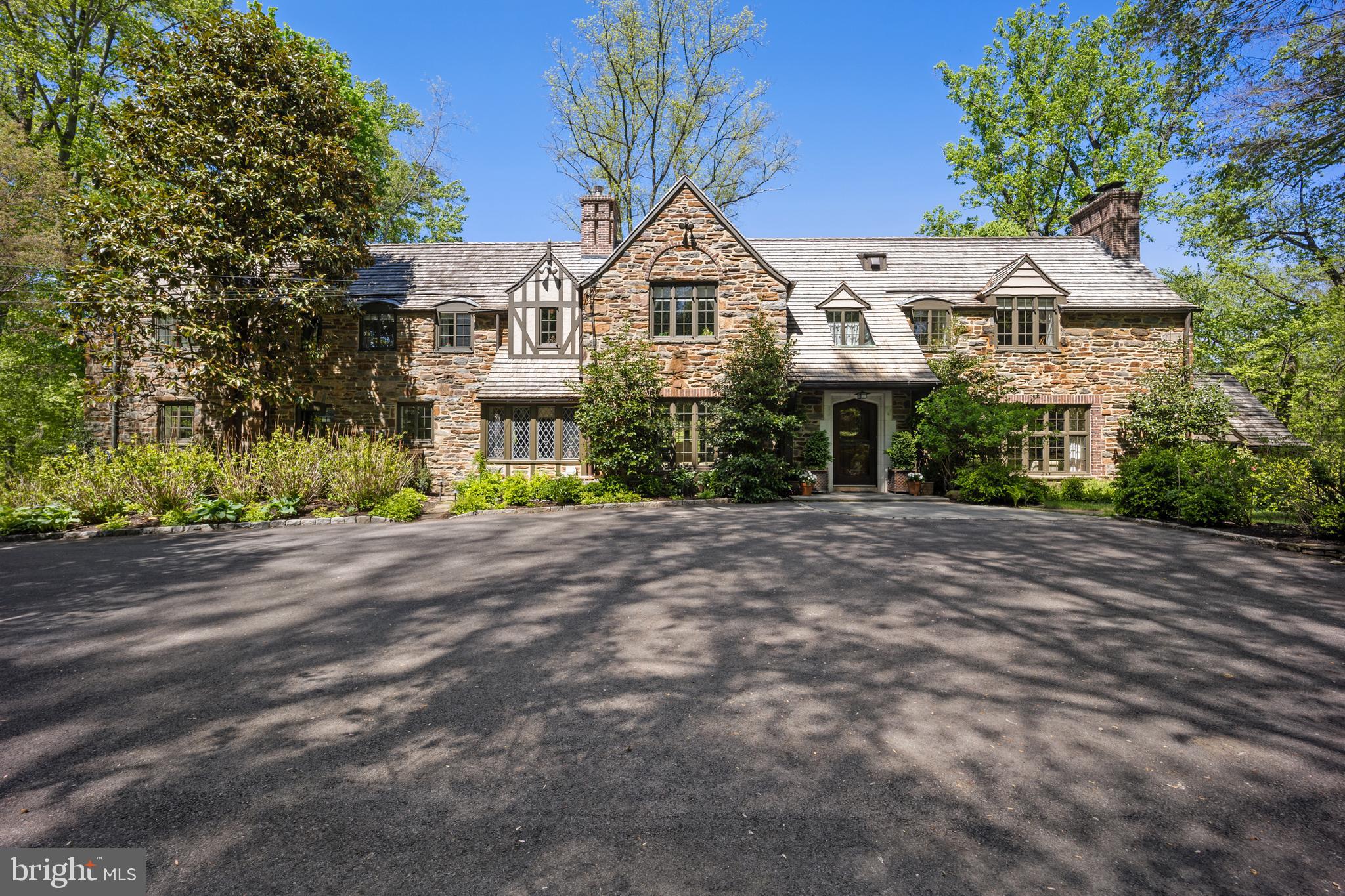 On the Main Line, homes of this caliber are measured not only by the sweep of the land and square footage of the home, but also by the discipline of its stewards—knowing what to improve and knowing what to preserve.   Set on 2.25 lush acres of park-like grounds, this spectacular “Legacy Estate” is precisely the kind of storied property the Main Line is known for — a private sanctuary where modern comfort has been woven in with a thoughtful hand, but the soul of the home was never compromised.  As you approach the property, slow your pace and admire the scene.  Set back from the road, the stone home sits high above a sweeping park-like lawn framed by privacy landscaping, accented by a charming bridge that arcs over a quiet curve of Mill Creek.   The driveway offers both a circular turnaround and plentiful parking, perfect for everyday convenience and effortless entertaining.  Step through the arched entry into a foyer anchored by a dramatic curved staircase, soaring ceilings with period moldings, and gleaming hardwood floors. To the right, the formal living room is lined with windows and centered on a wood-burning fireplace with new liner and firebox. Beyond, a library with cathedral beamed ceiling, fireplace, hidden bar, and access to the side patios offers one of the home's most inviting retreats. To the left of the foyer, the generously sized dining room features linen wall coverings and French doors opening to a slate patio — equally suited to outdoor parties or morning coffee. Adjacent, a breakfast room with lead-glass windows, beamed ceiling, and slate floor is outfitted with a custom built-in butler's pantry with lighted bar. The Chef's Kitchen delivers both luxury and function: a Lacanche range, Wolf steam oven, oversized island, statuary marble countertops, and generous cabinetry. Beyond, the original staff wing provides two bedrooms, a full marble bath with radiant heat floors, and access to both levels via the back staircase. Upstairs, the primary suite features a vaulted ceiling, gas fireplace, and balcony overlooking the grounds. The primary bath offers a soaking tub, oversized shower, double vanity, marble tile, radiant heat floors, and heated towel racks. Three additional bedrooms are served by two Jack-and-Jill baths, both with radiant heat floors. A hallway laundry room and attic storage complete the upper level. As you decend to lower level, you will find a landing with powder room and door to a patio. Below is the finished lower level-- a destination of its own.   A large Recreation Room with fireplace has French doors that open to another slate patio.  A redlight sauna, wet bar, powder room and exercise area, all with radiant heat flooring, provide a spa-like setting while the Wine Cellar with 2 zoned refrigeration will accommodate a collection of up to 2500 bottles!  A utility room houses 2 new water heaters, new HVAC servicing the basement and 1st floor, the security panel and laundry hookup.   A mudroom with boot wall and lockers is conveniently located next to the garage. The two-car garage with new doors houses a reverse osmosis water system, whole-house water softener/chlorine removal system, and EV charging station. Additional improvements to the home include a Generac generator, refurbished windows, two 200-amp electrical panels, heated gutters, a cedar shake roof, irrigation system, and an elevation certificate providing the property with minimal flood insurance.  Walking distance to Rosemont train station, downtown Bryn Mawr and Ashbridge Park, with walking trails, sport courts and playground.  Top-rated schools, and the Main Line's best dining and shopping. A full list of updates is available upon request.