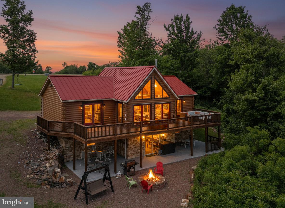 Wake up to panoramic mountain views that stretch for miles — framed through walls of windows in an authentic White Pine log home, set on 12.86 private acres above the Deep Creek Lake region.
 Located minutes from Deep Creek Lake, Maryland's largest freshwater lake, this property delivers the full four-season mountain lifestyle — from summer boating and hiking to winter skiing at Wisp Resort.
With only the cove, spans of pastures, and mountains, as far as the eye can see, it is perfect for an everyday escape to relax and recharge by the fire table.  Or, spanning the width of the home, directly above the patio, it is fashioned for entertaining family and friends.   The twenty-foot vaulted ceilings and exposed beams frame the enormous great room, capturing panoramic mountain views through the floor-to-ceiling windows. Flanking the great room are a full bath and three spacious bedrooms, one of which is an en suite and boasts a sliding glass door to the deck and vaulted ceiling.  Two bedrooms and the great room have open lofts. The kitchen is equipped with top-of-the-line appliances, including a microwave that can also air fry, bake, grill, and more. The finished walk-out lower level adds a second great room, two additional bedrooms, an extra-large full bathroom, a complete kitchen, a laundry room, and a pantry, all with glass sliding doors leading to the concrete patio.
This family- friendly home can be considered multi-purpose in its ability to provide a respite from everyday living, whether it is used as a vacation home or permanent home. For those interested in a second home, there is a turn-key option. What could be better than having a vacation home that could also provide a premier vacation rental income? With no HOA or restrictions, you can do that! The patio is pre-wired and ready for a hot tub, the stone fire pit and chairs are ready, an open field for football, volleyball, etc., awaits a party, and a large pole building to store a boat, motorhome, and all other recreational equipment, making this property the complete package.
This is more than a home; it is a front-row seat to the mountains in every season.