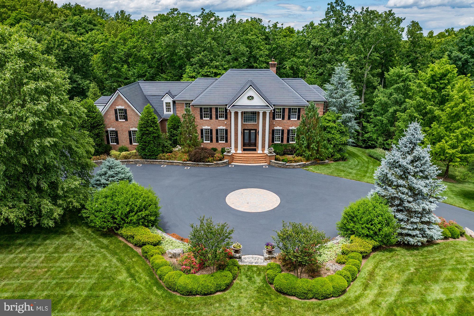 This custom-built estate in the prestigious Courtland Rural Village community is gracefully sited on nearly 20 wooded acres with frontage along scenic Goose Creek. Built by renowned Creighton Enterprises, this secluded manor estate offers over 7,600 square feet of refined living space, combining timeless architecture, modern technology, and extraordinary privacy in one of Loudoun County's most exclusive conservation communities.

Beyond a custom wrought-iron security gate, a sweeping drive winds through professionally landscaped grounds before arriving at the residence, creating a memorable approach befitting a private country estate. A grand circular carriage sweep, extensive hardscaping, and mature woodland surroundings establish a dramatic sense of arrival, while the property's frontage on Goose Creek and neighboring conservation land provide an incomparable natural setting, just minutes from Leesburg's shops, restaurants, wineries, and commuter routes.

Inside, thoughtfully designed living spaces blend sophistication and functionality. Formal and informal gathering areas are anchored by multiple fireplaces, expansive windows framing park-like views, and finely crafted architectural details throughout. The gourmet kitchen is designed for both everyday living and elegant entertaining, featuring an induction cooktop with motorized pop-up ventilation, dual dishwashers, generous storage, and two pantries.

Occupying its own private wing, the luxurious primary suite offers a true retreat within the home. The thoughtfully designed space features a raised sleeping area, fireplace, sitting room, and private balcony overlooking the property's serene wooded surroundings. The dedicated dressing room with a granite-topped double vanity leads to a spa-inspired bath with a freestanding soaking tub and oversized frameless glass shower. Two custom walk-in closets provide exceptional storage and organization. Each secondary bedroom is generously proportioned and complemented by a spacious closet and private en suite bath, creating a comfortable and refined experience for family and guests.

The walk-out lower level is designed as an entertainer's retreat, featuring a custom bar with dishwasher, wine cooler, and microwave, spacious recreation areas, a guest suite, and direct access to the covered patio and outdoor living spaces.

The expansive deck, covered patio, and outdoor kitchen provide seamless indoor-outdoor entertaining opportunities while overlooking the property's picturesque wooded landscape.

Modern infrastructure and efficiency enhancements elevate the home well beyond typical luxury offerings. Highlights include a Tesla Solar Roof, two Tesla Powerwall 3 battery systems with six expansion packs, a permanently installed backup generator, whole-house spray foam attic insulation, three-zone HVAC with smartphone controls, whole-house water filtration and softening systems, and a comprehensive Vivint security and surveillance system. Additional conveniences include upper and lower-level laundry facilities, a 16-zone irrigation system, invisible fencing, and a three-car side-load garage complemented by extensive guest parking.

Rarely does a property offer this level of privacy, natural beauty, architectural presence, and modern efficiency in a location so convenient to downtown Leesburg, Dulles Airport, and Northern Virginia's renowned wine country.