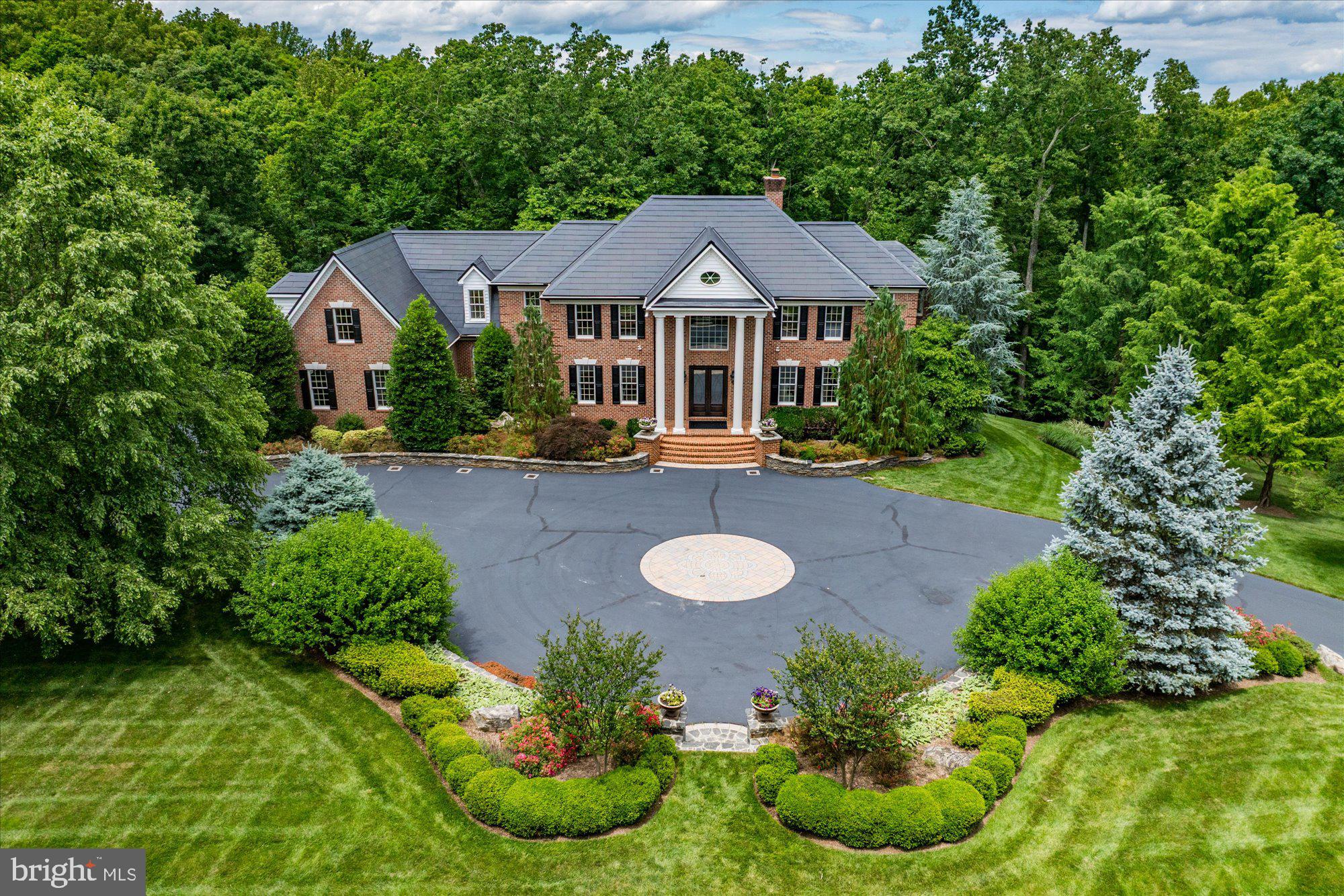 This custom-built estate in the prestigious Courtland Rural Village community is gracefully sited on nearly 20 wooded acres with frontage along scenic Goose Creek. Built by renowned Creighton Enterprises, this secluded manor estate offers over 7,600 square feet of refined living space, combining timeless architecture, modern technology, and extraordinary privacy in one of Loudoun County's most exclusive conservation communities.

Beyond a custom wrought-iron security gate, a sweeping drive winds through professionally landscaped grounds before arriving at the residence, creating a memorable approach befitting a private country estate. A grand circular carriage sweep, extensive hardscaping, and mature woodland surroundings establish a dramatic sense of arrival, while the property's frontage on Goose Creek and neighboring conservation land provide an incomparable natural setting, just minutes from Leesburg's shops, restaurants, wineries, and commuter routes.

Inside, thoughtfully designed living spaces blend sophistication and functionality. Formal and informal gathering areas are anchored by multiple fireplaces, expansive windows framing park-like views, and finely crafted architectural details throughout. The gourmet kitchen is designed for both everyday living and elegant entertaining, featuring an induction cooktop with motorized pop-up ventilation, dual dishwashers, generous storage, and two pantries.

Occupying its own private wing, the luxurious primary suite offers a true retreat within the home. The thoughtfully designed space features a raised sleeping area, fireplace, sitting room, and private balcony overlooking the property's serene wooded surroundings. The dedicated dressing room with a granite-topped double vanity leads to a spa-inspired bath with a freestanding soaking tub and oversized frameless glass shower. Two custom walk-in closets provide exceptional storage and organization. Each secondary bedroom is generously proportioned and complemented by a spacious closet and private en suite bath, creating a comfortable and refined experience for family and guests.

The walk-out lower level is designed as an entertainer's retreat, featuring a custom bar with dishwasher, wine cooler, and microwave, spacious recreation areas, a guest suite, and direct access to the covered patio and outdoor living spaces.

The expansive deck, covered patio, and outdoor kitchen provide seamless indoor-outdoor entertaining opportunities while overlooking the property's picturesque wooded landscape.

Modern infrastructure and efficiency enhancements elevate the home well beyond typical luxury offerings. Highlights include a Tesla Solar Roof, two Tesla Powerwall 3 battery systems with six expansion packs, a permanently installed backup generator, whole-house spray foam attic insulation, three-zone HVAC with smartphone controls, whole-house water filtration and softening systems, and a comprehensive Vivint security and surveillance system. Additional conveniences include upper and lower-level laundry facilities, a 16-zone irrigation system, invisible fencing, and a three-car side-load garage complemented by extensive guest parking.

Rarely does a property offer this level of privacy, natural beauty, architectural presence, and modern efficiency in a location so convenient to downtown Leesburg, Dulles Airport, and Northern Virginia's renowned wine country.