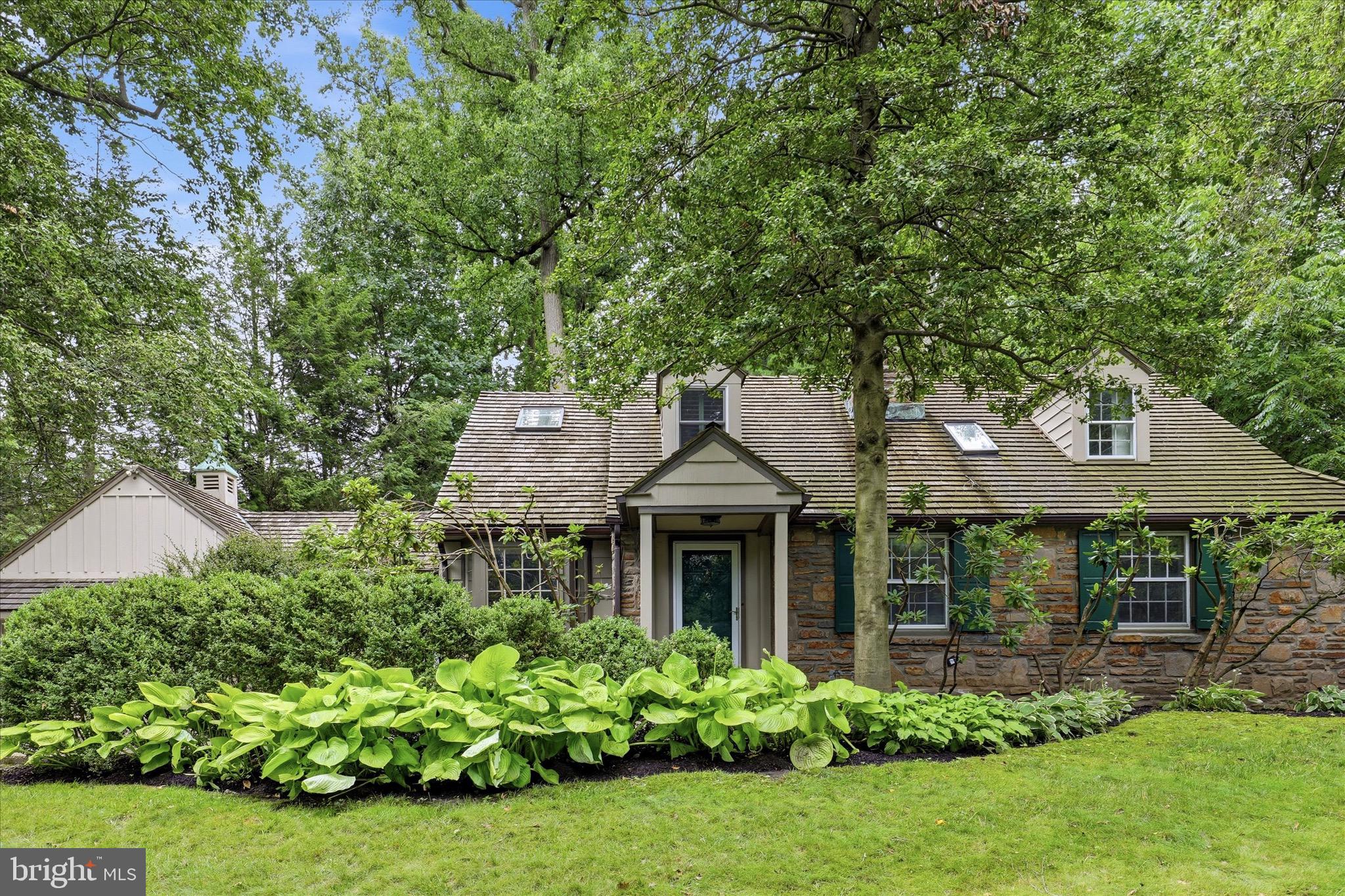 Welcome to 816 Old Gulph Road, where timeless craftsmanship, custom design, and beautifully curated indoor-outdoor living come together in the heart of Bryn Mawr.
Set among mature trees and professionally landscaped grounds, this distinctive Main Line residence offers exceptional privacy, character, and quality throughout. From the moment you arrive, the home’s classic architecture, stone façade, attached garage, and lush garden setting create a warm and memorable first impression.
Inside, the home showcases remarkable attention to detail with custom millwork, elegant moldings, hardwood flooring, recessed lighting throughout the first floor, and wiring for surround sound that extends from the interior living spaces to the stone patio. The gracious living room is anchored by a gas fireplace and framed by custom built-in bookcases, creating a sophisticated yet comfortable space for gathering, reading, or entertaining. Oversized windows bring in abundant natural light and frame beautiful views of the surrounding landscape.
The formal dining room offers an elegant setting for hosting and features chair rail detail, rich trim, recessed lighting, and French doors that open directly to the stone patio, allowing for effortless indoor-outdoor entertaining. The gourmet kitchen is thoughtfully designed with custom contemporary cabinetry, premium integrated stainless-steel appliances, a paneled built-in dishwasher, subzero refrigerator, self-cleaning double convection oven, a range hood, custom five-burner gas cooktop, extensive storage, and a bright breakfast area with direct access to the gardens and patio.
The first floor offers excellent flexibility with two spacious bedrooms. One bedroom remains a comfortable main-level bedroom with dual closets, while the second has been converted into a warm and inviting den with chair rail molding, built-in sound, and French doors leading outdoors—ideal as a home office, library, sitting room, or guest space. A luxurious full bath completes the main level, finished floor-to-ceiling in limestone and featuring custom cabinetry, a Jacuzzi tub, steam shower, glass enclosure, built-in niches, and spa-inspired finishes.
Upstairs, natural light pours through a skylight above the staircase, leading to a private owner's retreat. The spacious primary bedroom offers generous proportions, room for a sitting area or workspace, multiple windows, skylights, a ceiling fan, and peaceful views of the surrounding trees. Originally designed with a fourth bedroom, the upper level has been thoughtfully reimagined to create an expansive custom dressing room with extensive built-in wardrobe systems, open shelving, drawers, hanging storage, shoe storage, and dedicated organization throughout. The ensuite bath is beautifully appointed with premium finishes, a custom double vanity topped with rich green marble, and a steam shower, creating a private spa-like sanctuary.
The lower level adds exceptional functionality with two wine cellars, a dedicated storage room, a laundry area with utility sink, and convenient exterior access.
The outdoor spaces are a true highlight of the property. Professionally designed landscaping surrounds the home with mature specimen trees, hydrangeas, perennial gardens, layered planting beds, stone walkways, and private garden views from nearly every room. The stone patio is wired for outdoor speakers and offers a wonderful setting for dining, entertaining, or quiet relaxation. Dedicated tomato and herb gardens add charm and practicality, while stone steps lead to an elevated upper lawn bordered by mature trees, creating additional space to relax, garden, or simply enjoy the peaceful setting.
Combining timeless architecture, luxurious finishes, custom storage, flexible living spaces, and beautifully designed grounds, 816 Old Gulph Road presents a rare opportunity to own a truly distinctive residence in one of Bryn Mawr's most sought-after locations.