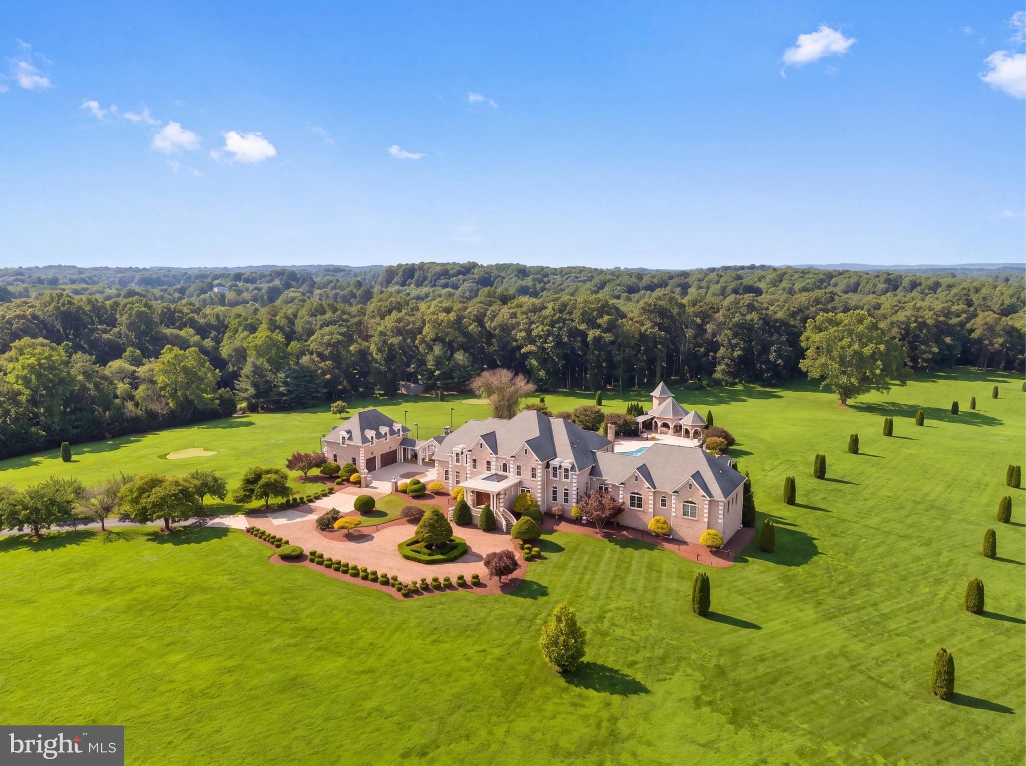 Privately situated beyond a gated entrance at the end of an established enclave, 15325 Masonwood Drive is a country estate set on 37.8 acres of pasture, mature woods, and thoughtfully designed amenities in one of the Capital Region's most peaceful settings. Spanning approximately 18,400 square feet across a main residence and detached guest quarters, the property combines generous living spaces, extensive recreational amenities, and a rare sense of privacy in the heart of Darnestown.

A long private drive winds through fully fenced grounds before arriving at a motor court. Double staircases frame the entrance, while carved wooden front doors open to an entry vestibule with illuminated art niches. Beyond, a marble foyer features a sweeping staircase and Baccarat chandelier. Designed to accommodate both large-scale entertaining and everyday living, the main level features 12-foot ceilings with tray and vaulted details throughout. Formal living and dining rooms flank the foyer in a traditional center-hall layout, while a coffered-ceiling family room provides a more relaxed gathering space.

At the center of the home is a fully renovated chef's kitchen equipped with Thermador appliances and Sub-Zero refrigeration. Contemporary in design, the space features European-style cabinetry, a waterfall island, and recessed lighting. An adjoining breakfast area overlooks the surrounding grounds. Six bedrooms are located on the main level, including a newly created primary suite with a renovated bath. An additional primary suite occupies the upper level, offering privacy, motorized blinds, and views across the property.

The lower level introduces an extensive collection of recreational amenities. A ballroom serves as the centerpiece of the entertaining spaces and is complemented by a temperature-controlled wine cellar, theater room, fitness center, sauna, steam shower, an additional bedroom, and expansive walkout living areas. Covered outdoor spaces with integrated gas lines for grilling provide a seamless connection to the grounds beyond.

The outdoor amenities are among the estate's defining features. A private 9-hole golf course winds through the landscape, accompanied by a heated in-ground pool, tennis and basketball sport court, and an outdoor kitchen and bar pavilion with a grilling station, ice maker, and beverage refrigeration. Terraces and open lawn areas create ample opportunities for entertaining while preserving the property's sense of seclusion.

A detached two-car garage includes a fully equipped guest apartment above with living areas, a kitchen, and en-suite accommodations. The lower level has been renovated to include an additional kitchen, two dens, a full bath, laundry facilities, and flexible-use space well suited for guests, extended stays, or estate staff. Supporting the property are multi-zoned geothermal heating and cooling systems, updated septic infrastructure, and numerous recent mechanical improvements.

Offering an uncommon combination of acreage, amenities, and privacy, 15325 Masonwood Drive presents a distinctive estate opportunity in one of Montgomery County's most scenic settings.