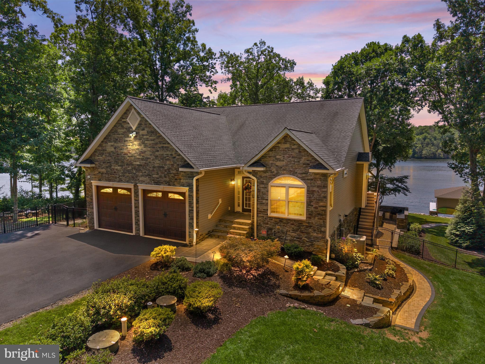 Lake Anna lake life doesn't get much better than this! On the point of a private cove on the public side of the lake in sought-after Pleasure Island, this beautifully remodeled transitional Colonial offers nearly 3,000 finished square feet of thoughtfully designed living space. Sold fully furnished, it features panoramic water views, exceptional indoor and outdoor entertaining spaces, and approximately 340 feet of fully riprapped shoreline on 2.3 acres. Located south of the Route 208 bridge, this home has every detail today's luxury lake buyer is looking for.
A striking stone front elevation, full-lite entry door with matching sidelights and transom window welcome you into a bright foyer showcasing hardwood flooring, crown molding, chair rail accents, and elegant arch-top grooved interior doors accented with sleek modern hardware throughout. The open-concept floor plan is centered around the newly remodeled gourmet kitchen featuring raised-panel soft-close cherry cabinetry, quartz countertops, an oversized center island with seating for four, stainless farmhouse sink, built-in convection microwave and wall oven, gas cooktop with range hood, stainless steel appliances, spacious pantry, recessed lighting, and an elongated hexagon tile backsplash. Extended built-in cabinetry with glass accents adds storage and serving space in the dining area.

The kitchen flows seamlessly into the dining area and family room where rich hardwood flooring, recessed lighting, a gas fireplace with wood mantel, and breathtaking panoramic lake views create the perfect gathering space.

The main-level primary suite features hardwood flooring, a tray ceiling with ceiling fan, bay window overlooking the water, and a sliding barn door leading to the ensuite bath with double vanity, frameless glass shower, walk-in closet, and private water closet. A second main-level bedroom features a tray ceiling, oversized arched window, ceiling fan, double-door closet, and easy access to a full hall bath with tile flooring and tub/shower with transom window. Completing the main level are a spacious laundry room with built-in cabinetry, utility sink, and interior access to the oversized two-car garage with rare 8-foot garage doors.

The finished walkout lower level offers engineered wood flooring, recessed lighting, a spacious recreation room highlighted by a whitewashed wood accent wall, and an impressive wet bar with farmhouse-style cabinetry, built-in wine storage, glass display cabinets, and refrigerator. Two additional bedrooms with water views, a private den or office, full bath with tub/shower, and generous storage room complete the lower level.

Outdoor living is equally impressive. Enjoy two screened porches—one off the kitchen and one off the recreation room—both overlooking the lake. The expansive patio features an outdoor kitchen with wet bar, built-in grill, side burner, mini refrigerator, built-in seating, illuminated pergola, and hot tub. Stone walkways surround the home and provide a gentle walk to the lake with no stairs. At the water's edge, the impressive boathouse features low-maintenance composite decking, two covered boat slips with lifts, a dock bar with refrigerator, screened porch, deep water, fully riprapped shoreline, and panoramic views. A waterfront stone fire pit creates the perfect setting for unforgettable sunsets.

Additional features include a whole-house generator, security system, water filtration system, electronic air filter, Xfinity high-speed internet and cable TV, irrigation system, rare paved driveway, storage shed, and a partially fenced rear yard.

Rarely does a Lake Anna property combine pristine condition, 2.3 acres, approximately 340 feet of shoreline, deep water, a double-slip boathouse with lifts, extensive hardscaping, panoramic views, and exceptional indoor and outdoor entertaining spaces. Offered fully furnished with kayaks, this is a truly turnkey opportunity to start enjoying the Lake Anna lifestyle from day one.