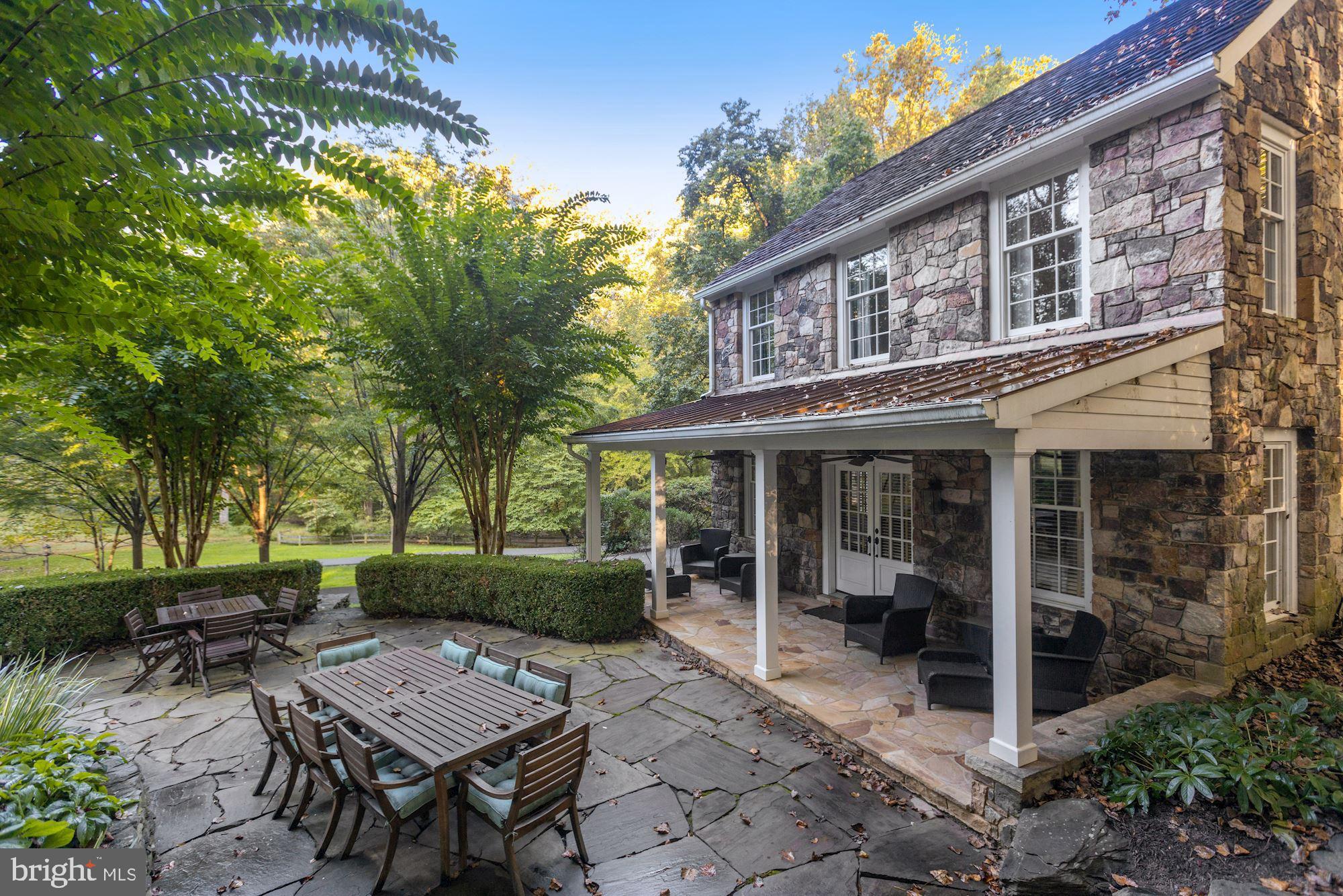 Sited on almost 2-acres with pastoral views, this charming farmhouse has been completely rebuilt, refurbished, renovated, and expanded.  Rustic details in this home integrate reclaimed wood from a circa 1790's Southern Maryland log structure into a thoroughly modern context, preserving its character through wood-beamed ceilings, wide-planked hardwood floors, painted walls with a hand-hewn effect, stylized barn doors, exposed brick and elegant wood paneling to round out the finishes. The heart of the home features what is believed to be the original fireplace with its fieldstone hearth located in the wonderfully warm kitchen with classic English-style cupboards and gourmet appliances,  A circular driveway, separate guest house and detached three car garage add to the enchanting property.   Two covered porches and a stone patio allow the outdoors to blend seamlessly with the interior, and large beautiful windows enhance almost every room. A family entryway from the rear yard leads to the kitchen, the true heart of this home, flanked by both formal and casual wings. Two staircases connect to the second level where bedrooms are bright, spacious, and restful and baths are updated, accented by clean marble tops and classic tile finishes. The owner's suite's expansive sitting area with fireplace leads into a generous walk-in closet and fresh spa-like bath with steam shower. The lower level with wine cellar, wet bar, full bath, exercise room and recreation room maintains the theme of restful living, as do the perfectly proportioned living quarters in the separate guest house. Friends and family will benefit from the separate studio suite with bathroom and full kitchen, where au-pair living configurations can also abound. Offering ultimate privacy and plentiful greenery views, the almost two-acre grounds are a secluded retreat with easy access to both Georgetown Pike and Old Dominion Rd, maintaining the convenience of accessible amenities while preserving a countryside feel that is utterly timeless.