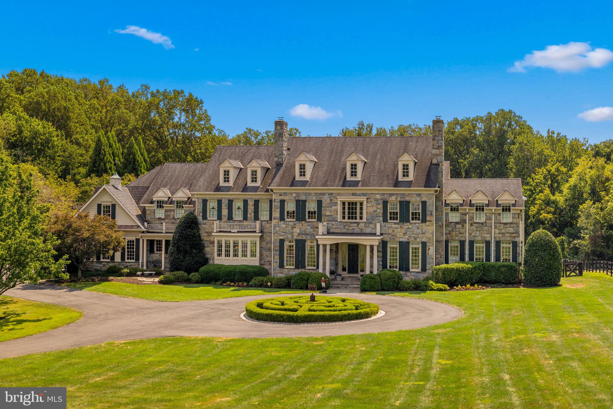 First time offered for sale, this exceptional 5-acre estate is nestled at the end of a private road 
surrounded by lush gardens and mature trees. The custom designed field stone manor home boasts timeless elegance and offers over 12,000 Sq ft of living space.   A circular drive framed by boxwoods leads you to the grand portico. Entering the home, grandeur unfolds with soaring 12’ ceilings, luxurious cornice moldings, wide plank floors and a towering 2 story wall of windows looking out to the verdant backyard.  The two-story foyer with double curved staircase and in-laid rosewood compass medallion in the center are breathtaking. The main level features elegant formal rooms grand in scale and include a living room and dining room with period fireplace mantels and antique lighting. Unique features include a butler’s pantry hidden behind pocket doors, custom designed pine library, extra wide hallways, a separate guest coat closet, formal powder room and light-filled conservatory with double doors opening to the porch. The kitchen boasts Sub-Zero, Viking Professional, and Thermador appliances as well as custom cabinetry and a large island with warming oven.  A sunken family room flows off the kitchen with custom built-ins, floor to ceiling stone fireplace with gas logs and large windows bringing in lots of light. A morning room is off to the side with
double doors leading to the backyard terrace and fountain. The first floor includes a pantry, catering kitchen with additional Sub Zero, mudroom with cubbies, half bath and sports closet. Two separate staircases lead to the upper level where 5 spacious bedrooms with en-suite bathrooms can be found. Arches mark the hallways to each end of the house. The laundry room has linen closets on each side of the entry door, built in cabinets and shelves for folded laundry. A children’s library with built-in bookshelves and window seats for storage can be found at the end of one hallway while the master suite sits at the other end. A circular entry foyer with inlaid wood medallion leads to the master bedroom where a sitting room with gas fireplace, coffered
ceiling, 2 expansive walk-in closets and separate cedar-lined closet await. The bath is adorned with Carrera marble, dual vanities, whirlpool tub beneath a Palladian window and walk-in marble shower. The lower level includes a sports game area designed for 3 TVs to keep up with games or play X-Box; custom bar area, billiards room, sitting area with fireplace, exercise room, half bath, au pair suite with en-suite bathroom and 2 storage closets. A professionally designed and installed home theater features Klipsch surround sound and leather seats. A custom-designed wine cellar accommodating over 800 bottles features a built-in humidor. The outdoor patio with towering stone fireplace, built-in gas grill and bar are designed for year round enjoyment and ideal for gatherings under the stars. Formal gardens with boxwood hedges and fountain set the stage. A 50’ x 20’ heated pool with retractable cover and hot tub are hidden off to the left. Stone pillars with an antique gate frame the exit from the pool area to he rest of the property. There is room for tennis/pickleball courts or for a barn and riding ring. The garage has 2/3 parking spots including a double bay for a large SUV. A parking area outside the garage accommodates additional cars.  This property boasts 4-zone HVAC, updated water heater and water monitoring system, water purification system and pressure systems, whole-house CAT5 wiring and audio, and a 30-year Grand Manor roof. <iframe width="560" height="315" src="https://www.youtube.com/embed/vRgKKRW7To4?si=SMmUkCT3A0XRgD9g" title="YouTube video player" frameborder="0" allow="accelerometer; autoplay; clipboard-write; encrypted-media; gyroscope; picture-in-picture; web-share" referrerpolicy="strict-origin-when-cross-origin" allowfullscreen></iframe>