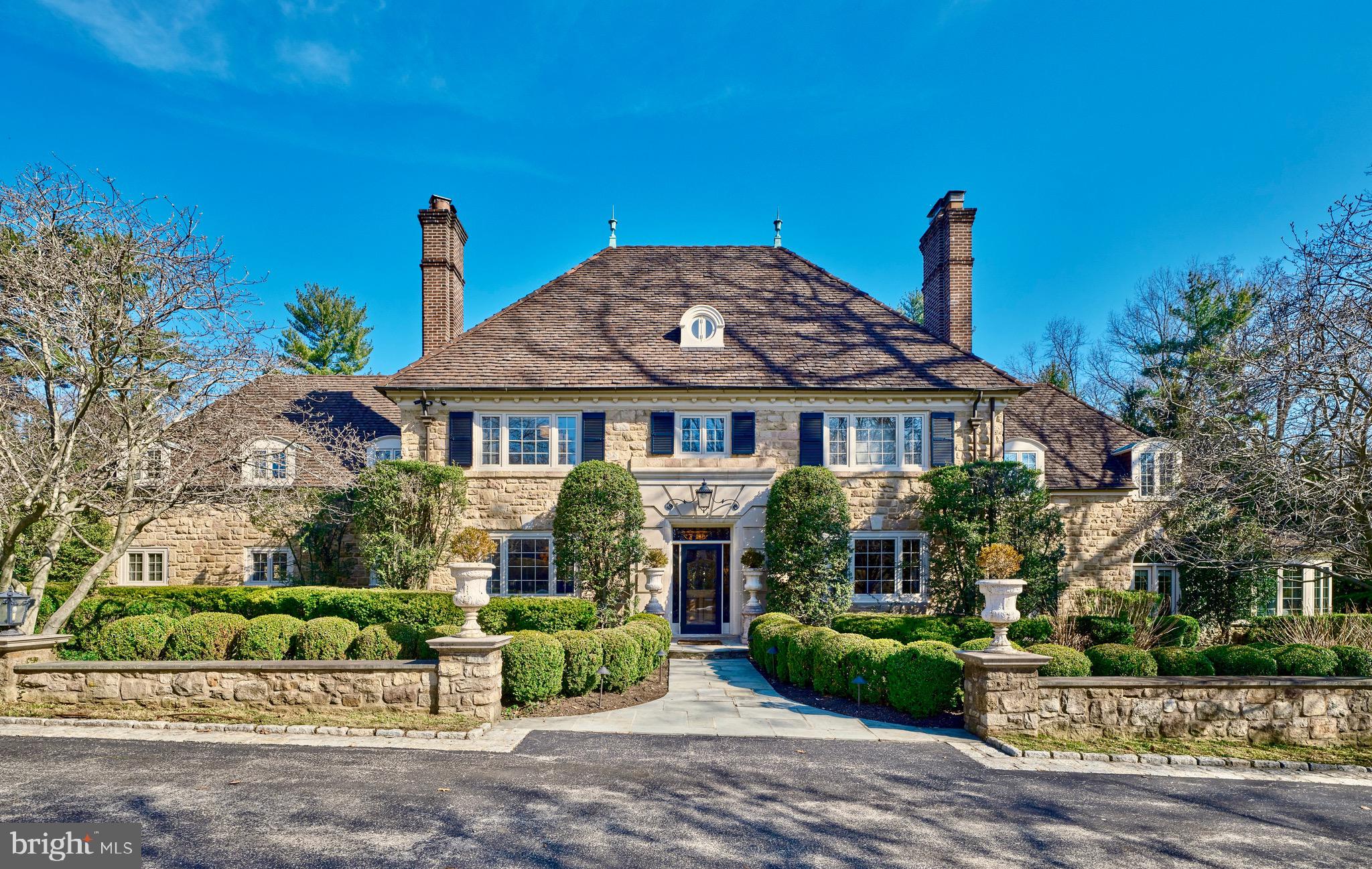 A Gracious Main Line Estate | Situated on one of the most coveted streets in Northside Bryn Mawr within the award-winning Lower Merion School District, this distinguished property presents the opportunity to acquire a thoughtfully enhanced 1938 stone residence set on two acres of private grounds in the heart of the Main Line. Positioned along prestigious Ridgewood Road, the estate merges enduring character with resort-caliber amenities including a regulation sport court, swimming pool and spa, guest house, formal gardens, stone terraces, and a charming courtyard. The residence offers 6,273 square feet of interior living space, with approximately 8,846 total estate square feet including additional structures, four fireplaces, and parking for more than eight vehicles across the temperature controlled two-car attached and two-car detached garages + gated driveway. Additionally, there is a third one-car garage located at the rear of the property, attached to the pool/guest house.
At the center of the home is a fully renovated chef’s kitchen designed for both daily living and larger gatherings. The space features Calacatta Paonazzo honed marble countertops and backsplash, bespoke cabinetry, and a professional appliance suite including a 60-inch Wolf dual fuel range, Sub-Zero refrigerator and freezer, Sub-Zero refrigerator drawers, and Sub-Zero wine storage. A well-appointed butler’s pantry with an additional dishwasher and ice maker provides exceptional support for hosting.
The main level unfolds through formal living and dining rooms, a cherry-paneled library with a fireplace, and a tranquil sunroom defined by exposed stone floors and walls, a custom bar, and expansive garden views.
Upper levels provide five bedrooms including a primary suite featuring vaulted ceilings, sitting area, walk-in closets, and a marble spa bath,
The walk-out lower level expands the residence with a recreation room centered around a stone fireplace, fitness studio, wine room, laundry area, and additional flexible-use spaces.

This remarkable offering presents privacy and estate-scale living, complemented by a welcoming atmosphere of warmth and a true sense of home, on one of the Main Line’s most established addresses.