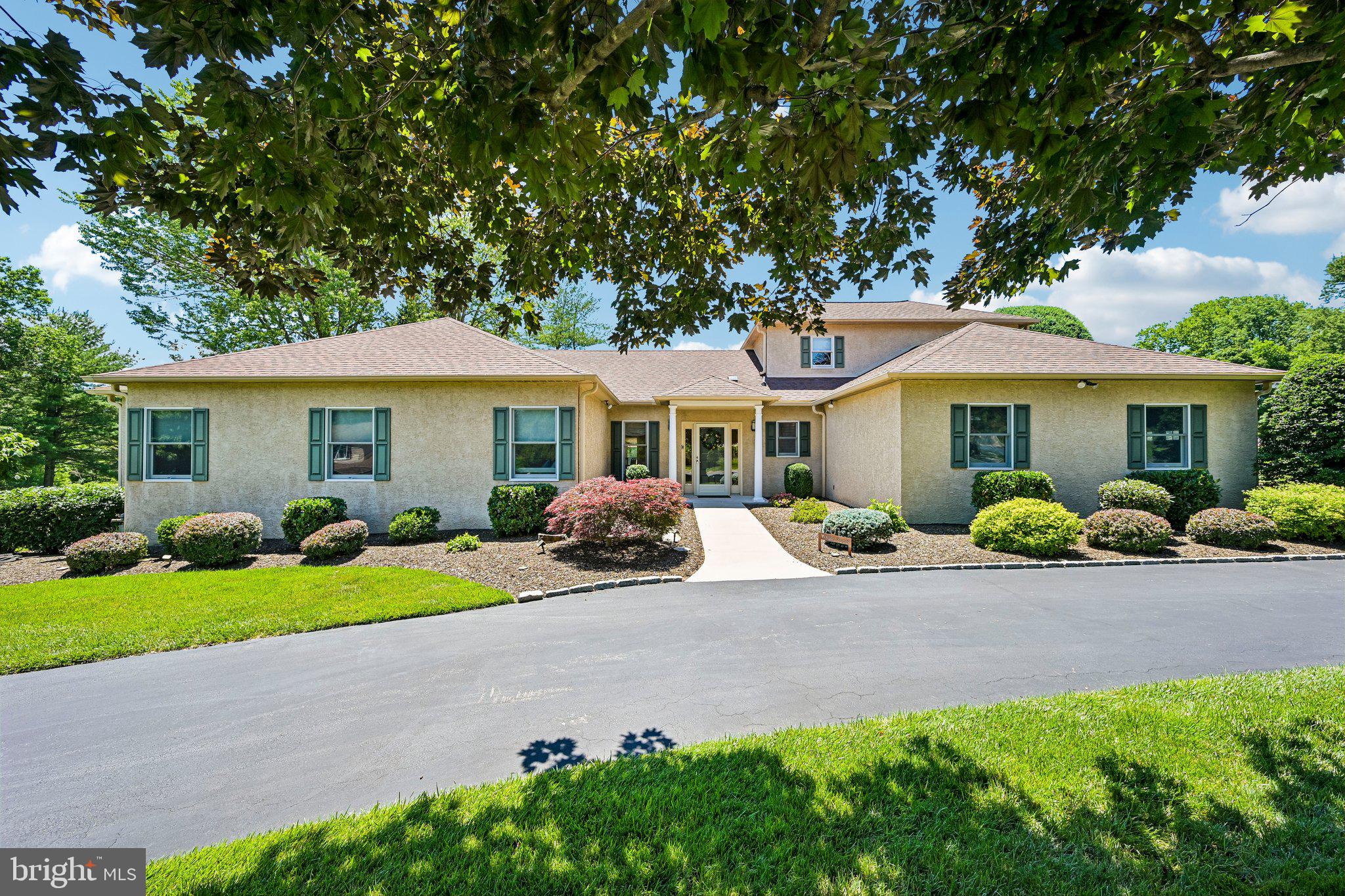 Lovingly maintained by its original owners since it was custom built in 1985 by Sal Paone, this custom ranch offers a refined blend of privacy, thoughtful updates, and resort-style outdoor living. Set on a corner lot with a circular driveway and beautifully maintained grounds, this 4-bed, 5.5-bath residence delivers more than 3,000 square feet of living space with a layout that has been expanded over time.
From the level entry, the home opens into an elegant and well-kept interior where wood floors, generous windows, and a graceful floor plan set the tone. The formal living and dining room combination overlooks the rear grounds, creating a serene backdrop for everyday living and entertaining. At the heart of the home is a gourmet kitchen remodeled 3 years ago. Designed with both beauty and function in mind, it features crisp white cabinetry, stainless steel WiFi-connected appliances, including a GE refrigerator with water dispenser, beverage refrigerator, and GE electric induction cooking, along with a large island with seating, eat-in table space, bar and wine storage, multiple prep zones, pantry cabinets, and sweeping views of the backyard. The kitchen connects naturally to the expanded living spaces, giving the home an effortless sense of flow.
Just off the kitchen, the first family room features a brick gas fireplace with mantle, plantation shutters, and a comfortable connection to the kitchen. The first addition offers a large family room with radiant heat tile floors, exterior access, TV space, and abundant windows. A second living area creates a sunroom experience with rich wood ceiling details and an inviting indoor-outdoor feel that adds to the home’s custom appeal. The bedroom layout is equally thoughtful. Three bedrooms are positioned off the main living area, including a spacious primary suite with thoughtful details such as light switches near the bed and remote window shades, along with a walk-in closet and access to the deck. The spa-style primary bathroom, updated in 2018, features radiant heated floors, an automated fan, a large rain shower, and a neutral gray design. A second bedroom includes a custom updated ensuite bath with designer details, a wide doorway, a Toto toilet, an English designer-grade butterfly sink, and an oversized shower with one-step entry. This bedroom also includes a mini-split system for added heating and cooling. The third bedroom offers great closet space. A newly updated 2024 laundry room with Electrolux washer and dryer, cabinetry for storage, and an updated neutral gray bathroom from 2018 with tub/shower complete the first floor.
Upstairs, the fourth bedroom suite includes a cozy seating area, walk-in closet, and full bath, offering a private and versatile retreat for a guest room or in-law suite. The  finished basement further extends the versatility of the home with more living space, a full bath, office, recreation area, cedar closet, workshop, and storage. The 2-car garage includes a mini-split HVAC system and a professional golf simulator setup, allowing for year-round use. A whole-house generator provides uninterrupted comfort and peace of mind by powering the entire home during outages. The backyard is the showstopping feature of this home and has been the centerpiece of family gatherings for many years. It offers a private resort-style setting with a fenced yard, privacy hedges, grassy lawn with playground, heated in-ground pool, hot tub, Trex deck, fire pit, and pavilion with a 55-inch weatherproof television. Together, these amenities create a true backyard retreat for relaxing, entertaining, and making lasting memories. The stucco was replaced 8 years ago, and the home has benefited from multiple additions and updates over the years. Served by the Upper Dublin School District and  located near the PA Turnpike, trains to Philadelphia, and Dreshertown Plaza, this elegant custom ranch offers a rare blend of privacy, comfort and flexible living spaces.