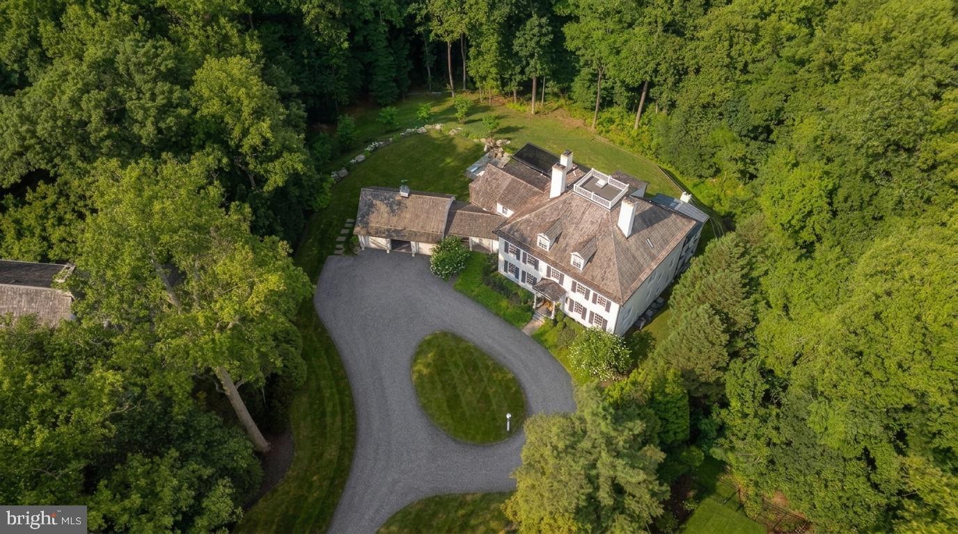Tucked away behind the nationally-renowned Congressional Country Club, its namesake Country Club Drive is one of Bethesda’s most prestigious streets, with a mere 26 of the very finest estate homes dotted along sweeping curves in a picturesque setting. Within this rarified air, at the apex of a verdant cul-de-sac, is this quintessential colonial estate home. Tucked away far back from the street, its elegant approach is via an elegant circular driveway, revealing a white brick facade capped by a cedar shake roof evoking cues of classic old-world New England colonials situated on large swaths of land, and exuding an ethos of quiet luxury. Contrasting black shutters infuse the classic exterior with a modicum of modernity as one approaches the central front door via flagstone walkway. The blend of tradition and currency is further carried through the interiors, which have been comprehensively reimagined to suit the tastes of a contemporary luxury clientele while retaining its quintessential elegance. A traditional center hall foyer is flanked by embassy sized formal living and dining rooms. The former can be discreetly closed off via pocket doors, enjoying an ethereal palette augmented by natural light flooding in from the Palladian window on its far side, illuminating the roaring fireplace wall flanked by custom built-ins. The latter also showcases a fireplace, one of five in the home, this one featuring a bold, dark marble surround to complement the moody, sophisticated palette à la fine dining establishment – for sophisticated large scale entertaining. A transverse gallery bifurcates the main level’s formal and informal spaces, with the large family room and its wall of glass, rustic floor-to-ceiling stone fireplace wall, and patio access serving as a midpoint. The chef’s kitchen is the heart of the informal wing. Enjoying almost a European-level of minimalism, its white shaker cabinetry and matching counters conceal a comprehensive suite of state-of-the-art appliances, and are contrasted by a dark, full-height backsplash wall. A large family entrance and mudroom, additional powder room, connection to the butler’s pantry, and direct access to the oversized three-car garage are conveniently tucked away in this wing. A private library with built-ins connected to a spacious den surrounded by glass, both with coffered ceilings, completes the main level. A transverse hallway on the upper level commences at the top of the sweeping staircase and mirrors that of the gallery below. The exquisite primary suite spans the entire width of the upper level, with a large bedroom overlooking the lush grounds. The central dressing room is akin to a luxury boutique in scale and layout, with multiple nooks all surrounded by extensive illuminated built-ins. Minimalist yet still lavish, the primary bath boasts the ubiquitous double vanity, freestanding soaking tub, separate water closet, and walk-in shower. Three additional generously proportioned bedrooms, each with a designer ensuite bath, complete the upper level alongside a spacious and conveniently located laundry room. A finished third level comprises two additional private bedroom suites, ideal for young adults, a fitness studio, bonus space, or a fully private telecommuting solution, as well as ample storage space. A comprehensive entertainment zone, the lower level revolves around a substantial recreation room which spans over 47 feet in length. A professional home cinema is found at one end, while a large fitness center and step-down game room, currently set up as a golf simulator, are found at the other. A spa-inspired bath including a full sauna completes the space. The home’s outdoor space is another certain highlight, occupying 2.06 coveted acres in a proximate Bethesda location. The manicured landscaping is complemented by a flagstone patio, comprising a pergola above a modern linear fire pit, full outdoor kitchen, and sunken hot tub.