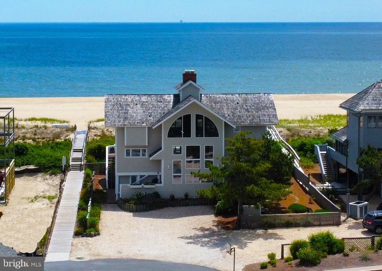 Absolutely stunning oceanfront views from nearly every angle of this timeless beach home that is situated on a large lot with 75 ft of oceanfront property. Architecturally designed for multiple generations to enjoy time together at the beach, this spacious home offers 5 bedrooms, 4 full and 1 half bath plus a large additional family room. The impressive great room is full of coastal charm and character featuring a 2-story stone fireplace, exposed beam soaring wood ceilings, and wide plank wood walls painted a crisp white.  The kitchen has been beautifully updated with new cabinetry, stainless steel appliances, and large center island with seating. Open the large glass doors between the kitchen and screened porch and easily combine the 2 dining areas for beachfront entertaining and continue onto the oceanfront deck that spans the entire length of the home. Also on the main level is a spacious bedroom with access to the oceanfront deck and an adjacent full bathroom. Upstairs there are 2 primary bedrooms, one of which has private access to a balcony with views up and down the coastline. The lower level offers a large additional family room, 2 bedrooms, and 1.5 baths. From the lower level you can step out onto a large covered porch with a lovely porch swing and multiple outdoor showers plus access to the dune crossover to the beach. Offered fully furnished, this home is ready to be enjoyed. Positioned on a large parcel in a private North Bethany neighborhood, this impressive home is adjacent to the dune crossover and is close to the town of Bethany with a beautiful lifeguarded beach.