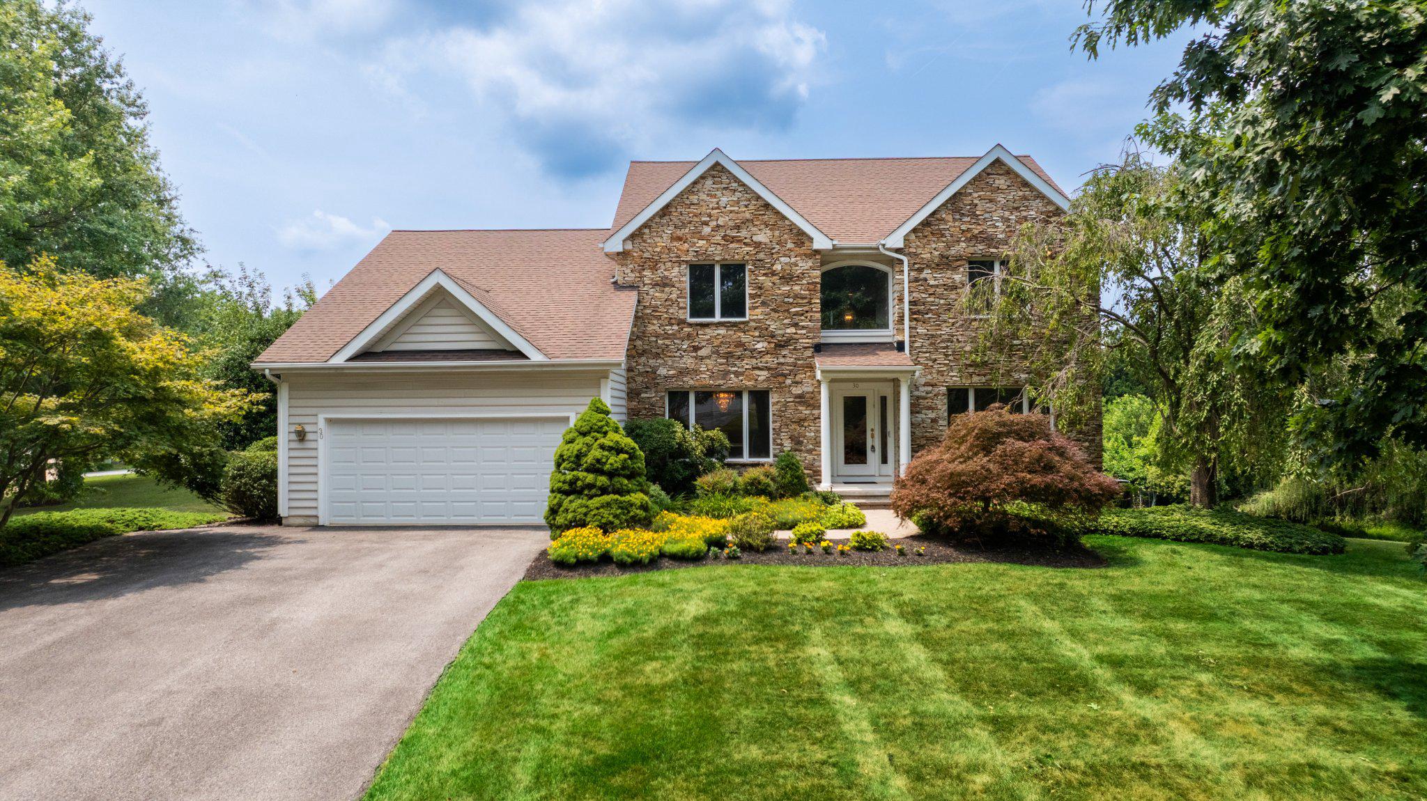 Welcome to this exceptional stacked stone-front home, gracefully sited on a beautifully landscaped three-quarter-acre corner lot in the highly sought-after Worthington Park community. A lighted brick paver walkway leads to the inviting entrance, where soaring ceilings, abundant natural light, timeless neutral décor, and impeccable maintenance create an immediate sense of elegance. Meticulously cared for and truly move-in ready, this home offers an exceptional blend of luxury, comfort, and thoughtful design.

The flowing circular floor plan begins with a dramatic two-story foyer showcasing beautiful hardwood floors that extend throughout the living room, dining room, and center hall. At the heart of the home is the impressive two-story family room, highlighted by a marble fireplace and seamlessly connected to the beautifully appointed gourmet kitchen. Designed for both everyday living and entertaining, the kitchen features custom Brookhaven solid maple cabinetry, granite countertops with a tumbled marble backsplash, stainless steel appliances, a warming drawer, a center island with cooktop, and a spacious breakfast area. Just beyond, the stunning sunroom addition is surrounded by floor-to-ceiling windows on three sides, offering panoramic views of the picturesque backyard.

The expansive main-level primary suite is a private retreat, featuring a vaulted ceiling, two walk-in closets, and a dedicated study—a desirable builder upgrade ideal for a home office or sitting room. The luxurious spa-inspired bath is beautifully finished with travertine, offering a Kohler soaking tub, custom Brookhaven dual-sink vanity with granite countertop, and an oversized walk-in shower with multiple shower heads for a true spa experience.

Upstairs, three generously sized bedrooms share a well-appointed full bath. The expansive walkout lower level provides exceptional flexibility with abundant space for recreation, games, fitness, and storage, along with a true fifth bedroom and full bath—perfect for guests, extended family, or an au pair suite.

Outdoor living is equally impressive, with a spacious brick paver patio and composite deck with retractable awning overlooking beautifully landscaped grounds. Professionally designed and meticulously maintained, the lush backyard features a vibrant mix of mature trees, flowering shrubs, and colorful perennial gardens, creating a private, park-like setting that offers beauty and tranquility throughout the seasons.