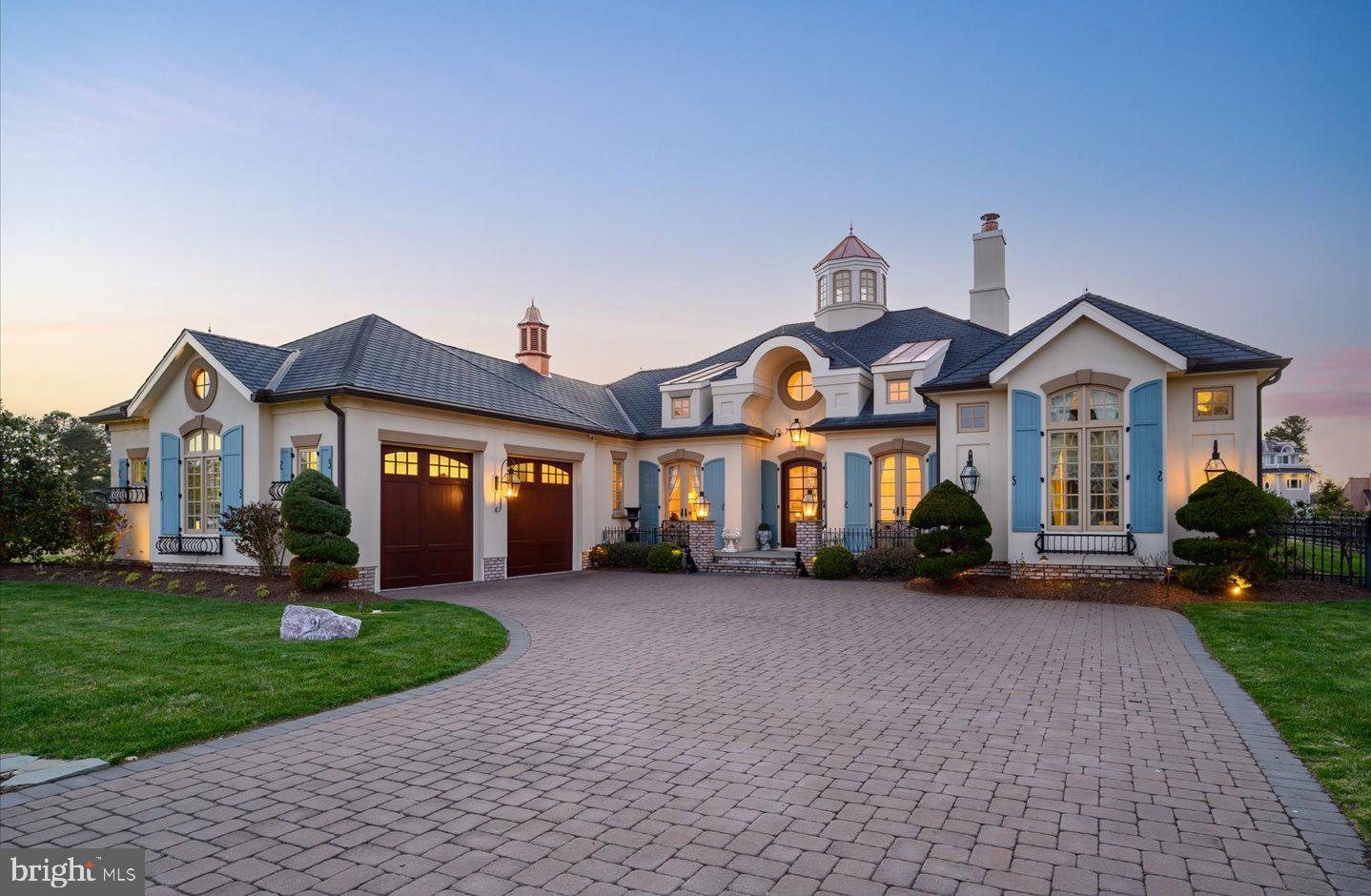 Welcome to 91 Blackpool Road—an exquisite French country-inspired waterfront estate nestled within the prestigious Rehoboth Beach Yacht & Country Club. Perfectly positioned along the serene Bald Eagle Lagoon with direct access to Rehoboth Bay, this architectural masterpiece offers an exceptional blend of elegance, craftsmanship, and coastal luxury—with the added convenience of one-floor living. From the moment you arrive, the home’s striking curb appeal, paver driveway, and lush landscaping set the tone for what awaits inside. A grand, light-filled foyer crowned by a dramatic cupola welcomes you into a thoughtfully designed open floor plan, where soaring vaulted and beamed ceilings and abundant natural light create a warm yet sophisticated atmosphere. Spanning 3,616 heated square feet, this 4-bedroom, 3.5-bath residence is rich in high-end finishes, including radiant heated marble floors, hardwood flooring, and spa-inspired marble baths. The gourmet kitchen is a true showpiece, featuring commercial grade dual refrigerators, an ILVE French gas range with hood, wall oven, dishwasher, marble countertops, tile backsplash, and a spacious pantry—seamlessly flowing into the dining area and expansive living room, ideal for entertaining. A beautiful wet bar with beverage fridge and ice maker enhances the home’s entertaining appeal, while a cozy den provides a more intimate retreat. The waterfront owner’s suite is a private sanctuary, offering tranquil views, an oversized custom closet with built-ins and center island, and a dedicated laundry area for added convenience. Every detail has been carefully curated for comfort and luxury. Outdoor living is equally impressive. A screened, covered porch overlooks the water, while the expansive terrace invites you to relax or entertain beside the heated saltwater pool and spa. The bulkheaded lot with riprap shoreline provides both beauty and function, and a private boat dock complete with boat and jet ski lifts makes enjoying life on the water effortless. Additional highlights include a laundry/mudroom with ample storage, a two-car courtyard garage, and most furnishings included for a turnkey opportunity. As part of this sought-after community, optional membership to the Rehoboth Beach Country Club offers access to an 18-hole championship golf course, clubhouse, pool, tennis, and pickleball. This is a rare opportunity to own a truly distinctive waterfront home where timeless European charm meets modern coastal living.