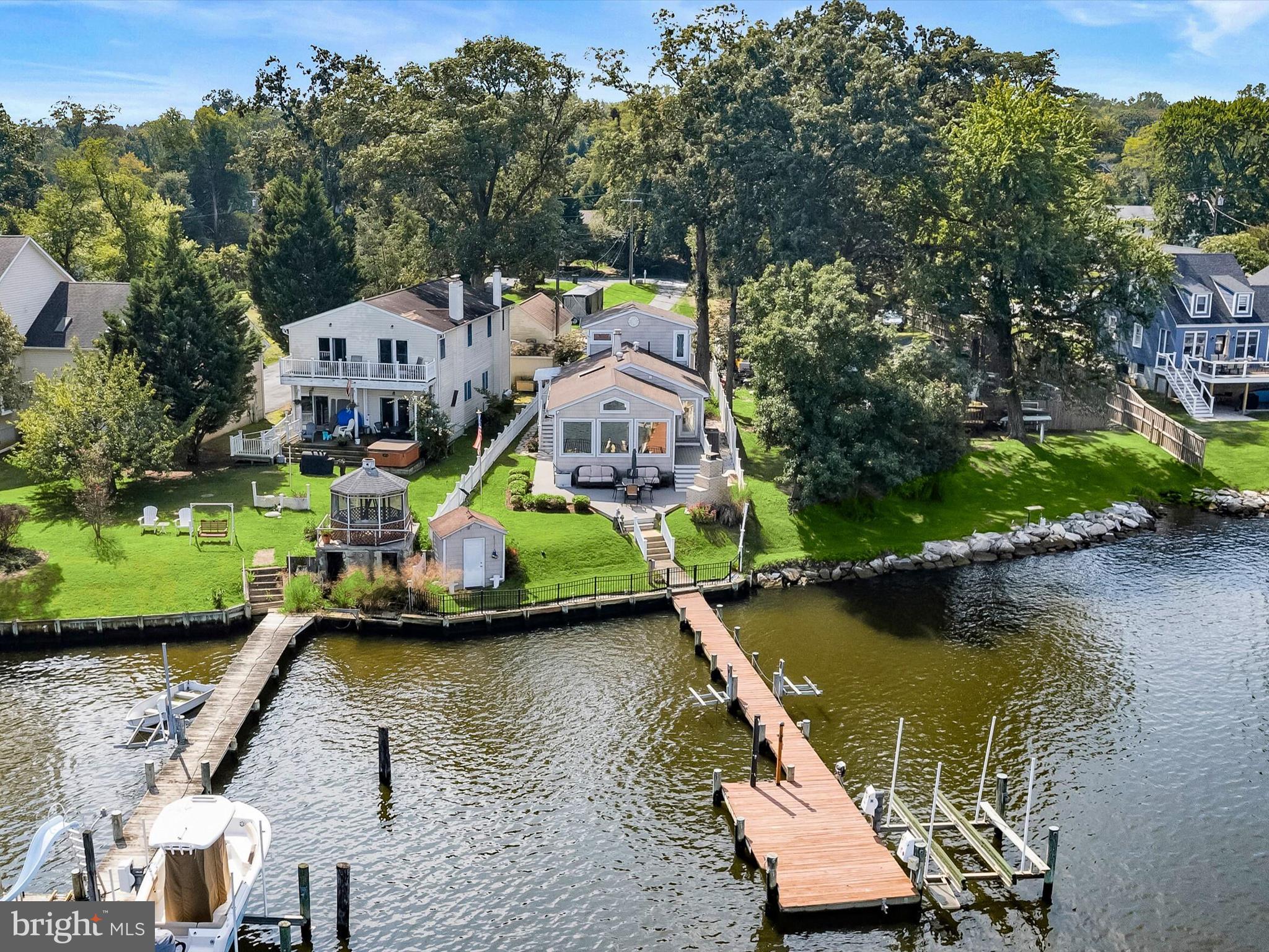 Imagine waterfront living on Bodkin Creek with direct access to the Chesapeake Bay, where every day feels like a retreat. This home is fully equipped with a private pier with 8ft MLW, a boat lift, two jet ski lifts, an outdoor shower, and 30 Amp electric service, perfect for boating, fishing, or simply enjoying the water. Step inside to a spectacular living room with a cathedral wood-planked and beamed ceiling, three oversized windows framing serene water views, and a striking stone accent wall. A pass-through to the kitchen with a seating bar connects the spaces effortlessly, while hardwood floors flow into the dining room, ideally situated between the living room and kitchen, with easy access to the expansive Trex deck overlooking the water. The kitchen impresses with a vaulted ceiling and skylight, granite countertops, stainless steel appliances including a double oven, and a center island with breakfast bar. Another breakfast bar in the pass-through overlooks the living room, perfectly combining function with water views. The main level also includes a renovated full bath with generous shower and a primary bedroom with a walk-in closet and loft, complemented by a convenient laundry room just off the entry to the bedroom. A newly built staircase (to replace spiral staircase previously there) leads to the lower level, which includes two additional bedrooms, one featuring a Clear Light Infrared sauna for ultimate relaxation, as well as a hall bath and storage closets. Outdoor living is equally impressive, with a Trex deck and outdoor stone fireplace overlooking the water, vinyl privacy fencing along the side, and aluminum fencing on the waterfront that preserves unobstructed views. Additional features include a 1-car detached garage, carport, and storage shed in the driveway. The property is enhanced with numerous modern updates, including complete deck and stair replacement with Trex composite, a professionally installed mini-split air conditioner in the primary bedroom loft, and upgraded garage electrics with two electric vehicle chargers. Other upgrades include a new garage door and opener, pier maintenance and repairs, new heating oil tank and replaced oil lines, shed roof replacement, new washer and dryer with proper vent installation, roof repairs, water softener upgrades, generator maintenance, basement vent fan installation, and a professionally installed IP camera security system with three exterior cameras and full on-site recording. Every detail of this waterfront property has been meticulously curated to combine luxury, functionality, and effortless water enjoyment, offering a lifestyle defined by comfort and relaxation.