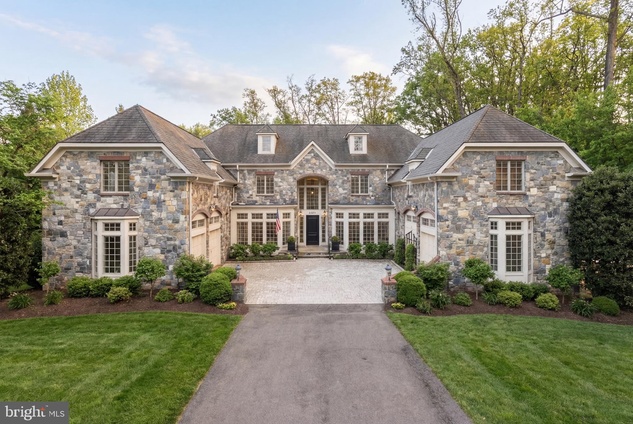 Few homes in one of McLean's most coveted enclaves offer this combination of scale, sophistication, and a setting that feels genuinely private. Set on nearly three-quarters of an acre in highly sought after Langley Forest, this thoroughly updated English-style residence delivers close to 9,500 square feet across four finished levels — with eight bedrooms, six full baths, and two half baths — architecture and volume that announce themselves the moment you arrive and deepen with every room you enter.

The motor court sets the arrival sequence. Two flanking garages frame the approach with the kind of symmetry that belongs on a different continent, while extensive professional landscaping — layered plantings, mature specimen trees, considered hardscaping — carries that intention all the way to the rear. The backyard is fully fenced, a large and genuinely private expanse that functions as a true outdoor room.
Inside, the scale is immediate. Soaring ceilings throughout the home — vaulted in the family room, grand in the formal rooms, generous on every level — give the interiors a presence that photographs struggle to capture. Custom millwork, gleaming hardwoods, and refined finishes establish the tone in the living and dining rooms flanking the entry foyer. The family room commands attention with its vaulted ceiling and oversized windows that pull the landscape in. The gourmet kitchen is the working heart of the home — light-flooded, generous in counter and cabinet space, with a breakfast area that opens directly to the rear terrace and screened porch. A library with a fireplace anchors the north wing.

Eight bedrooms across four levels offer flexibility that few homes can match. The main level suite handles guests or multigenerational living without compromise. The upper-level primary suite is a destination unto itself — sitting room, custom cherry walk-in closet, and a spa bath with separate vanities. A third suite provides an additional private retreat ideal for extended family or a dedicated executive workspace. The lower level completes the picture with a recreation room and wet bar, wine cellar, home theater, exercise room, and sauna.

Minutes to Tysons, Georgetown, and Dulles. Langley High School pyramid.