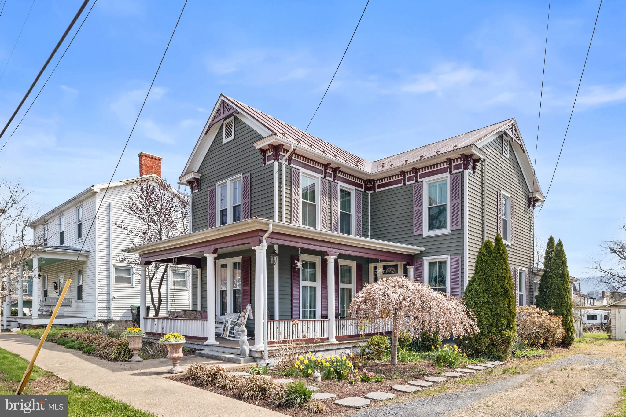 This lovely Victorian greets you with it’s bold and commanding presence softened by perennial plantings for 4 seasons of beauty. A cheery original, ornate yellow door bids you welcome.  Once inside, you’ll find that this home has been lovingly updated without compromising it’s beautiful character and charm.  Original entrance columns, nine foot ceilings, hardwood floors, transoms over interior doors, lots of built-ins and a sweeping staircase are just a few of the quality features.   Sunshine filters in through large windows and gas logs offer a cozy den to relax at the end of the day.  A new and functional kitchen with upgraded counters, custom built cabinetry, massive island space and modern appliances are a cook’s dream.  The dining room will easily seat an extended table and is tastefully decorated with wallpaper from days past.  Showcase your treasured dishes in the built in cabinetry.   The main level also includes the front parlor or the perfect at home office with custom built-in bookcases.   A bath has been added for convenience to this main level.   On the upper level you’ll find 4 bedrooms, full bathroom and laundry, plus those winding back stairs that are a shortcut to the kitchen.  Did I mention the stairs to the attic?  Use as storage or finish off for more living space!  There’s even more to enjoy- stepping into the screened porch with hookups ready for a hot tub, and ample sized deck cut around a live tree offering shade during the summer.  A detached garage, great for housing the mower or extra storage and private driveway are additional features.
The partially fenced back yard offers both privacy and open space, including two raised garden beds ready for spring planting.  The major components of this home have been updated such as vinyl siding, windows, HVAC system, and freshly painted roof and gingerbread trim.   So make your move in 2026!  Take in the scenic mountains and breathe in the country air, it’s waiting here for you.