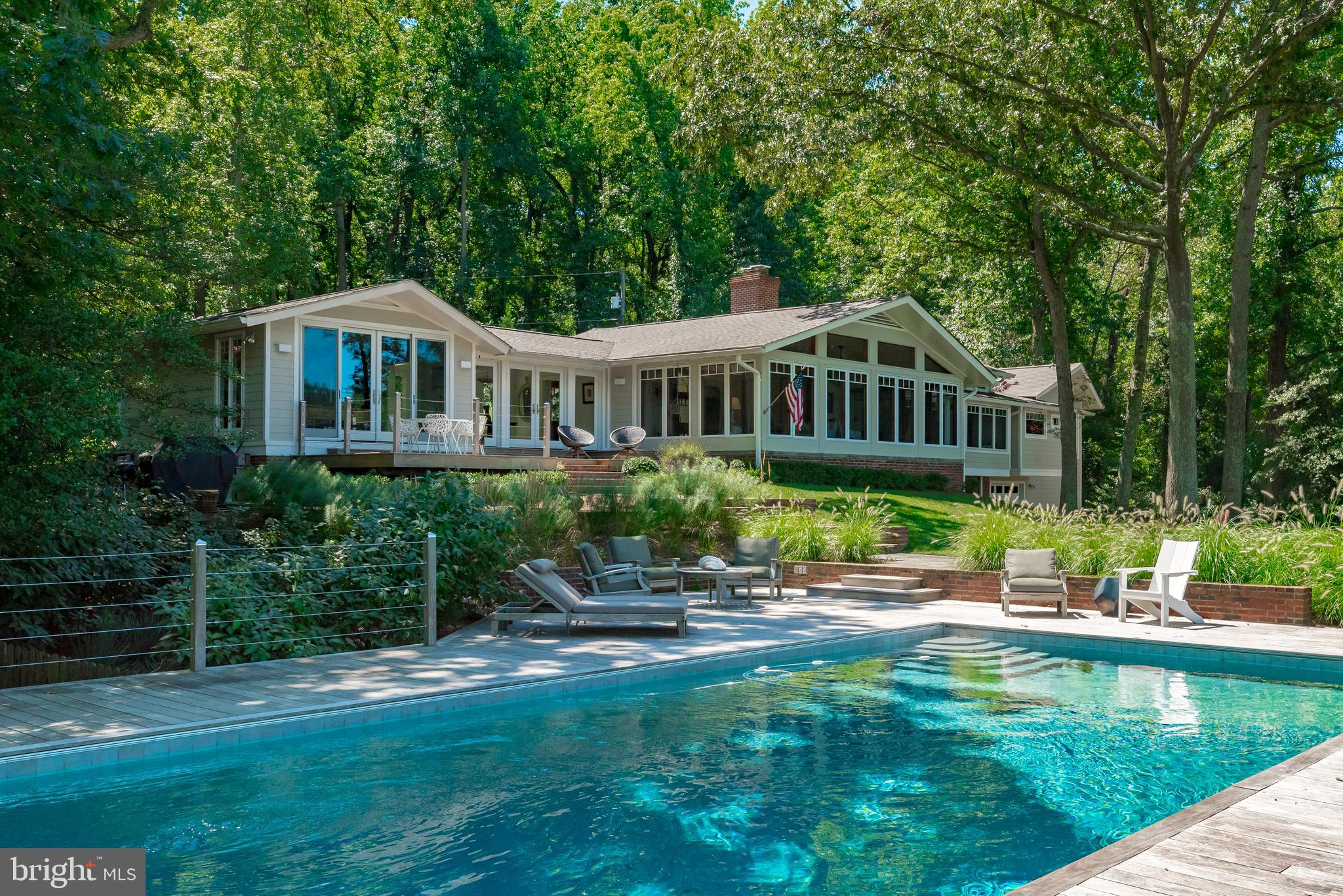 Possibly the largest and most private parcel in Bay Ridge, 197 West Lake Drive presents a rare opportunity to own a spectacular coastal waterfront property in one of Annapolis' most popular neighborhoods. Just minutes from the United States Naval Academy and the boutiques, shopping, and restaurants of historic downtown Annapolis, this inspired, contemporary, light-filled 4BR/3BA home is located down a long, private drive on a peaceful 2-acre lot with 440 feet of sheltered water frontage. Sustainably landscaped, the expansive lawn slopes gently down to the water with sweeping views of Lake Ogleton, while the protected, private pier, buffeted by undisturbed wetlands, provides unlimited access to the Chesapeake Bay. Grandfathered, custom boat house with boat lift and waterside saltwater pool. Separate waterfront outbuilding with loft allows for seamless indoor/outdoor living. Completely remodeled gourmet kitchen connects to great room with wood-burning fireplace, full zinc-topped wet bar with copper sink and ice maker, and soaring, vaulted ceilings ideal for entertaining. Radiant heated flooring in foyer, kitchen, and primary bath. Partially finished basement with walk-out family room and lots of storage. New, oversized, detached 2-car climate-controlled garage with electric vehicle charger. New generator with extended running fuel powers the entire property. This home has only been owned by two families and has been lovingly maintained and updated with many significant improvements. The home is also notable for being featured in the 2008 Ridley Scott film Body of Lies starring Leonardo DiCaprio and Russell Crowe. Home to the Chesapeake Bay Foundation, Bay Ridge is a very active community with many amenities and opportunities to be social year-round, like the annual Fourth of July Parade. Great walkability and scenic routes for cycling. Ride your golf cart to the marina, clubhouse, and ball courts, including pickleball! There's something for everyone in this historic neighborhood. Rt. 50 and 97 provide direct access to Baltimore, BWI, Ft. Meade/NSA, Washington, DC, and the Eastern shore. Welcome home!