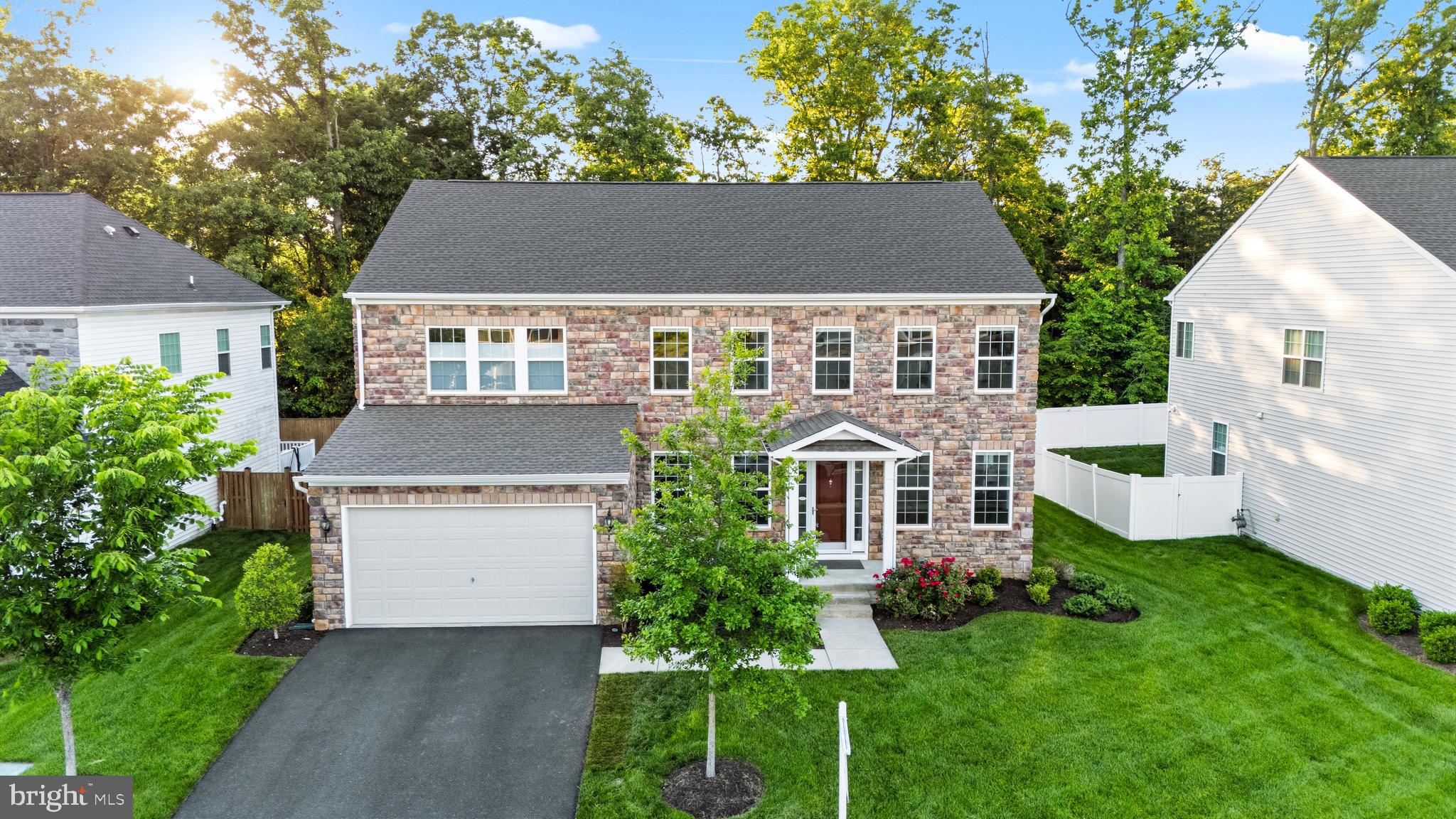 Welcome to 8934 Hubbard Way in Laurel Hills Crossing, Lorton. Five bedrooms, five and a half baths, 4,459 finished square feet across three levels, all-stone front, two-car garage. The kind of home that buyers wait months for in this community.

The main level lives big and lives smart. A two-story family room with a marble-surround fireplace sits at the center, with floor-to-ceiling sheers and a statement staircase. Wide-plank LVP runs throughout. The kitchen has white shaker cabinets with gold hardware, granite counters, gas cooktop, double wall ovens, French door refrigerator, walk-in pantry, and a dark contrasting island with seating under twin gold and crystal pendants. The breakfast nook opens to a composite deck that overlooks woods, not neighbors.

The formal dining room features wainscoting, crown molding, and a statement chandelier. There is a separate formal living room and a main-level in-law suite with a private full bath, which gives you real single-level living for guests, a parent, or anyone who needs to skip the stairs. Off the mud room is the bonus flex space the current owners call the Costco Room, with a built-in wrap-around wooden workspace and storage below. A powder room and Graber Blinds throughout finish out the main level.

Upstairs, the primary suite is a true retreat with windows on two walls, blackout Graber Blinds, a crystal fan chandelier, dual walk-in closets plus a third accessory closet, and a spa-style en-suite. Three more bedrooms share two full baths, both with granite vanities and espresso cabinetry. Laundry is on the upper level where it belongs.

The lower level is what sets this home apart. The main rec room has space for a sectional, wall-mounted TV, and a linear electric fireplace, plus a full wet bar with white shaker cabinets, granite counters, a peninsula with seating, beverage fridge, stainless dishwasher, and three tiers of display shelving. The game room is built for a poker table, with a custom wine wall and lounge seating. A lower-level bedroom with walk-in closet sits next to a full bath. A private home gym is already set up. Built-in Sonos speakers wire the whole level.

Laurel Hills Crossing is one of Fairfax County's most well-kept communities. Tot lots, two pet relief areas, open green space, and Laurel Hill Golf Club inside the community footprint. The Workhouse Arts Center and Bunnyman Brewery are directly across the street. South Run Park, Occoquan Regional Park, and the Laurel Hill mountain biking trails are minutes away.

Schools: Silverbrook Elementary, South County Middle, South County High. All within the South County pyramid and all highly rated within FCPS.

Commute is built for Northern Virginia life. I-95, Fairfax County Parkway, Route 123, and the Lorton VRE station all within reach. Fort Belvoir is minutes away. Springfield Town Center, Whole Foods, Trader Joe's, Wegmans, and Potomac Mills all close by.

Stone front, three finished levels, in-law suite on the main, full bar and game room downstairs, and a private home gym. From its curated finishes to its undeniable presence at the pinnacle of the community, this is a rare Fairfax County home that delivers both character and lasting value.