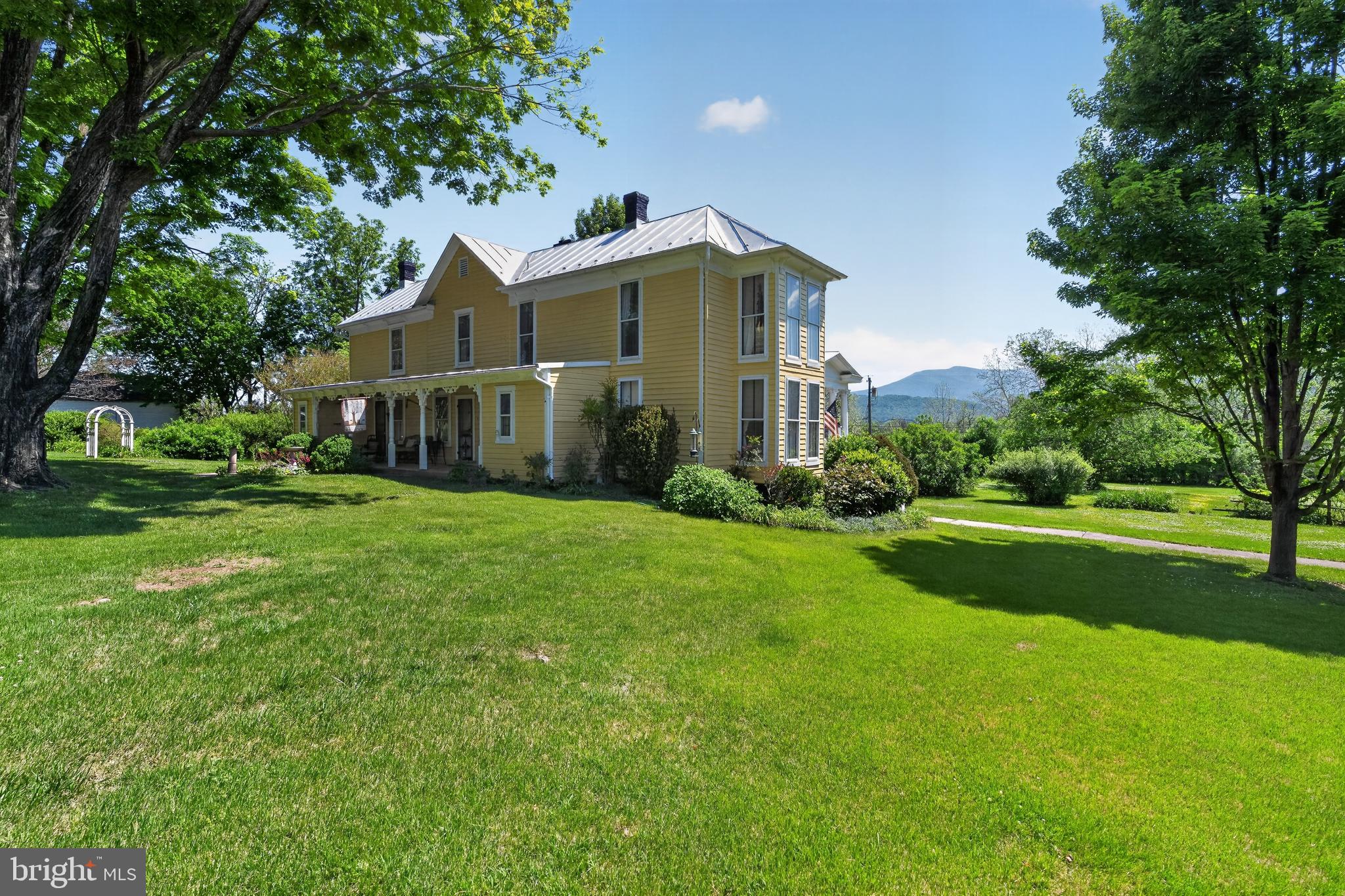 For more than a century, “The Ole Yellar House” has stood as one of the valleys most beloved landmarks, locals of generations have whispered about, admired, and waited decades to call their own. It’s golden façade glowing against the Blue Ridge backdrop like a beacon of welcome.
Built in 1885, this storied estate invites you to step into its narrative. Sunlight pours across warm hardwood floors that have carried generations of footsteps — each one adding to the home’s quiet, enduring soul. 4 gracious bedrooms and 2  timeless baths offer a blend of elegance and authenticity, where every detail feels intentional, preserved, and deeply loved. A lifetime of stories held gently in the walls.
Outside, the story widens. A picturesque barn stands proudly on the grounds, its weathered boards whispering tales of seasons past. Walking through the mature landscaping feels like stepping into a quiet, living sanctuary — shaded paths, blooming textures, and the sense that nature has been lovingly tending this home for generations. Wide porches wrap the home like an embrace, framing sweeping mountain views that shift with the light and the world seems to soften— morning mist, golden hour glow, and star drenched nights. It’s the kind of place where time slows, tea tastes sweeter, and the world feels a little softer.
Set just moments from Shenandoah National Park, renowned hiking trails, and the quiet charm of Virginia’s small mountain towns, this property offers a lifestyle rooted in beauty, serenity, and heritage. It is a sanctuary, a storybook, and a once in a generation opportunity.
So many have waited for this moment — watching, hoping, imagining. Now the next chapter belongs to you. Claim the legacy. Live the story. Welcome home to The Ole Yellar House.